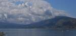 Blick über den See von Annecy auf das hügeliges Gelände und die tief hängenden Wolken an den Bergspitzen.