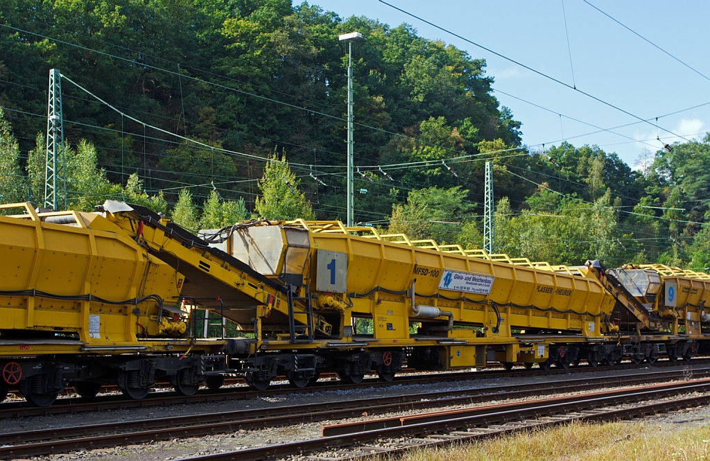 Plasser & Theurer Materialfrder- und Siloeinheit MFSD 100 der MGW Gleis- und Weichenbau-GmbH (Berlin) Nr. 1 (Schweres Nebenfahrzeug Nr. 97 19 29 55057-4) EBA-Nr. 00 D05 A009,  abgestellt in Betzdorf/Sieg am 22.09.2012.
Die MFS 100 und dienen zum Transport von Schotter, Abraum und Pufferspeicher bei der Bettungsreinigung bzw.Planumsverbesserung. Hauptvorteil ist der kontinuierliche Frder-, Speicher- und Entladevorgang. Eine Zusammenstellung von beliebig vielen MFS-Wagen zu einem Zug mit jeweils gewnschter Speicherkapazittist mglich. Der  Fllvorganges beginnt beim  vordersten Wagen (in Arbeitsrichtung), die folgenden Wagen dienen als Frderstrae.
Die MFSD 100 sind nur als Durchlader einsetzbar, das bergabeband nicht schwenkbar,  somit keine Entladung zum Nachbargleis mglich.
Diese Einheit wurde 2003 unter der Fabriknummer 4064 gebaut.
Technische Daten: Lnge ber Puffer 22.900 mm > Lnge inkl. Frderband 26.550 mm > Achszahl 8 (2 Drehgestelle mit je 4 Achsen) > max. Achslast (beladen) 18t > Eigenmasse 54 t > max. zulssige Zuladung 90 t > Motorleistung 160 kW fr Antrieb der Frderbnder > max. Geschwindigkeit im Zugverband 100 km/h > max. Fassungsvermgen 68 m.