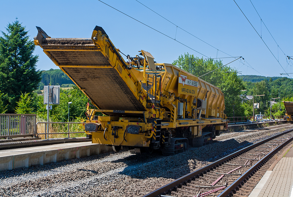 Baustelle im Bahnhof Katzenfurt (Lahn-Dill-Kreis) am 20.07.2013: Der MFS 40/4-A-ZW der H. F. Wiebe, Schweres Nebenfahrzeug 99 80 9052 002-9 D-GBM (ex 97 19 13 502 57-3) ist nun wieder leer und fährt auf seinen Raupenfahrwerken wieder zurück an den MFS 40/4-B-ZW.

Der MFS 40/4-A-ZW wurden 2009 von Plasser & Theurer unter der Fabriknummer 5480 gebaut und an die Wiebe Gleisbaumaschinen GmbH (Achim) geliefert.

Die MSF-ZW können sich durch seine beiden selbstständig angetriebenen Raupenfahrwerke im gleislosen Baustellenbereich fortbewegen, bzw. durch seine beiden Laufdrehgestelle, vorausgesetzt er besitzt vor sich einen MFS oder einen Schutzwagen mit Auflagerbock für vorragendes Schwenkband, in Züge eingestellt werde

Die beiden MFS 40/4-ZW sind für den gleislosen Einsatz konzipiert. Der MFS 40/4-ZW-B ist, im Bereich des Beladebandes, mit einem Bagger ausgerüstet, mit dessen Hilfe das vorhandene Planum/Aushub aufgenommen und über das Förderband in den Bunker befördert und gespeichert wird. Ist der Bunker fast voll, fährt der ebenfalls mit Raupenfahrwerken ausgestatteten MFS 40/4-ZW-A heran und der Aushub wird an ihn übergeben. Der MFS 40/4-ZW-B kann kontinuierlich weiter arbeiten, während nun der MFS 40/4-ZW-A, in der Zwischenzeit das Material auf im Gleis stehende gleisgebundene MFS, bringt und an diese übergibt. Die MFS sind mit einer eigenen Energieversorgungseinheit ausgestattet, wodurch ein individueller, also voneinander unabhängiger, Einsatz gewährleistet ist.  

TECHNISCHE DATEN des MFS 40/4-ZW-A:
Hersteller: Plasser & Theurer, Fabriknummer 5480 (2009)
Spurweite: 1.435 mm (Normalspur) / oder auf Raupenfahrwerke
Gesamtlänge: 23.840 mm (über alles) 
Länge über Puffer: 19.900 mm
Drehzapfenabstand: 13.000 mm
Breite: 3.150 mm
Höhe: 3.950 mm
Eigengewicht: 66.200 kg
Gesamtgewicht auf Drehgestell: 87.000 kg (leer)
Gesamtgewicht auf Raupe beladen: 126 t
Eigenfahrgeschwindigkeit auf Raupen: bis 3 km/h
Eigenfahrgeschwindigkeit im Gleis: bis 5 km/h
Max. Siloinhalt: 40 m³
Förderleistung: 500 m³/h
Kleinster befahrbarer Gleisbogen: R 150 m
Dieselmotor: wassergekühlter 6-Zylinder Reihenmotoren mit Common-Rail-Einspritzsystem, Turboaufladung und Ladeluftkühlung, vom Typ Deutz TCD 2013 L06 2V mit einer Leistung von 160 kW  
Höchstgeschwindigkeit im Zugverband: 100 km/h (geschleppt)