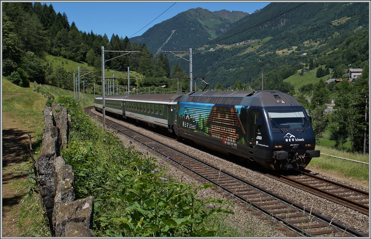 Das  behäbige  Bauernhaus auf der Re 460 023-5 jedoch will nicht so ganz in die alpensüdländliche Landschaft passen. Links im Bild sieht man die typischen, auf weiten Strecken der Südrampe die Gotthardbahn säumenden Steinplatten, ganz im Hintergrund ist die steilste Standseilbahn von Piotta ach Piora (Ritom) zu erahnen. 24. Juni 2015