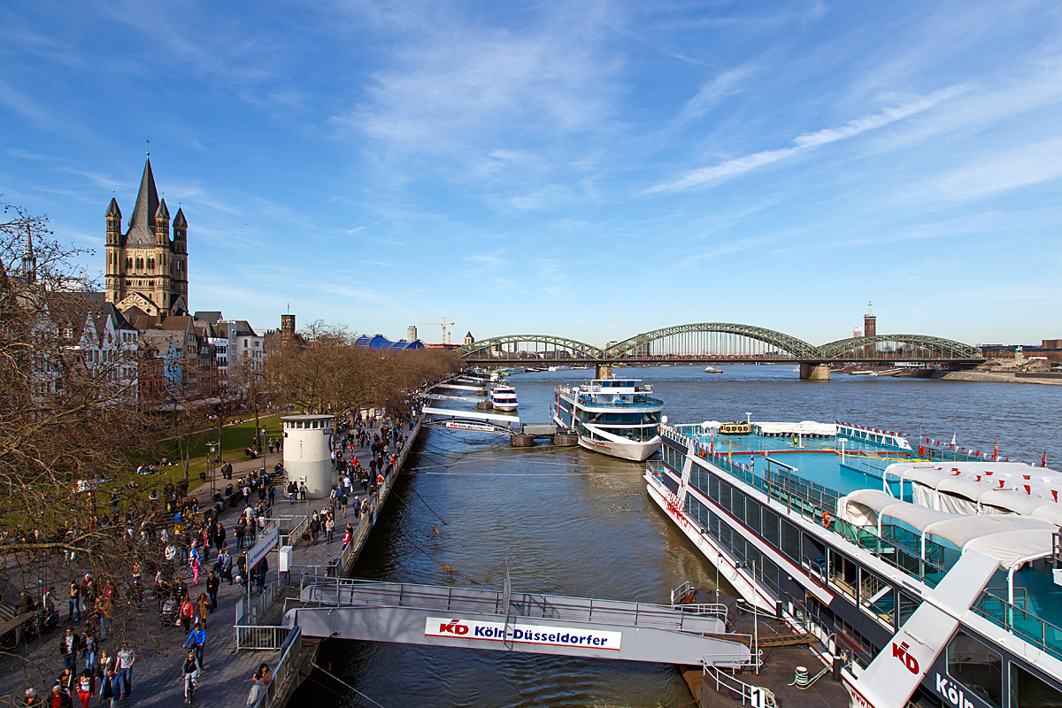 
Der Blick auf die Hohenzollernbrcke in Kln am 08.03.2015. 

Etwas weiter rechts von ihr befindet sich der Bahnhof Kln Messe/Deutz (nicht im Bild) und links von ihr ist der Hauptbahnhof.

Die Hohenzollernbrcke wurde von 1907 bis 1911 gebaut.Sie ersetzte die Dombrcke, die den Anforderungen des stetig zunehmenden Eisenbahnverkehrs nicht lnger gewachsen war. Das Besondere am Bau der neuen Brcke war, dass sie unter laufendem Betrieb der Dombrcke errichtet wurde und diese nach und nach ersetzte. Sie bestand nach ihrer Fertigstellung aus drei nebeneinander liegenden Fachwerkbogenbrcken mit jeweils drei Bgen.

Ein Teil war zu dieser Zeit, wie auch bei der Dombrcke, dem Straen- und Straenbahnverkehr vorbehalten, whrend die beiden anderen Teile vier Gleise aufnehmen konnten. Zustzlich gab es auf beiden Seiten Geh- und Radwege.

Die Hohenzollernbrcke ist die einzige Brcke in Kln, die nicht durch Bomben zerstrt wurde. Vielmehr bernahm es die Wehrmacht am 6. Mrz 1945 selbst, den herannahenden Alliierten durch Sprengung der Brcke eine Rheinberquerung zu erschweren. Nach dem Krieg wurde bis 1948 zunchst eine der (zweigleisigen) Bahnbrcken wieder aufgebaut. Die Straenbrcke wurde aus verkehrlichen Grnden nicht wiederhergestellt. In den Jahren 1956 bis 1959 und von 1986 bis 1987 wurde jeweils ein weiterer Fachwerkbogen hinzugefgt, so dass die Bahn heute ber sechs Gleise auf der Hohenzollernbrcke verfgt. Die zwei nrdlichen Gleise sind der S-Bahn vorbehalten. Bei der Hohenzollernbrcke gibt es zu beiden Seiten Geh- und Radwege, die von der Stadt Kln unterhalten und gepflegt werden, whrend sich die Brcke selbst, wie auch die Sdbrcke, im Eigentum der Deutschen Bahn AG befindet.

Mit etwa 1220 Zugfahrten pro Tag ist sie eine der meistbefahrenen Eisenbahnbrcken in Deutschland.  Das Bauwerk gilt, zusammen mit dem Klner Hauptbahnhof, als zentraler Engpass im Schienenverkehr in der Region Kln.

Technische Daten:
Typ: sechsgleisige Eisenbahnbrcke mit Geh- und Radwegen auf beiden Seiten
Bauart: drei nebeneinander liegende Fachwerkbgenbrcken
Baujahre: je eine Brcke 1946 bis 1948, 1956 bis 1959 und 1986 bis 1987
Spannweiten: 111,88 Meter - 167,75 Meter - 122,56 Meter, insgesamt 409,19 Meter
Gesamtbreite: 26,20 Meter 