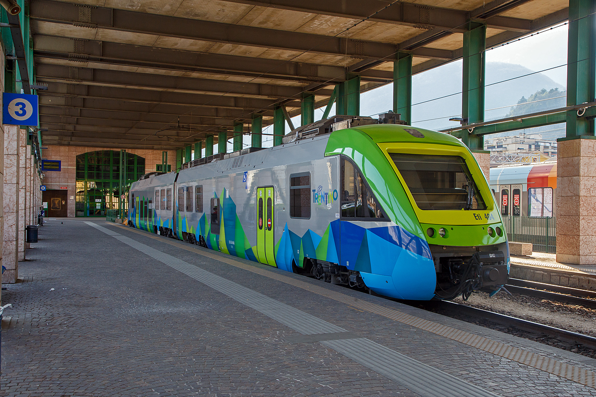 Der Eti 8/8 – 404 der Ferrovia Trento-Malè (FTM) steht am 26.03.2022 im Schmalspurbereich vom Bahnhof Trento/Trient.

Dier Elektrotriebzug ETi 400 (ETi 8/8) von der Ferrovia Trento-Malè (FTM) ist ein zweiteiliger Elektrozug mit einer Spurweite von 1.000 mm für den Nahverkehr, der zur Familie Alstom Coradia Meridian gehört. Seit 2005 wurden 14 Exemplare von Alstom Ferroviaria S.p.A. in Savigliano gebaut, die in der Serie Eti 8/8 401-414 registriert sind und den Spitznamen „kleiner Bär“ tragen.

Der Aufbau besteht aus zwei Niederflur-Fahrzeugteilen und ist gewichtssparend aus laminiertem Aluminium gefertigt. An Bord gibt es einen Bereich für den Transport von Fahrrädern und auf jeder Seite zwei Türen, in deren Nähe sich zwei Behindertenplätze befinden. Zu diesen ist auch die Toilette nutzbar. Der Antrieb erfolgt über 8 Drehstrom-Asynchronmotoren über Umrichter, jeweils mit Scheibenbremsen und lastvariabler Luftfederung von Knorr-Bremse. Das Bremsen erfolgt hauptsächlich elektrisch, aber unter 10 km/h wird pneumatisch gebremst. Der ETi 400-Zug verwendet ein RailMaster-Kommunikationssystem, das GPS- und GSM-Datenleitungen verwendet. Im Juni 2012 wurde die Installation des ATP-Sicherheitssystems abgeschlossen. Die Triebwagen sind mit einer Klimaanlage ausgestattet.

TECHNISCHE DATEN:
Hersteller: Alstom Ferroviaria S.p.A. in Savigliano (Italien) / 2005
Gebaute: 14
Spurweite: 1.000 mm (Meterspur)
Achsfolge: Bo´ Bo´+ Bo´ Bo´
Gebaute: 14
Länge: 40.200 mm
Breite: 2.650 mm
Höhe: 3.860 mm
Drehzapfenabstände: 6.800 mm
Leergewicht: 75,8 t
Leistung: 1.360 kW / 1.850 PS (8 x 170 kW)
Anfangsbeschleunigung: 1,1 m/sec²
Höchstgeschwindigkeit: 120 km/h
Motoren: 8 Stück Drehstrom-Asynchronmotoren
Stromsystem: 3 kV DC
Sitzplätze: 98 + 6 Klappsitze
Stehplätze: 140
Behindertenplätze: 2
Behindertentoilette: ja

Diese Triebzüge befahren die Bahnstrecke Trient – Malè – Mezzana, offiziell Ferrovia Trento – Malè – Mezzana, ist eine meterspurige und elektrifizierte Schmalspurbahn. Sie führte ursprünglich von Trient nach Malè und wurde 2003 nach Marilleva und 2016 weiter nach Mezzana verlängert. Betrieben wird sie heute von Trentino Trasporti S.p.A., dem Unternehmen der Autonomen Provinz Trient für den öffentlichen Personennahverkehr. Der frühere Name der Betreibergesellschaft lautete Ferrovia Elettrica Trento-Malè (FETM) beziehungsweise Ferrovia Trento-Malè (FTM). Die Bahn ist ferner auch unter dem deutschen Namen Nonstalbahn bekannt, weil sie in das gleichnamige Tal führt.

Die Strecke beginnt beim Bahnhof Trento FS und führt den Talboden entlang mit mehreren Betriebsausweichen zur Station Mezzocorona, wo Anschluss an das Netz der Trenitalia besteht. Ab Mezzolombardo verlässt die Strecke den Talboden und steigt ins Nonstal an. Über zahlreiche Viadukte und Tunnels wird schließlich die neue Endstation Mezzana erreicht. Die wohl spektakulärste Brücke ist der 1959 eingeweihte Santa-Giustina-Viadukt über den Fluss Noce, mit einer Spannweite von 78 Metern und einer Höhe von 140 Metern die zu ihrer Zeit höchste Bahnbrücke der Welt. Die maximale Steigung beträgt 50 Promille, der kleinste Kurvenradius 80 Meter.Die Höchstgeschwindigkeit beträgt 90 km/h. Derzeit verkehren manche Kurse nur bis/ab Malè und zur Verstärkung werden Schnellkurse angeboten.
