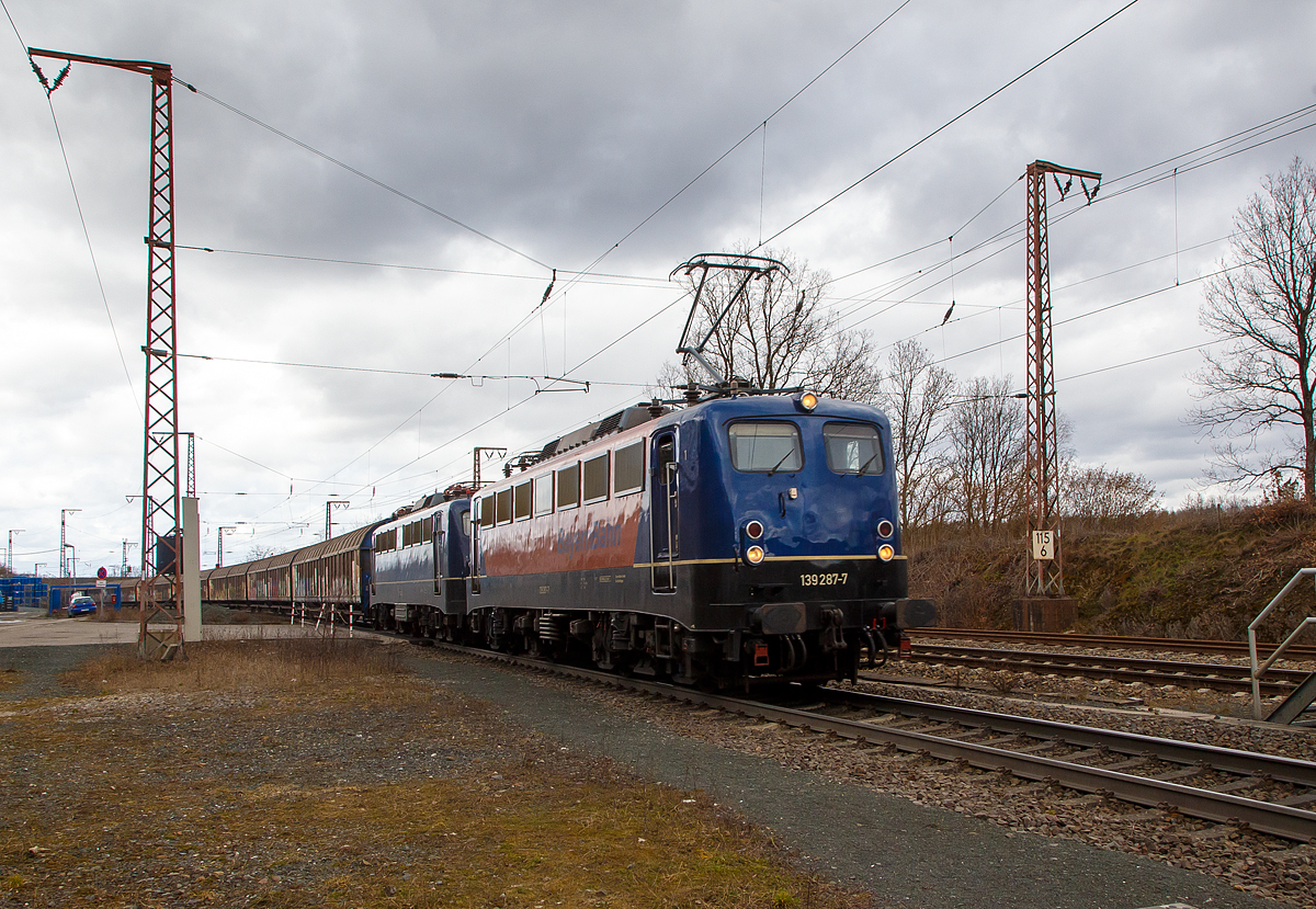 Die 139 287-7 (91 80 6139 287-7 D-BYB) mit der kalten 139 262-0 alias 110 262-3 (91 80 6139 262-0 D-BYB) beide von der BayernBahn GmbH fahren am 12.03.2021 mit dem sogenannten  Henkelzug  (Langenfeld/Rhld. nach Gunzenhausen), durch Rudersdorf (Kr. Siegen) in sdlicher Richtung bzw. Richtung Dillenburg.

Die 139 287-7:
Vorne die 139 287-7 wurde 1963 von Krauss-Maffei AG in Mnchen-Allach unter der Fabriknummer 18956 gebaut, der elektrische Teil ist von den Siemens-Schuckert-Werke (SSW) in Berlin. Als DB E10 287 wurde in Dienst gesetzt, mit der Einfhrung des EDV-Nummernsystems wurde sie zum 01.01.1968 zur DB 110 287–0. Die Lok ist mit Einholmstromabnehmern ausgerstet, sie ist die letzte gebaute Kasten 110er. Zur 139er wurde sie erst 1994 nach einem Umbau, der Lokkasten wurde auf Drehgestelle der Baureihe 140 (E40) gesetzt und es folgte die Umzeichnung in DB 139 287-7. Zum Mai 2009 erfolgte die Z-Stellung bei der DB AG. Zum 1.Oktober 2011 wurde die Lok durch die BayernBahn GmbH erworben und erhielt anschlieend eine Untersuchung. Die Neulackierung in kobalt-blau/orange erhielt sie dann 2017.

Die 139 262-0 alias 110 262-3:
Die 139 262-0 wurde 1962 von Krauss-Maffei AG in Mnchen-Allach unter der Fabriknummer 18921 gebaut, er elektrische Teil ist von den Siemens-Schuckert-Werke (SSW) in Berlin. Als DB E 10 262 wurde in Dienst gesetzt, mit der Einfhrung des EDV-Nummernsystems wurde sie zum 01.01.1968 zur DB 110 262-3. Auch sie wurde erst 1994, nach dem Erhalt von Drehgestellen der Baureihe 140 (E40) zu einer 139er. Nach dem Umbau wurde sie in DB 139 262-0 umgezeichnet. Ende April 2012 erfolgte die Z-Stellung bei der DB AG und im Mai 2015 wurde sie an die BayernBahn GmbH verkauft und erhielt anschlieend eine Untersuchung. Die Neulackierung in stahlblau erhielt sie dann 2016.
