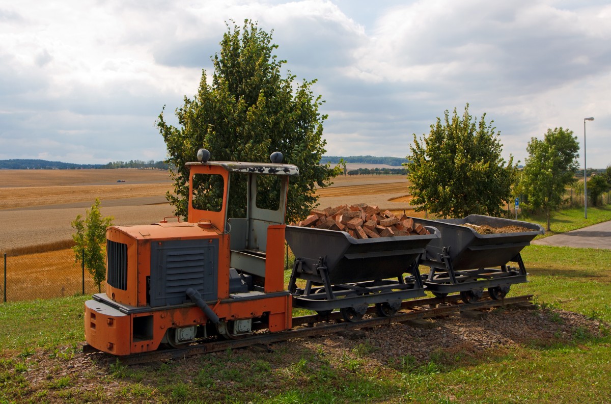 Die 600mm  LKM Ns1b  Diesel-Feldbahnlok, als Denkmallok mit zwei Loren bei Amand Umwelttechnik in Grumbach bei Freital, am 26.08.2013 aufgenommen vom Gehweg aus. 

Die Lok vom Typ Ns 1 b wurde 1960 vom VEB Lokomotivbau Karl Marx Babelsberg (LKM) unter der Fabriknummer 260103 gebaut und an den VEB Ziegelwerk in Grumbach geliefert. 

Diese kleinste Lok des LKM-Typenprogramms entspricht in Aufbau, Größe und Leistung der Jung-Lok EL 105, sogar das Getriebe beider Loks ist austauschbar. Mit ihrem geringen Gewicht und dem kurzen Achsstand war sie auch auf Gleisanlagen mit kleinem Schienenprofil und schwachem Unterbau zu fahren. Der ursprüngliche stehende Einzylindermotor wurde später (wie bei vielen Ns 1 b) durch einen Vierzylinder-V-Motor ersetzt, was Improvisationen an der Auspuffanlage erforderlich machte: An beiden Seiten der Motorverkleidung wurden die Bleche aufgeschnitten und Auspuffrohre mit Schalldämpfern durchgeführt.

Technische Daten:
Hersteller:  LKM
Fabriknummer:  247418
Baujahr:  1957
Spurweite: 600 mm (Lieferbar war 485 mm ဓ 600 mm)
Bauart:  B-dm
Leistung:  15 PS Nenndrehzahl:  1500/min
Dienstgewicht:  2,8 t
Länge über Puffer:  2.320 mm
Breite:  1.020 mm
Höhe:  2.355 mm (mit Führerhaus)
Achsstand:  720 mm
Zugkraft:  500 kg
Geschwindigkeit:  8 km/h
Kleinster bef. Halbmesser:  7,5 m
Treibraddurchmesser:  376 mm
Leistungsübertragung:  mechanisch, Kette
Übersetzungsstufen:  2
Bremse:  Handhebelbremse
Kupplungstyp:  Ketten-Kupplung

Obwohl von der Type NS 1 ca. 700 Stück gebaut wurden, hat ihre Zahl nach der deutschen Einheit erheblich abgenommen. Während die Stillegung von Feldbahnen in der BRD seit den 60er Jahren allmählich verlief, vollzog sich dieser Prozess in den neuen Bundesländern durch Werksschließungen oder Umstellung der Förderung auf LKW oder Bandförderung innerhalb weniger Jahre. 