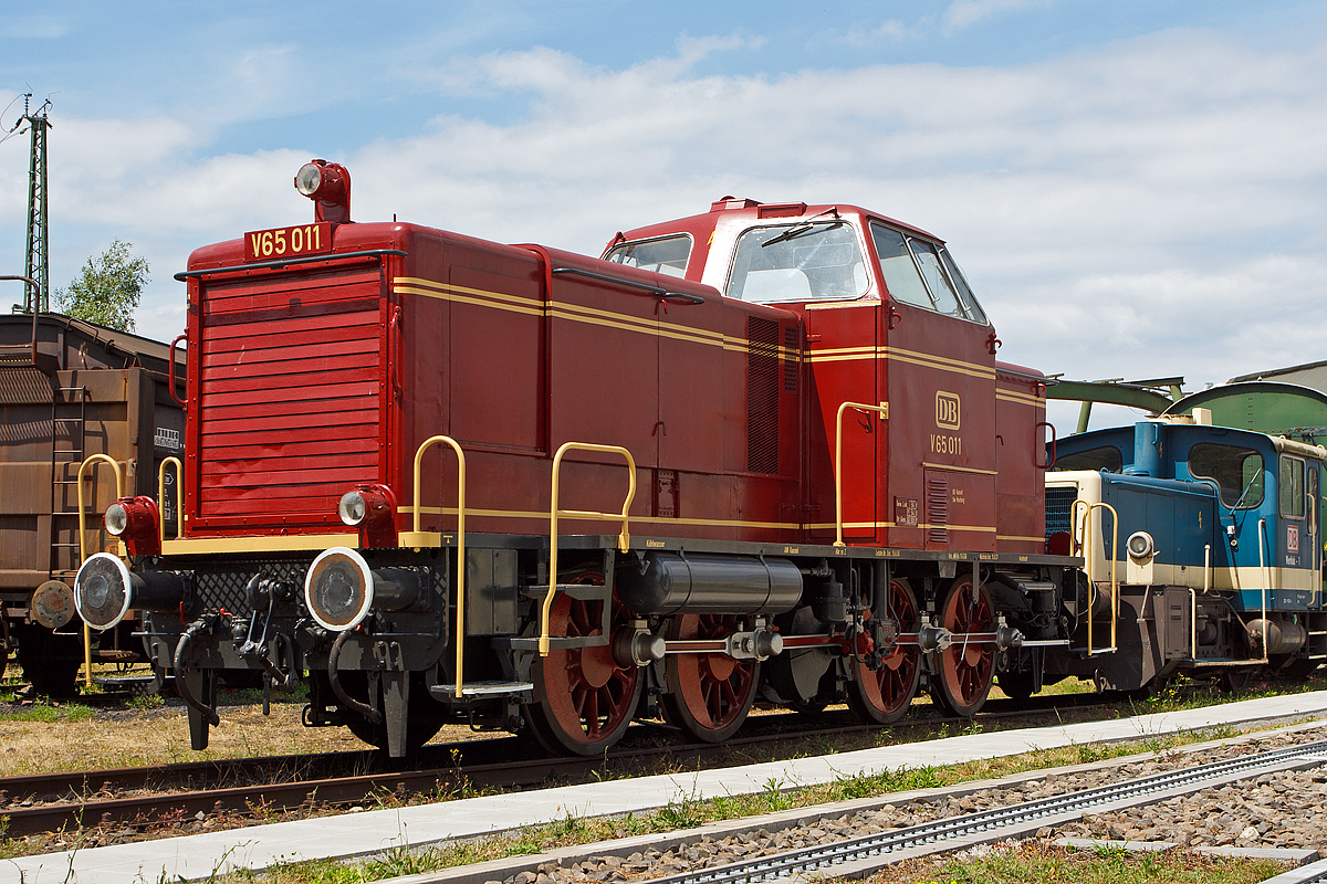 
Die DB V 65 011, ex DB 265 011-7, am 22.06.2014 im DB Museum Koblenz-Lützel.

Die V 65 wurde 1955 bei MaK (Maschinenbau Kiel) unter der Fabriknummer 600014 gebaut und als V 65 011 an die Deutsche Bundesbahn (DB) geliefert. Die Umzeichnung in DB 265 011-7 erfolgte 1968, die Ausmusterung bei der DB 1977. Seit 2011 ist sie nun hier im DB Museum Koblenz. 

Für den Einsatz auf Nebenbahnen wurde die aus der zum ersten Typenprogamm von MaK gehörigen 600 D die V 65 der DB entwickelt und in 15 Exemplaren an die DB geliefert. Neben der etwas höheren Motorleistung unterscheidet sie sich in diversen Details von der 600 D. Äußerlich am auffälligsten sind die glatten Seiten der Motorhaube, die waagerechten Lamellen des Frontlüfters und die freistehenden Lampen. Ebenfalls neu ist der mit Koks betriebene Dofa-Ofen zum Vorwärmen und Warmhalten.

Nachdem ein Weiterbau der V 65 zugunsten der V 100.10 aufgegeben wurde, kam diese Splittergattung bis 1964 zunächst im Nebenbahndienst im Raum Marburg/Lahn zum Einsatz, wobei neben Güterzügen auch der Personenverkehr auf dem Dienstplan stand. Anschließend gelangten die Loks in den Norden und verdiente ihr Gnadenbrot im Rangierdienst in Hamburg-Altona, Hamburg-Harburg und Puttgarden.

Die Technik der V65 
Die Lok ist auch technisch interessant: Erst mit der V16 wurde es kurz vor dem Krieg möglich, die Kraft des Motors hydraulisch zu übertragen. Im Gegensatz zur Dampfmaschine kann der Dieselmotor nicht aus dem Stand ziehen. Eine Kupplung wie im KFZ würde die Kräfte und Gewichte der Eisenbahn nicht überleben. Während des Krieges wurden nur Rangierdieselloks für die Wehrmacht in dieser Technik gebaut. Nach dem Krieg war die V 65 die erste hydraulische Streckendiesellok. Als Antriebsmaschine dient ein langsam laufender MaK- 6-Zylinder- Schiffsdiesel vom Typ MS 301 C mit 72 Liter Hubraum. Das hört man besonders beim Beschleunigen und Starten der Lok. Vom Strömungsgetriebe wird die Kraft auf eine Blindwelle übertragen und gelangt von dort mit Treibstangen auf die vier Achsen- wie bei der Dampflok
Der Stangenantrieb war die Ursache, dass nur 15 Exemplare gebaut wurden. Für höhere Geschwindigkeiten hat man Dampfloks größere Räder gegeben, um die Drehzahl zu begrenzen. Man stelle sich einmal die V65 mit 2m -Rädern der BR 01 Schnellzugdampflok vor.
Ein großer, langsam laufender Dieselmotor darf nicht einfach kalt gestartet werden. Der Verschleiß wäre enorm. So wird die Lok ca. zwei Stunden “vorgeheizt”, ähnlich einer Dampflok. Nur wird hier nicht Kesselwasser erhitzt, sondern das Motoröl. Ab einer Temperatur von etwa 40° C kann der Motor gestartet werden. 

Für 72 Liter Hubraum gibt es keinen Elektrostarter. Deshalb wird der Motor mit Druckluft von 30 bar gestartet. Das ist ein akustisches Schauspiel.

Die Kraftübertragung von der Blindwelle zu den Achsen über Kuppelstangen stellt den technischen Übergang von der Dampflok zur modernen Lok dar. Auch viele Ellok Typen aus der Länderbahnepoche zeigten diese archaische Technik. Damit war allerdings die Höchstgeschwindigkeit begrenzt. Man konnte nicht die Räder vergrößern, wie bei Dampflokomotiven. Das war einer der Hauptgründe für die DB, sich bei Streckenlokomotiven für den Antrieb über Drehgestelle zu entscheiden.

Im Gegensatz zu späteren Lieferungen an Privatbahnen, hatten die DB- Lok freistehende Laternen, wie Dampflokomotiven

Bis 1980 wurde die gesamte Baureihe ausgemustert, nachdem vor allem die Gewerkschaften auf eine vorzeitige Ausmusterung drängten: Durch den langsam laufenden MaK-Motor soll sich im Führerhaus regelmäßig eine beträchtliche Hitze entwickelt haben.

Von den 15 gebauten Loks blieben mit V 65 001 und V 65 011 nur zwei in Deutschland erhalten. Die ehemalige V 65 004 hingegen geht in Italien einer ungewissen Zukunft entgegen.

Technische Daten:
Spurweite:  1435 mm
Achsfolge:  D
Länge über Puffer:  10.740 mm
Achsstand:  5.800 mm
größte Breite:  3.100 mm
größte Höhe über Schienenoberkante:  4.150 mm
Raddurchmesser neu:  1.250 mm
kleinster befahrbarer Gleisbogen:  50 m
Dienstgewicht:  54 t
Kraftstoffvorrat: 1.130 l
Heizbrennstoff Koks: 100 Kg
    
Motor : MaK- 6-Zylinder- Viertakt-Schiffsdiesel vom Typ MS 301 C
Leistung:  650 PS (479 kW)
Drehzahl: 750  U/min
Hubraum: 72 Liter

Getriebe: Voith Typ  L 37 z
Höchstgeschwindigkeit  80 km/h