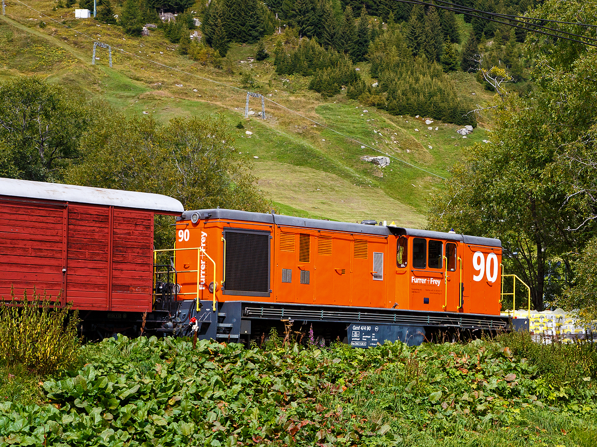 Die Die Furrer + Frey Gmf 4/4 90 abgestellt am 07.09.2021 beim DFB Bahnhof Realp  (1.538 m ü. M.). 

Eine ehemalige modernisierte und umgespurte rumänische FAUR L 45 H (Baujahr 1969 unter Fabriknummer 20867 in Spurweite 760 mm), die ex CFR 87-0023-9 (C.F.R. steht für Căile Ferate Române der staatlichen Eisenbahngesellschaft Rumäniens.

Weil es etwas länger ist fange ich mit der Zusammenfassung und den Technischen Daten an, wer es ausführlich mag kann sehr gerne weiterlesen.

Zusammenfassung:
Der Fahrleitungsbauer Furrer + Frey in Bern hat im Oktober 2014 eine vierachsige Diesellokomotive aus Rumänien mit rund 500 kW Leistung an der Welle nach Umbau und Hauptrevision erfolgreich in Betrieb genommen. Die Arbeiten hatte das Werk Krieglach der Tecsol GmbH in der Steiermark in weniger als zehn Monaten ausgeführt. Dabei wurde die Lokomotive von bosnischer Spur (760 mm) auf Meterspur umgebaut und mit einem modernen Dieselmotor ausgerüstet. Nach erfolgreicher dynamischer Inbetriebsetzung bei der MGB ist die Gmf 4/4 90 seit Mitte
Oktober 2014 für Einsätze auf den meterspurigen  Adhäsions-Bahnnetzen in der Schweiz bereit.

TECHNISCHE DATEN der Adhäsions-Diesellokomotive Gmf 4/4 90
Spurweite:  1.000 mm
Achsanordnung:  B’ B’ (4 Triebachsen)
Länge über Puffer:12.000 mm
Breite über Rahmen: 2.440 mm
Breite über Kasten: 2.200 mm
Höhe: 3.320 mm
Drehzapfenabstand: 5.500 mm
Achsabstand im Drehgestell :1.700 mm
Raddurchmesser:  750mm (neu) / 710 mm (abgenutzt)
Dienstgewicht: 40 t
Maximale Radsatzlast: 10 t
Antrieb: dieselhydraulisch
Leistung Hauptdieselmotor:  520 kW bei 2100 U/min, gedrosselt auf 490 kW bei 1800 U/min 
Leistung Hilfsdieselmotor: 50 kW bei 1500 U/min
Anfahrzugkraft bis 10 km/h:  90 kN
Höchstgeschwindigkeit: Schnellgang 50 km/h / Rangiergang 22 km/h (55 km/h geschleppt)
Kleinster befahrbarer Kurvenradius: 45 m
Kraftstoffvorrat: 970 Liter
Anhängelasten: bis 70 ‰ mit bis 50 t bei 10 km/h

Seit mehr fast Jahren projektiert und baut die in Bern ansässige Firma Furrer + Frey AG Fahrleitungen für normal- und schmalspurige Eisenbahnen, Bergbahnen, Trambahnen und Trolleybusse im In- und Ausland. 2013 standen für die kommenden Jahre bei mehreren Tunnelgewerken schweizerischer Meterspurbahnen Sanierungen und Arbeiten zur Erhöhung der Sicherheit an, die generell einen größeren Bedarf an meterspurigen thermischen Diensttriebfahrzeugen auslösten. In diesem Hinblick auf die damit anstehenden Erneuerungen und Neubauten von Fahrleitungen hatte sich F+F deshalb im Herbst 2013 entschieden, eine leistungsfähigere thermische Lokomotive Gmf 4/4 zu beschaffen. Umfangreiche Marktabklärungen zeigten, dass im gewünschten Zeitraum von weniger als einem Jahr einzig die Beschaffung einer gebrauchten und entsprechend den Bedürfnissen von F+F um zu bauenden Maschine kostengünstig und erfolgreich umzusetzen war.

Im Herbst 201 3 konnte die TecSol GmbH in Anger (Steiermark) kurzfristig eine vierachsige Umbau-Diesellokomotive rumänischer Herkunft anbieten, die die geforderten Eckwerte erfüllte. Die aus dem Jahr 1969 stammende Lokomotive vom Typ  Faur L45H mit der Fabriknummer 20867 ist eine von insgesamt 334 Exemplaren, die FAUR in Bukarest hergestellt hatte. Sie wurde 2014 in Krieglach (Steiermark) hauptrevidiert, remotorisiert und von bosnischer Spurweite (760 mm) auf Meterspur umgebaut. 

Von der ursprünglichen Lokomotive wurden der Rahmen, die Vorbauten, das Mittelführerhaus, das Verteilgetriebe und die beiden kardanisch angetriebenen Drehgestelle beibehalten. Die übrigen Komponenten, wie Dieselmotor mit Partikelfilter und Generatoren, Kühlanlage inklusive Kühlerventilator, 01- und Wasserpumpen, Hilfsdieselmotor, Generator-Gruppe mit Partikelfilter, Dieselölbehälter, Bordnetzumrichter, Kompressor, Vakuumpumpe, Druckluftgerüst, Magnetschienenbremsen und die Fahrzeugleittechnik, wurden neu eingebaut.

Mechanischer Teil:
Das Untergestell ist eine Schweißkonstruktion aus Walzprofilen, Blechen und Abkantprofilen. Der Rahmen wird gebildet aus je zwei äußeren und inneren Längsträgern, zwei Hauptquerträgern, mehreren diagonal und quer angeordneten Verstärkungsträgern sowie zwei kastenförmig angebauten Endplattform-Vorbauten. Er wurde verstärkt und auf eine Längsdruckfestigkeit von 800 kN ausgelegt. Auf dem Rahmen aufgebaut ist das Mittelführerhaus, an das am Ende I ein langer Vorbau und am Ende II ein kurzer Aufbau angrenzt. 

Für Einsätze bei verschiedenen Meterspurbahnen können die modular auf angeschraubten Adapter-Wechselplatten montierten schweizerischen Zug- und Stoßvorrichtungen: 
•	Zp1 , 500/750 mm über Schienenoberkante (SOK), für Einsatz unter anderem bei der Montreux - Berner Oberland-Bahn (MOB);
•	Zp2, 620 mm über SOK, für Einsatz unter anderem bei der Matterhorn – Gotthard Bahn (MGB) und bei der Rhatischen Bahn (RhB);
•	GFN  hoch , 620/650 mm über SO K, für Einsatz unter anderem bei der Biere - Apples -Morges-Bahn (MBC-BAM), bei den Berner Oberland-Bahnen (BOB), bei der MGB
•	GFN  tief , 500 mm über SOK, für Einsatz unter anderem beim Regionalverkehr Bern - Solothurn (RBS) und bei Aare - Seelandmobil (ASm).
auf einfache Weise mit Hilfe eines Krans oder Gabelstaplers gewechselt werden.

Das Drehmoment des Dieselmotors wird über ein im Rahmen gelagertes hydraulisches Turbogetriebe (Fahrtrichtungswahl und verschleißfreie Bremse) mit darunter angebautem Nachschaltgetriebe (Auswahl für Strecken-/Rangiergang) pro Drehgestell über eine Kardanwelle auf die unter sich in den Drehgestellen ebenfalls kardanisch gekuppelten Radsätze übertragen. Das Turbogetriebe lässt dank den pro Fahrtrichtung getrennten Wandlern verschleißfreie Bremsungen zu, womit das Befahren starker Gefälle möglich ist (Steilstreckenfähigkeit).Jedes Drehgestell verfügt über zwei Bremszylinder, die auf die je einseitig pro Rad angeordnete Bremsklötze wirken. Als Feststellbremse wirkt pro Drehgestell je ein Federspeicher-Bremszylinder.

Thermischer Teil:
Die Lokomotive ist mit einem im Rahmen gelagerten sechszylindrigen Hauptdieselmotor Caterpillar C18 mit rund 500 kW Leistung an der Welle und einer Dieselpartikelfilteranlage ausgerüstet. Weiter ist ein Hilfsdieselmotor-Generator-Aggregat mit einer Leistung von 50 kVA mit Partikelfilter installiert. Damit wird die Energieversorgung 3 x 400 V auch bei abgestelltem Hauptdieselmotor gewährleistet, was bei Arbeitseinsätzen in Talrichtung markante Treibstoff-Einsparungen ermöglicht. Die Lokomotive entspricht den in der Schweiz geltenden Vorschriften für den Gesundheitsschutz auf Untertagebaustellen. Dadurch sind die Voraussetzungen für Einsätze dieser Lokomotive auch bei Arbeiten in allen Bahntunneln gegeben.

Elektrischer Teil:
Die Lokomotive verfügt über ein Steuerstromnetz 24 V DC und eine zusätzliche 12-V-Batterie für den Hilfsdieselmotor. Zudem erzeugt ein DC/DC-Wandler aus dem 24-V-Netz 110 V für die Steuerung des Kompressors. Vom Hauptdieselmotor über Keilriemen angetriebene zwei kleinere Generatoren erzeugen das Bordnetz 3 x 400 V AC. Über je einen eigenen Frequenzumrichter werden der Kompressor, die Vakuumpumpe und der Kühlerventilator frequenzvariabel betrieben. Die beiden Zusatzöl- und Zusatzkühlwasserpumpen für den hydraulischen Bremsbetrieb, die Kühlwasservorheizung des Hauptdieselmotors, die Zusatzheizung für den Führerraum sowie die beiden Umwälzpumpen für die Kühlwasservorwärmung des Hauptdieselmotors und die Umwälzpumpe für die Führerraumheizung werden mit konstanter Frequenz von 50 Hz ab dem Bordnetz versorgt. Alternativ wird das Bordnetz über die Fremdeinspeisungsstecker ortsfest gespeist. Die 24-V-Batterieladung erfolgt von der Lichtmaschine des Hauptdieselmotors. Möglich ist aber auch von der Sammelschiene 3 x 400 V über einen Transformator 400 V / 230 V oder über die einphasige Fremdeinspeisung mit 230 V AC. Die 12-V-Batterieladung erfolgt von der Lichtmaschine des Hilfsdieselmotors oder über die 230-V-Fremdeinspeisung. Da der Hilfsdieselmotor mit 12 V angelassen wird, könnte die Lokomotive bei leeren Batterien auch mit einem Überbrückungskabel von jedem Auto aus wieder gestartet werden.

Stirnseitig ist an beiden Vorbauten je eine Kamera zur besseren Beobachtung des Fahrweges mit Bildübertragung auf einen Monitor pro Führerpult installiert. Die eingebaute Funkfernsteuerung  LocControl 100  erlaubt dem Lokomotivführer die Bedienung auch außerhalb des Führerstandes. Zwei gelbe Leuchten auf dem Dach zeigen den aktiven Funkfernsteuerbetrieb an. Vor Beginn einer Bewegung geben Rückfahrwarner beidseitig in der Gleisachse drei kurze Töne zur Warnung von Personen im Gleisfeld ab. Blaue Leuchten auf dem Dach zeigen zudem Störungen oder zwingend erforderliche Handlungen des Lokomotivführers vor der Weiterfahrt an.

Pneumatischer Teil und Bremsen:
Die Lokomotive ist grundsätzlich druckluftgebremst, sie kann sowohl mit Vakuum als auch mit Druckluft gebremste Anhängelasten mitführen. Die Druckluftbremse der Lokomotive wirkt über ein Pilotventil auch vakuumgesteuert als automatische Bremse von der Vakuum-Hauptleitung her. Die Lokomotive verfügt über Klotzbremsen mit zwei Bremszylindern pro Drehgestell und je einer Samson-Bremssohle mit 3 % Phosphorgehalt pro Rad. Diese werden über die automatische Druckluftbremse (wahlweise mit 5 oder 4 bar Regeldruck), über die elektrisch gesteuerte direkte Bremse (Rangierbremse), über die Vakuumbremse mit einem Regeldruck von - 52 cm Hg oder über die Federspeicher-Feststellbremse zur Wirkung gebracht. Als Feststellbremse sind zwei Federspeicherzylinder in den beiden Vorbauten integriert. Pro Drehgestell ist ein Steuerventil zur automatischen Druckluftbremse vorhanden. Zusätzlich bremst eine verschleißfreie hydraulische Retarderbremse das Fahrzeug und ermöglicht seine Steilstreckenfähigkeit. Die Ausführungsbestimmungen zur schweizerischen Eisenbahnverordnung verlangen beim Befahren von Strecken mit unabhängigem Bahnkörper und mehr als 60‰ Neigung (unter anderem MOB, Berninabahn der RhB) eine Sicherheitsbremse, die von der Reibung zwischen Rad und Schiene unabhängig ist. Zur Erfüllung dieser Forderung dient eine Magnetschienenbremse.

Inbetriebnahme:
Im Herbst 2014 folgten zwei sehr intensive Wochen mit dynamischen Inbetriebsetzungsfahrten auf dem Netz der MGB zwischen Ackersand , Visp, Brig und Grengiols, sowie am Nätschen unterhalb der 2.033 Meter hohen Station Oberalppass. Dabei konnten die einwandfreie Funktion der Lokomotive festgestellt und die nötigen Feineinstellungen vorgenommen werden. Bremswegmessungen und Lastfahrten mit 50 t Anhängelast auf den bis zu 70 ‰ steilen Abschnitten der MGB wurden Anfang Oktober ebenfalls erfolgreich absolviert. Am 10. Oktober 2014 kontrollierte das Bundesamt für Verkehr (BAV) die Lokomotive im Rahmen der technisch-betrieblichen Sicherheitsprüfung zwischen Brig und Ackersand. Wenige Tage nach der erfolgreichen Abnahme durch das BAV und nach zwei Tagen Triebfahrzeugführerschulung ging die Lokomotive in Einsatz.

Quelle: Furrer + Frey (mit Eisenbahn-Revue 12/2014)
 Gmf 4/4 90 abgestellt am 07.09.2021 beim DFB Bahnhof Realp  (1.538 m ü. M.). 

Eine ehemalige modernisierte und umgespurte rumänische FAUR L 45 H (Baujahr 1969 unter Fabriknummer 20867 in Spurweite 760 mm), die ex CFR 87-0023-9 (C.F.R. steht für Căile Ferate Române der staatlichen Eisenbahngesellschaft Rumäniens.

Weil es etwas länger ist fange Zusammenfassung und den Technischen Daten an, wer es ausführlich mag kann sehr gerne weiterlesen.

Zusammenfassung:
Der Fahrleitungsbauer Furrer + Frey in Bern hat im Oktober 2014 eine vierachsige Diesellokomotive aus Rumänien mit rund 500 kW Leistung an der Welle nach Umbau und Hauptrevision erfolgreich in Betrieb genommen. Die Arbeiten hatte das Werk Krieglach der Tecsol GmbH in der Steiermark in weniger als zehn Monaten ausgeführt. Dabei wurde die Lokomotive von bosnischer Spur (760 mm) auf Meterspur umgebaut und mit einem modernen Dieselmotor ausgerüstet. Nach erfolgreicher dynamischer Inbetriebsetzung bei der MGB ist die Gmf 4/4 90 seit Mitte
Oktober 2014 für Einsätze auf den meterspurigen  Adhäsions-Bahnnetzen in der Schweiz bereit.

TECHNISCHE DATEN der Adhäsions-Diesellokomotive Gmf 4/4 90
Spurweite:  1.000 mm
Achsanordnung:  B’ B’ (4 Triebachsen)
Länge über Puffer:12.000 mm
Breite über Rahmen: 2.440 mm
Breite über Kasten: 2.200 mm
Höhe: 3.320 mm
Drehzapfenabstand: 5.500 mm
Achsabstand im Drehgestell :1.700 mm
Raddurchmesser:  750mm (neu) / 710 mm (abgenutzt)
Dienstgewicht: 40 t
Maximale Radsatzlast: 10 t
Antrieb: dieselhydraulisch
Leistung Hauptdieselmotor:  520 kW bei 2100 U/min, gedrosselt auf 490 kW bei 1800 U/min 
Leistung Hilfsdieselmotor: 50 kW bei 1500 U/min
Anfahrzugkraft bis 10 km/h:  90 kN
Höchstgeschwindigkeit: Schnellgang 50 km/h / Rangiergang 22 km/h (55 km/h geschleppt)
Kleinster befahrbarer Kurvenradius: 45 m
Kraftstoffvorrat: 970 Liter
Anhängelasten: bis 70 ‰ mit bis 50 t bei 10 km/h

Seit mehr fast Jahren projektiert und baut die in Bern ansässige Firma Furrer + Frey AG Fahrleitungen für normal- und schmalspurige Eisenbahnen, Bergbahnen, Trambahnen und Trolleybusse im In- und Ausland. 2013 standen für die kommenden Jahre bei mehreren Tunnelgewerken schweizerischer Meterspurbahnen Sanierungen und Arbeiten zur Erhöhung der Sicherheit an, die generell einen größeren Bedarf an meterspurigen thermischen Diensttriebfahrzeugen auslösten. In diesem Hinblick auf die damit anstehenden Erneuerungen und Neubauten von Fahrleitungen hatte sich F+F deshalb im Herbst 2013 entschieden, eine leistungsfähigere thermische Lokomotive Gmf 4/4 zu beschaffen. Umfangreiche Marktabklärungen zeigten, dass im gewünschten Zeitraum von weniger als einem Jahr einzig die Beschaffung einer gebrauchten und entsprechend den Bedürfnissen von F+F um zu bauenden Maschine kostengünstig und erfolgreich umzusetzen war.

Im Herbst 201 3 konnte die TecSol GmbH in Anger (Steiermark) kurzfristig eine vierachsige Umbau-Diesellokomotive rumänischer Herkunft anbieten, die die geforderten Eckwerte erfüllte. Die aus dem Jahr 1969 stammende Lokomotive vom Typ  Faur L45H mit der Fabriknummer 20867 ist eine von insgesamt 334 Exemplaren, die FAUR in Bukarest hergestellt hatte. Sie wurde 2014 in Krieglach (Steiermark) hauptrevidiert, remotorisiert und von bosnischer Spurweite (760 mm) auf Meterspur umgebaut. 

Von der ursprünglichen Lokomotive wurden der Rahmen, die Vorbauten, das Mittelführerhaus, das Verteilgetriebe und die beiden kardanisch angetriebenen Drehgestelle beibehalten. Die übrigen Komponenten, wie Dieselmotor mit Partikelfilter und Generatoren, Kühlanlage inklusive Kühlerventilator, 01- und Wasserpumpen, Hilfsdieselmotor, Generator-Gruppe mit Partikelfilter, Dieselölbehälter, Bordnetzumrichter, Kompressor, Vakuumpumpe, Druckluftgerüst, Magnetschienenbremsen und die Fahrzeugleittechnik, wurden neu eingebaut.

Mechanischer Teil:
Das Untergestell ist eine Schweißkonstruktion aus Walzprofilen, Blechen und Abkantprofilen. Der Rahmen wird gebildet aus je zwei äußeren und inneren Längsträgern, zwei Hauptquerträgern, mehreren diagonal und quer angeordneten Verstärkungsträgern sowie zwei kastenförmig angebauten Endplattform-Vorbauten. Er wurde verstärkt und auf eine Längsdruckfestigkeit von 800 kN ausgelegt. Auf dem Rahmen aufgebaut ist das Mittelführerhaus, an das am Ende I ein langer Vorbau und am Ende II ein kurzer Aufbau angrenzt. 

Für Einsätze bei verschiedenen Meterspurbahnen können die modular auf angeschraubten Adapter-Wechselplatten montierten schweizerischen Zug- und Stoßvorrichtungen: 
•	Zp1 , 500/750 mm über Schienenoberkante (SOK), für Einsatz unter anderem bei der Montreux - Berner Oberland-Bahn (MOB);
•	Zp2, 620 mm über SOK, für Einsatz unter anderem bei der Matterhorn – Gotthard Bahn (MGB) und bei der Rhatischen Bahn (RhB);
•	GFN  hoch , 620/650 mm über SO K, für Einsatz unter anderem bei der Biere - Apples -Morges-Bahn (MBC-BAM), bei den Berner Oberland-Bahnen (BOB), bei der MGB
•	GFN  tief , 500 mm über SOK, für Einsatz unter anderem beim Regionalverkehr Bern - Solothurn (RBS) und bei Aare - Seelandmobil (ASm).
auf einfache Weise mit Hilfe eines Krans oder Gabelstaplers gewechselt werden.

Das Drehmoment des Dieselmotors wird über ein im Rahmen gelagertes hydraulisches Turbogetriebe (Fahrtrichtungswahl und verschleißfreie Bremse) mit darunter angebautem Nachschaltgetriebe (Auswahl für Strecken-/Rangiergang) pro Drehgestell über eine Kardanwelle auf die unter sich in den Drehgestellen ebenfalls kardanisch gekuppelten Radsätze übertragen. Das Turbogetriebe lässt dank den pro Fahrtrichtung getrennten Wandlern verschleißfreie Bremsungen zu, womit das Befahren starker Gefälle möglich ist (Steilstreckenfähigkeit).Jedes Drehgestell verfügt über zwei Bremszylinder, die auf die je einseitig pro Rad angeordnete Bremsklötze wirken. Als Feststellbremse wirkt pro Drehgestell je ein Federspeicher-Bremszylinder.

Thermischer Teil:
Die Lokomotive ist mit einem im Rahmen gelagerten sechszylindrigen Hauptdieselmotor Caterpillar C18 mit rund 500 kW Leistung an der Welle und einer Dieselpartikelfilteranlage ausgerüstet. Weiter ist ein Hilfsdieselmotor-Generator-Aggregat mit einer Leistung von 50 kVA mit Partikelfilter installiert. Damit wird die Energieversorgung 3 x 400 V auch bei abgestelltem Hauptdieselmotor gewährleistet, was bei Arbeitseinsätzen in Talrichtung markante Treibstoff-Einsparungen ermöglicht. Die Lokomotive entspricht den in der Schweiz geltenden Vorschriften für den Gesundheitsschutz auf Untertagebaustellen. Dadurch sind die Voraussetzungen für Einsätze dieser Lokomotive auch bei Arbeiten in allen Bahntunneln gegeben.

Elektrischer Teil:
Die Lokomotive verfügt über ein Steuerstromnetz 24 V DC und eine zusätzliche 12-V-Batterie für den Hilfsdieselmotor. Zudem erzeugt ein DC/DC-Wandler aus dem 24-V-Netz 110 V für die Steuerung des Kompressors. Vom Hauptdieselmotor über Keilriemen angetriebene zwei kleinere Generatoren erzeugen das Bordnetz 3 x 400 V AC. Über je einen eigenen Frequenzumrichter werden der Kompressor, die Vakuumpumpe und der Kühlerventilator frequenzvariabel betrieben. Die beiden Zusatzöl- und Zusatzkühlwasserpumpen für den hydraulischen Bremsbetrieb, die Kühlwasservorheizung des Hauptdieselmotors, die Zusatzheizung für den Führerraum sowie die beiden Umwälzpumpen für die Kühlwasservorwärmung des Hauptdieselmotors und die Umwälzpumpe für die Führerraumheizung werden mit konstanter Frequenz von 50 Hz ab dem Bordnetz versorgt. Alternativ wird das Bordnetz über die Fremdeinspeisungsstecker ortsfest gespeist. Die 24-V-Batterieladung erfolgt von der Lichtmaschine des Hauptdieselmotors. Möglich ist aber auch von der Sammelschiene 3 x 400 V über einen Transformator 400 V / 230 V oder über die einphasige Fremdeinspeisung mit 230 V AC. Die 12-V-Batterieladung erfolgt von der Lichtmaschine des Hilfsdieselmotors oder über die 230-V-Fremdeinspeisung. Da der Hilfsdieselmotor mit 12 V angelassen wird, könnte die Lokomotive bei leeren Batterien auch mit einem Überbrückungskabel von jedem Auto aus wieder gestartet werden.

Stirnseitig ist an beiden Vorbauten je eine Kamera zur besseren Beobachtung des Fahrweges mit Bildübertragung auf einen Monitor pro Führerpult installiert. Die eingebaute Funkfernsteuerung  LocControl 100  erlaubt dem Lokomotivführer die Bedienung auch außerhalb des Führerstandes. Zwei gelbe Leuchten auf dem Dach zeigen den aktiven Funkfernsteuerbetrieb an. Vor Beginn einer Bewegung geben Rückfahrwarner beidseitig in der Gleisachse drei kurze Töne zur Warnung von Personen im Gleisfeld ab. Blaue Leuchten auf dem Dach zeigen zudem Störungen oder zwingend erforderliche Handlungen des Lokomotivführers vor der Weiterfahrt an.

Pneumatischer Teil und Bremsen:
Die Lokomotive ist grundsätzlich druckluftgebremst, sie kann sowohl mit Vakuum als auch mit Druckluft gebremste Anhängelasten mitführen. Die Druckluftbremse der Lokomotive wirkt über ein Pilotventil auch vakuumgesteuert als automatische Bremse von der Vakuum-Hauptleitung her. Die Lokomotive verfügt über Klotzbremsen mit zwei Bremszylindern pro Drehgestell und je einer Samson-Bremssohle mit 3 % Phosphorgehalt pro Rad. Diese werden über die automatische Druckluftbremse (wahlweise mit 5 oder 4 bar Regeldruck), über die elektrisch gesteuerte direkte Bremse (Rangierbremse), über die Vakuumbremse mit einem Regeldruck von - 52 cm Hg oder über die Federspeicher-Feststellbremse zur Wirkung gebracht. Als Feststellbremse sind zwei Federspeicherzylinder in den beiden Vorbauten integriert. Pro Drehgestell ist ein Steuerventil zur automatischen Druckluftbremse vorhanden. Zusätzlich bremst eine verschleißfreie hydraulische Retarderbremse das Fahrzeug und ermöglicht seine Steilstreckenfähigkeit. Die Ausführungsbestimmungen zur schweizerischen Eisenbahnverordnung verlangen beim Befahren von Strecken mit unabhängigem Bahnkörper und mehr als 60‰ Neigung (unter anderem MOB, Berninabahn der RhB) eine Sicherheitsbremse, die von der Reibung zwischen Rad und Schiene unabhängig ist. Zur Erfüllung dieser Forderung dient eine Magnetschienenbremse.

Inbetriebnahme:
Im Herbst 2014 folgten zwei sehr intensive Wochen mit dynamischen Inbetriebsetzungsfahrten auf dem Netz der MGB zwischen Ackersand , Visp, Brig und Grengiols, sowie am Nätschen unterhalb der 2.033 Meter hohen Station Oberalppass. Dabei konnten die einwandfreie Funktion der Lokomotive festgestellt und die nötigen Feineinstellungen vorgenommen werden. Bremswegmessungen und Lastfahrten mit 50 t Anhängelast auf den bis zu 70 ‰ steilen Abschnitten der MGB wurden Anfang Oktober ebenfalls erfolgreich absolviert. Am 10. Oktober 2014 kontrollierte das Bundesamt für Verkehr (BAV) die Lokomotive im Rahmen der technisch-betrieblichen Sicherheitsprüfung zwischen Brig und Ackersand. Wenige Tage nach der erfolgreichen Abnahme durch das BAV und nach zwei Tagen Triebfahrzeugführerschulung ging die Lokomotive in Einsatz.

Quelle: Furrer + Frey (mit Eisenbahn-Revue 12/2014)
