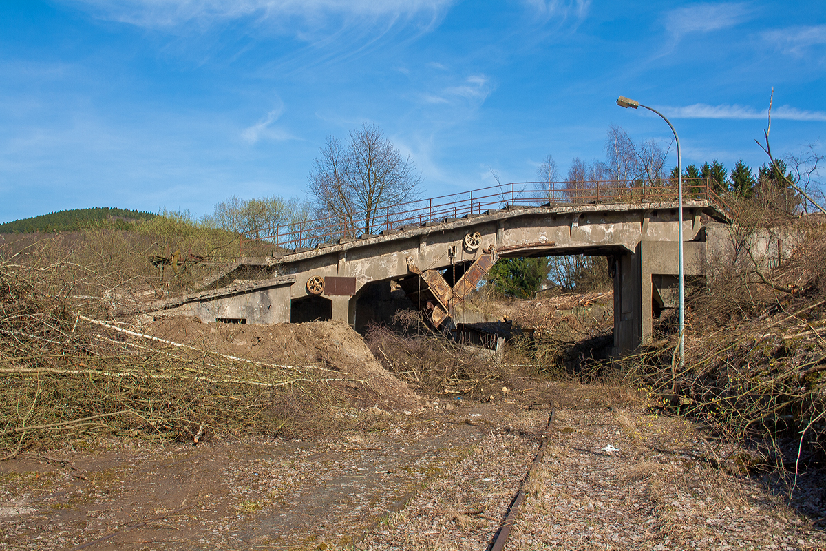 Die letzten Reste der Bremsbahn der Eiserfelder Steinwerke AG des Basaltbruches Mahlscheid (Mahlscheiderkopf). Die ehemalige Verladestation am 24.03.2011 (im gleichen Jahr angerissen) bei der alten Ziegelei in Herdorf.

Der ehemalige Steinbruch Mahlscheid (heute NSG) befindet sich im Westerwald an der Landesgrenze der Bundesländer Rheinland-Pfalz und Nordrhein-Westfalen im Bereich der Gemeinden Herdorf (Landkreis Altenkirchen) und Struthütten (Landkreis Siegen-Wittgenstein). Mitten durch den ehem. Steinbruch verläuft die Landesgrenze, so wurde der Bruch von zwei Firmen betrieben, zum einen auf der Herdorferseite (zu RLP) von der Firma Klein und zum anderen auf der Struthüttenerseite (zu NRW) von den Eiserfelder Steinwerke AG. Von beiden Brüchen führten Bremsbahnen hinab ist Tal. Die der Eiserfelder Steinwerke AG, war ca. 1,5 km lang und führte entlang der Landesgrenze nach hier hinab zur alten Ziegelei, wo das Gestein (Schotter) auf normalspurige Bahnwagen umgeladen wurde. Dafür führte vom Bahnhof Herdorf ein Anschlussgleis hinauf. 

Was ist eine Bremsbahn:
Eine Bremsbahn ist im Grunde eine Standseilbahn, aber ein sehr energiesparendes Konzept, zwei Wagen sind über ein Drahtseil verbunden, welches über eine Bremshaspel führt und kontrolliert abgebremst wird. Das zu fördernde Material wird mittels eines gebremsten Wagens hinabbefördert und der beladene schwererer Wagen zeiht somit den leeren Wagen wieder hinauf. Das Gewicht der zu Tal laufenden beladenen Wagen brachte einfach die dafür nötige Energie auf - also ein sehr energiesparendes Konzept.

Ob die Bremsbahn zwei parallel verlaufende Schienenstränge oder eine abtsche Weiche hatte, ist mir z.Z. nicht bekannt.
