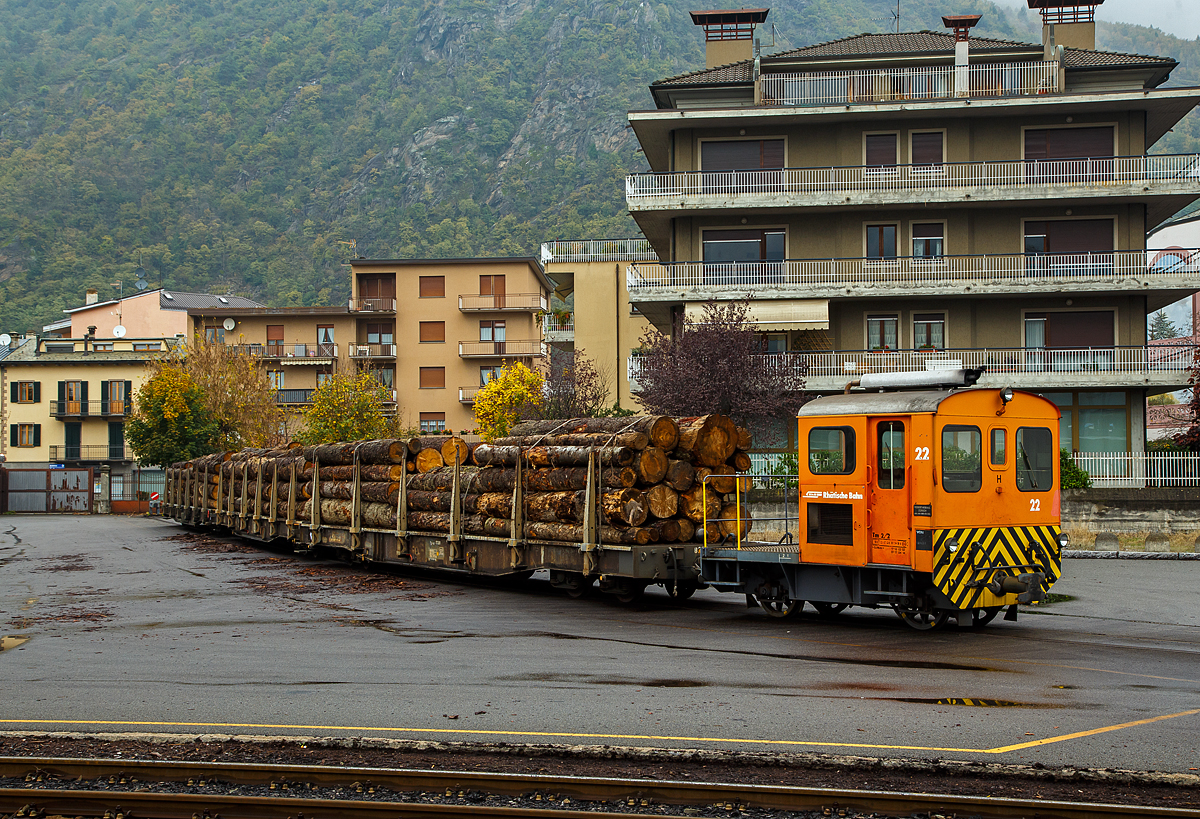 Die RhB Tm 2/2 22, ex RhB Tm 2/2 58, steht am 02.11.2019 mit drei angehangenen und mit Rundholz beladenen Flachwagen vom Typ “Sp-w“ der Serie 8271 – 8300 beim Bahnhof Tirano. 

Der Traktor vom Typ RACO 55 LA 4 wurde 1965 von RACO (Robert Aebi AG) unter der Fabriknummer 1717 gebaut. Im Jahr 1989 erfolgte die Remotorisierung mit einem Cummins Motor vom Typ 4BT 3.9 und die Umzeichnung in Tm 2/2 22.

Als Tm 2/2 werden diesel- oder benzinbetriebene Traktoren (Kleinlokomotiven) bezeichnet.
Die RhB besaß im Laufe der Jahre insgesamt 42 zweiachsige Traktoren mit Verbrennungsmotoren. Davon haben sechs eine Funkfernsteuerung und tragen deshalb die Bezeichnung Tmf 2/2. Die verbleibenden 36 Fahrzeuge teilen sich auf in 26 heute orange Rangierfahrzeuge und 10 heute gelbe Baudiensttraktoren. Insgesamt hatte die RhB 12 dieser baugleichen RACO 55 LA 4.

Zwischen 1957 und 1969 lieferte die Firma Robert Aebi (Raco) die dieselmechanischen Traktoren Tm 2/2 64–67, 62–63, 57–61 und schließlich noch Nummer 56. Die Nummerierung erfolgte vor den schon vorhandenen Tm 68 und 69. Basis für diese Fahrzeuge waren die Tm II der SBB. Der mechanische Aufbau wurde von RACO entwickelt und gebaut, der Dieselmotor war von Saurer-SLM. Die Kraftübertragung vom Motor auf die Achsen erfolgte mittels Kettenantrieb, dadurch sind diese Traktoren nur für den leichten Verschubdienst an Bahnhöfen geeignet. Bei einem Umbau in den Jahren 1989-90 wurden die Motoren von SLM durch solche von Cummins ausgetauscht, dabei wurden die Nummern auf 15 bis 26 geändert und die Traktoren dabei in die Ablieferungsreihenfolge gebracht. Die ursprünglich rotbraun, heute orange lackierten Fahrzeuge sind 5,06 m lang und 9 t schwer. Sie bestreiten den Rangierdienst auf Stationen mit kleinem bis mittlerem Güteraufkommen, wobei die meisten der 12 Traktoren ihrer jeweiligen «Heimatstation» fest zugeteilt sind.

TECHNISCHE DATEN:
Spurweite: 1.000 mm
Achsfolge: B
Länge über Puffer: 5.060 mm
Breite: 2.640 mm
Leergewicht: 9 t
Ladegewicht: 2 t
Höchstgeschwindigkeit: 30 km/h (55 km/h Schleppfahrt)
Motorbauart: 4-Zylinder-Dieselmotor
Motortyp: ab 1989/90 Cummins 4BT 3.9 (ursprünglich Saurer-SLM 4 VD 11)
Motorleistung: 62 kW (ursprünglich 44 kW)
Anfahrzugkraft: 30 kN (ursprünglich 25 kN)
Stundenzugkraft: 15 kN bei 10 km/h
Leistungsübertragung: Rollenkette

Die offenen, vierachsigen RhB Flachwagen mit Rungen vom Typ Sp-w der Serie 8271 – 8300 sind die Allrounder der Rhätischen Bahn schlechthin und werden vorwiegend für den Transport von Rundholz eingesetzt. An jeder Längsseite besitzen sie sechs Steckrungen.

TECHNISCHE DATEN vom Typ Sp-w (8271 bis 8300) :
Typenbezeichnung:  Sp-w
Wagennummern:  8271 bis 8300
Baujahr: 1979
Spurweite: 1.000 mm
Länge über Puffer: 16.540 mm 
Drehzapfenabstand: 11.000 mm 
Achsabstand im Drehgestell: 1.400 mm
Laufraddurchmesser: 750 mm (neu)
Breite über Alles: 2.700 mm
Ladelänge: 15.500 mm
Ladebreite:  2.310 mm
Rungenhöhe: 1.050 mm
Ladefläche: 34 m²
Eigengewicht:  ca. 15.600 kg
Ladegewicht:  33 Tonnen
Höhe ab Schienenoberkante: 965 mm