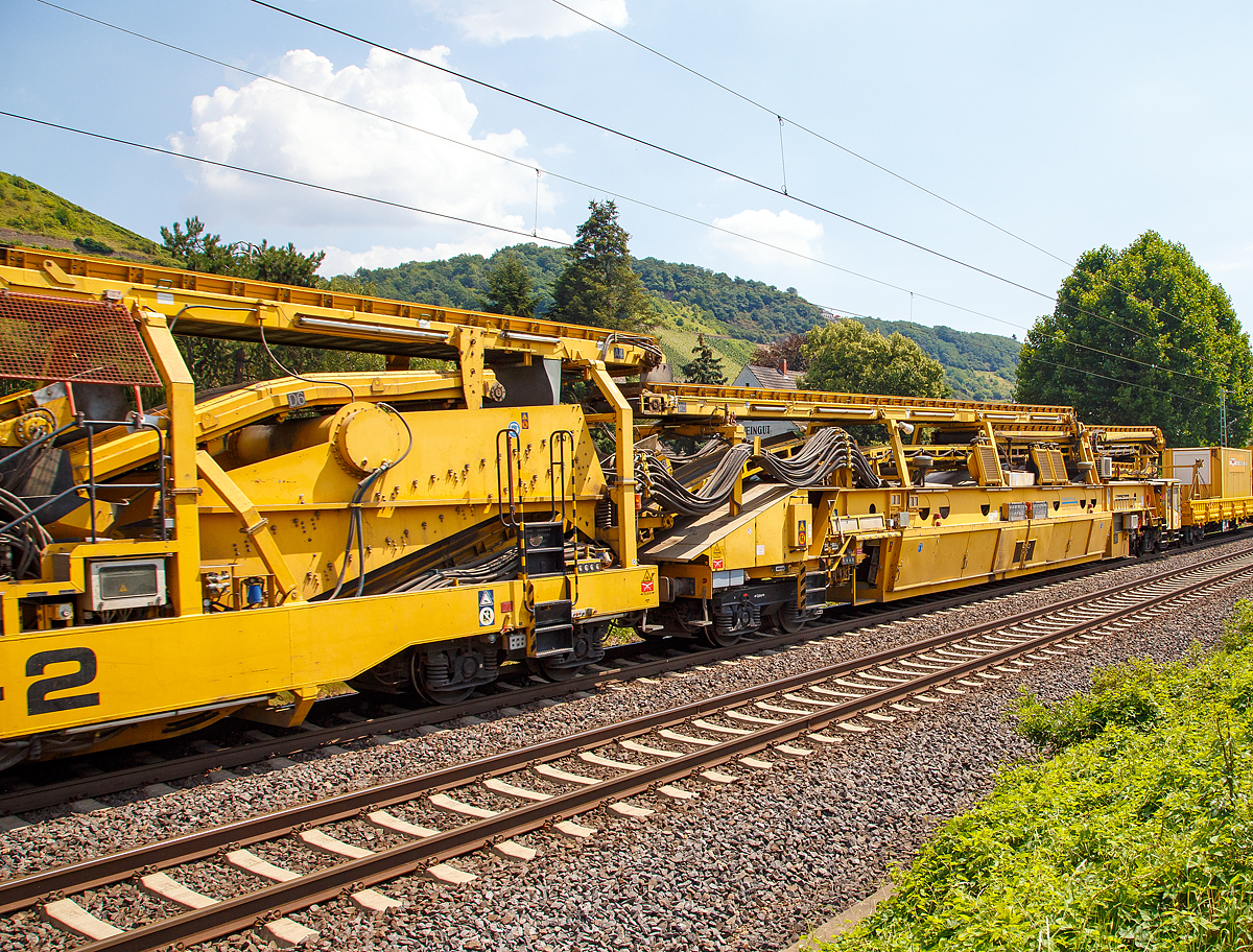 
Die Wiebe Recycling-Planumsverbesserungsmaschine mit Schotterrecycling RPMW 2002-2 am 14.07.2018 im Zugverband auf der Fahrt durch Leutesdorf,  auf der KBS 465 (Rechte Rheinstrecke) in Richtung Norden. 

Über 140 Meter lang, knapp 5 Meter hoch und gute 560 Tonnen schwer – die Gleisbaumaschine RPMW 2002-2 gehört zu den größten der Welt. Mit ihrer beachtlichen Leistung und dem umfänglichen Leistungsspektrum ist sie ein äußerst wichtiger Bestandteil des Maschinenparks der Unternehmensgruppe Wiebe.

Die Recycling Planumsverbesserungsmaschine führt verschiedene Gleisbauarbeiten durch – und das mit einer Motorengesamtleistung von über 2100 Kilowatt. Diese Kraft kommt bei Totalsanierungen zum Tragen, bei denen die RPMW 2002-2 mehrere Arbeitsschritte simultan ausführt: Die verschmutzte Schotterbettung wird ausgebaut, das abgetragene Bettungsmaterial aufbereitet, Schotter recycelt und die Unterbauplanumsschicht erneuert.

TECHNISCHE DATEN:
Hersteller: Plasser & Theurer
Baujahr, Erstzulassung: 2000
Spurweite: 1.435 mm
Anzahl der Achsen: 29, davon 12 angetrieben
Baumaschinennummer: Aushubmaschine 3369, Recyclingmaschine 3368, Antriebswagen 3367,  Stopf- u. Einschotterungsmaschine 3370
Motoren: Caterpillar 
Leistung: 2.860 PS
Gesamtlänge über Puffer: 140,90 m
Breite: 3,29 m
Höhe: 4,65 m
Gewicht: 560 t
V zul. im Zug eingestellt: 100 km/h
V max. bei Eigenfahrt: 20 km/h
Fahrradius: 120 m

Der große Unterschied zwischen Planumsverbesserungsmaschine und Bettungsreinigungsmaschinen besteht darin, dass die Planumsverbesserungsmaschine nicht nur den Schotter ausheben und recyceln kann, sondern auch einen Teil des Planums (Unterbau) ausheben (bis 1.200 mm unter SOK). Zudem kann die RPM vor der Neuschotterung (Recycling- mit Neumaterial) auch eine Planumsschutzschicht (PSS-Material) einbringen.
Der Neuschottern wird durch die Stopfeinrichtung 09-32 Stopfsatellit im Gleisbett verdichtet und das Gleis ist danach wieder mit 70 km/h befahrbar.

Hier im Bild ist der Anfang der Maschine (in Arbeitsrichtung), wo aber nicht der erste Arbeitsschritt beginnt, denn der beginnt an der Schotteraushubkette. Im Betrieb werden Materialförder- und Siloeinheit en (MFS) vor die Maschine gesetzt, zwei Förderbänder der Maschine ausgefahren und der Abraum in die MSF übergeben.