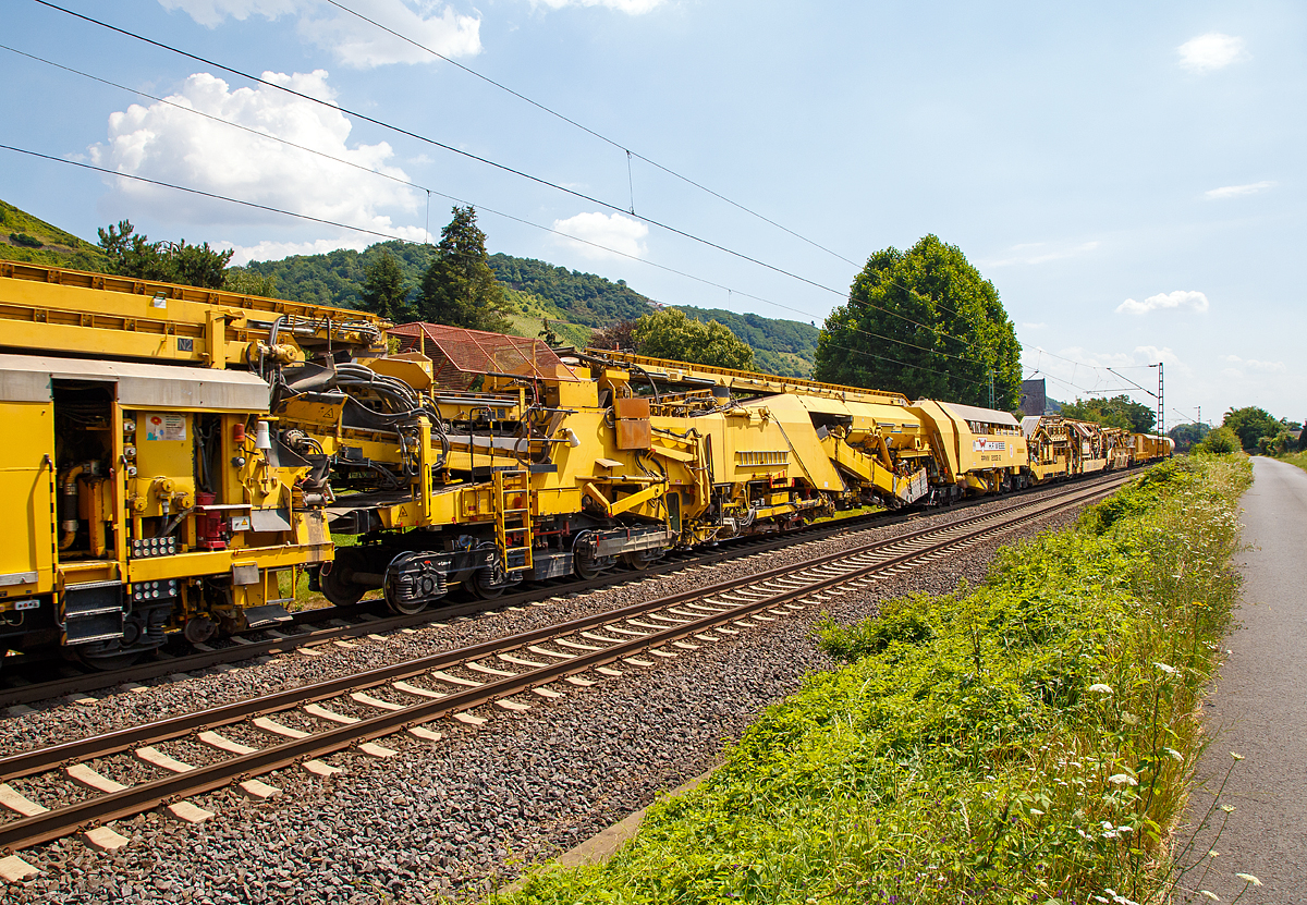 
Die Wiebe Recycling-Planumsverbesserungsmaschine mit Schotterrecycling RPMW 2002-2 am 14.07.2018 im Zugverband auf der Fahrt durch Leutesdorf,  auf der KBS 465 (Rechte Rheinstrecke) in Richtung Norden. 

Über 140 Meter lang, knapp 5 Meter hoch und gute 560 Tonnen schwer – die Gleisbaumaschine RPMW 2002-2 gehört zu den größten der Welt. Mit ihrer beachtlichen Leistung und dem umfänglichen Leistungsspektrum ist sie ein äußerst wichtiger Bestandteil des Maschinenparks der Unternehmensgruppe Wiebe.

Die Recycling Planumsverbesserungsmaschine führt verschiedene Gleisbauarbeiten durch – und das mit einer Motorengesamtleistung von über 2100 Kilowatt. Diese Kraft kommt bei Totalsanierungen zum Tragen, bei denen die RPMW 2002-2 mehrere Arbeitsschritte simultan ausführt: Die verschmutzte Schotterbettung wird ausgebaut, das abgetragene Bettungsmaterial aufbereitet, Schotter recycelt und die Unterbauplanumsschicht erneuert.

TECHNISCHE DATEN:
Hersteller: Plasser & Theurer
Baujahr, Erstzulassung: 2000
Spurweite: 1.435 mm
Anzahl der Achsen: 29, davon 12 angetrieben
Baumaschinennummer: Aushubmaschine 3369, Recyclingmaschine 3368, Antriebswagen 3367,  Stopf- u. Einschotterungsmaschine 3370
Motoren: Caterpillar 
Leistung: 2.860 PS
Gesamtlänge über Puffer: 140,90 m
Breite: 3,29 m
Höhe: 4,65 m
Gewicht: 560 t
V zul. im Zug eingestellt: 100 km/h
V max. bei Eigenfahrt: 20 km/h
Fahrradius: 120 m

Der große Unterschied zwischen Planumsverbesserungsmaschine und Bettungsreinigungsmaschinen besteht darin, dass die Planumsverbesserungsmaschine nicht nur den Schotter ausheben und recyceln kann, sondern auch einen Teil des Planums (Unterbau) ausheben (bis 1.200 mm unter SOK). Zudem kann die RPM vor der Neuschotterung (Recycling- mit Neumaterial) auch eine Planumsschutzschicht (PSS-Material) einbringen.
Der Neuschottern wird durch die Stopfeinrichtung 09-32 Stopfsatellit im Gleisbett verdichtet und das Gleis ist danach wieder mit 70 km/h befahrbar.

Hier in der Bildmitte die Planumsaushubkette:
Hat die Schotteraushubkette die Schotterschicht abgetragen, nimmt die Planumsaushubkette das verbleibende Boden- und Bettungsmaterial bis zum Erdplanum auf. Auch diese Aushubkette lässt sich stufenlos justieren, nämlich auf die gewünschte Räumbreite, Räumtiefe und Planumsquerneigung. Erneut transportieren die Förderanlagen den Aushub zur Maschinenfront, wo er auf Materialförder- und Siloeinheiten verladen wird.