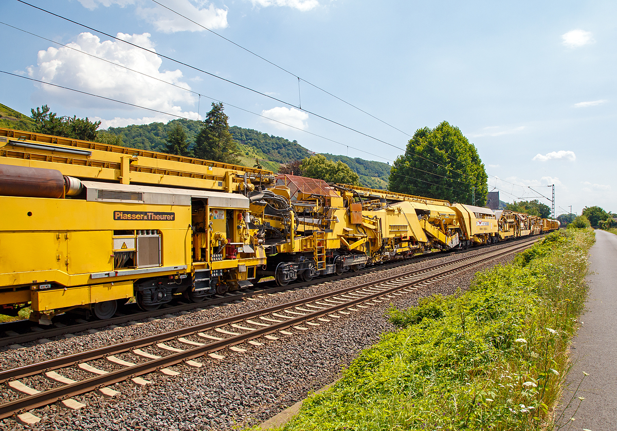 
Die Wiebe Recycling-Planumsverbesserungsmaschine mit Schotterrecycling RPMW 2002-2 am 14.07.2018 im Zugverband auf der Fahrt durch Leutesdorf,  auf der KBS 465 (Rechte Rheinstrecke) in Richtung Norden. 

Über 140 Meter lang, knapp 5 Meter hoch und gute 560 Tonnen schwer – die Gleisbaumaschine RPMW 2002-2 gehört zu den größten der Welt. Mit ihrer beachtlichen Leistung und dem umfänglichen Leistungsspektrum ist sie ein äußerst wichtiger Bestandteil des Maschinenparks der Unternehmensgruppe Wiebe.

Die Recycling Planumsverbesserungsmaschine führt verschiedene Gleisbauarbeiten durch – und das mit einer Motorengesamtleistung von über 2100 Kilowatt. Diese Kraft kommt bei Totalsanierungen zum Tragen, bei denen die RPMW 2002-2 mehrere Arbeitsschritte simultan ausführt: Die verschmutzte Schotterbettung wird ausgebaut, das abgetragene Bettungsmaterial aufbereitet, Schotter recycelt und die Unterbauplanumsschicht erneuert.

TECHNISCHE DATEN:
Hersteller: Plasser & Theurer
Baujahr, Erstzulassung: 2000
Spurweite: 1.435 mm
Anzahl der Achsen: 29, davon 12 angetrieben
Baumaschinennummer: Aushubmaschine 3369, Recyclingmaschine 3368, Antriebswagen 3367,  Stopf- u. Einschotterungsmaschine 3370
Motoren: Caterpillar 
Leistung: 2.860 PS
Gesamtlänge über Puffer: 140,90 m
Breite: 3,29 m
Höhe: 4,65 m
Gewicht: 560 t
V zul. im Zug eingestellt: 100 km/h
V max. bei Eigenfahrt: 20 km/h
Fahrradius: 120 m

Der große Unterschied zwischen Planumsverbesserungsmaschine und Bettungsreinigungsmaschinen besteht darin, dass die Planumsverbesserungsmaschine nicht nur den Schotter ausheben und recyceln kann, sondern auch einen Teil des Planums (Unterbau) ausheben (bis 1.200 mm unter SOK). Zudem kann die RPM vor der Neuschotterung (Recycling- mit Neumaterial) auch eine Planumsschutzschicht (PSS-Material) einbringen.
Der Neuschottern wird durch die Stopfeinrichtung 09-32 Stopfsatellit im Gleisbett verdichtet und das Gleis ist danach wieder mit 70 km/h befahrbar.

Hier in der Bildmitte die Planumsaushubkette:
Hat die Schotteraushubkette die Schotterschicht abgetragen, nimmt die Planumsaushubkette das verbleibende Boden- und Bettungsmaterial bis zum Erdplanum auf. Auch diese Aushubkette lässt sich stufenlos justieren, nämlich auf die gewünschte Räumbreite, Räumtiefe und Planumsquerneigung. Erneut transportieren die Förderanlagen den Aushub zur Maschinenfront, wo er auf Materialförder- und Siloeinheiten verladen wird.