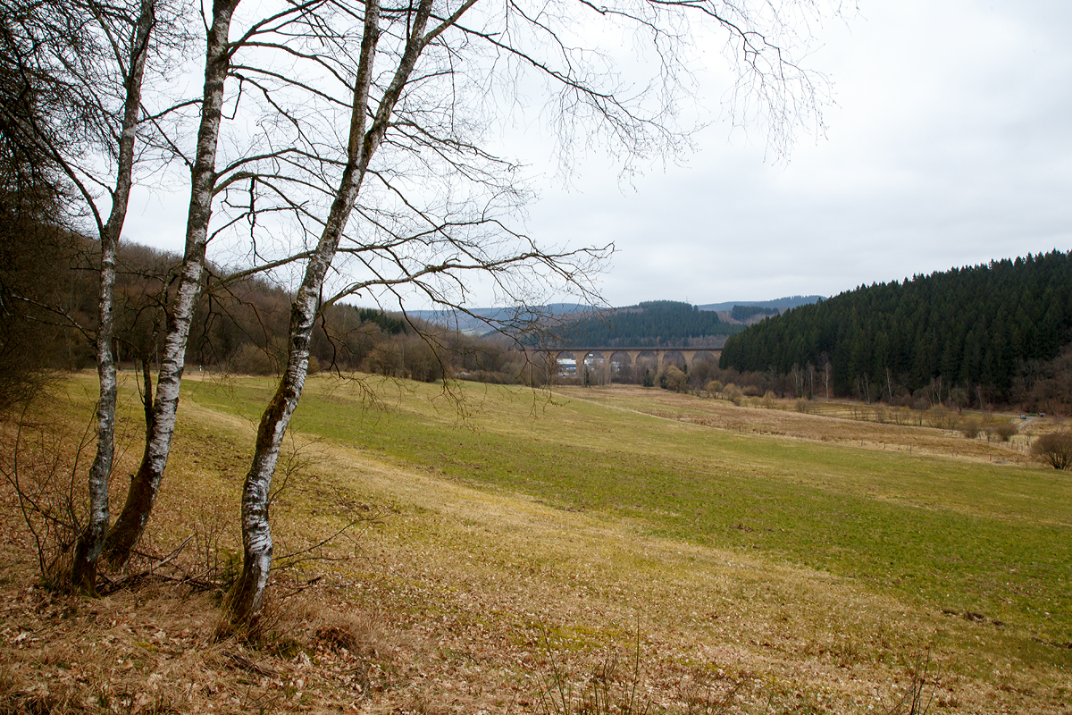 
Ein anderer Blick auf den Rudersdorfer Viadukt am 19.03.2016. 

Der Rudersdorfer Viadukt ist eines der drei Ingenieur-Großbauwerke im nördlichen Abschnitt der Dillstrecke (KBS 445) zwischen Siegen und Haiger auf dem Gebiet des heutigen Ortsteils Rudersdorf der Gemeinde Wilnsdorf, im Bereich von Streckenkilometer 114,9. Aufgrund der schwierigen Topografie und der begrenzten technischen Möglichkeiten war eine direkte Verbindung zwischen Siegen, Haiger und darüber hinaus Dillenburg zum Zeitpunkt des Baus der Deutz-Gießener Bahn vom heutigen Köln-Deutz nach Gießen beim Bau dieser Strecke in den 1850er-Jahren noch nicht möglich. Erst 1915 wurde diese direkte Verbindung zwischen Siegen und Haiger fertiggestellt. Das war vor allem für den aus dem Ruhrgebiet nach Süden führenden Kohleverkehr wichtig. Möglich wurde diese Streckenführung durch die drei großen Ingenieurbauwerke: Den Niederdielfener Viadukt, den Rudersdorfer Viadukt und den Rudersdorfer Tunnel. 

Bei diesem trüben Wetter war mit dieser Blende so kein Bild mit Zug möglich, so muss ich wohl an diese etwas höhere Fotostelle noch mal bei besserem Licht hin...