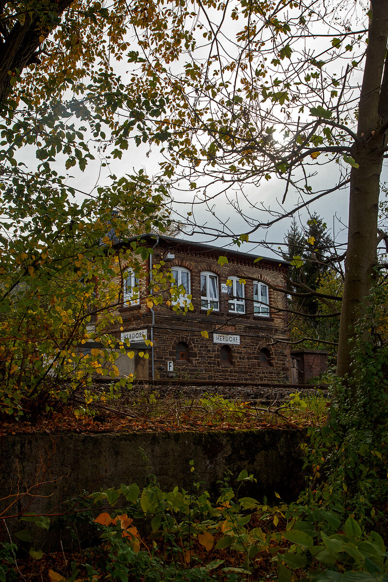 Ein etwas anderer Blick auf das1901 gebaute mechanische Weichenwärter Stellwerk Herdorf Ost (Ho), an der Bahnstrecke Betzdorf - Haiger (KBS 462 „Hellertalbahn“), hier am 03.11.2022.

Ja, in Herdorf gibt es immer noch den Luxus von zwei in Betrieb befindlichen Stellwerken das Stellwerk Herdorf Fahrdienstleiter (Hf) und das hier zusende Weichenwärter Stellwerk Herdorf Ost (Ho). Sie liegen in Sichtweite ca. 600 m entfernt, Hf beim Bahnhof und hier Ho in der Nähe zum Abzweig zur Anschlussstelle KSW (ex Freien Grunder Eisenbahn). Bis in die 1960-Jahre waren die Aufgaben des Weichenwärters noch sehr umfangreicher. Die Strecke war noch eine zweigleisige Hauptstrecke. Ursprüngliche Planungen sahen sogar vor, sie im Rahmen der Elektrifizierung der Siegstrecke ebenfalls zu elektrifizieren. Diese Erwägungen wurden aber leider nicht weiter verfolgt. Zudem gab es noch Anschlussstellen zur Herdorfer Friedrichs Hütte und zu den Eiserfelder Steinwerken AG.

Da die Stellwerkstechnik in Herdorf noch rein mechanisch ist, werden beide noch benötigt, bzw. ein Umbau auf ein Stellwerk ist wohl zu aufwendig.