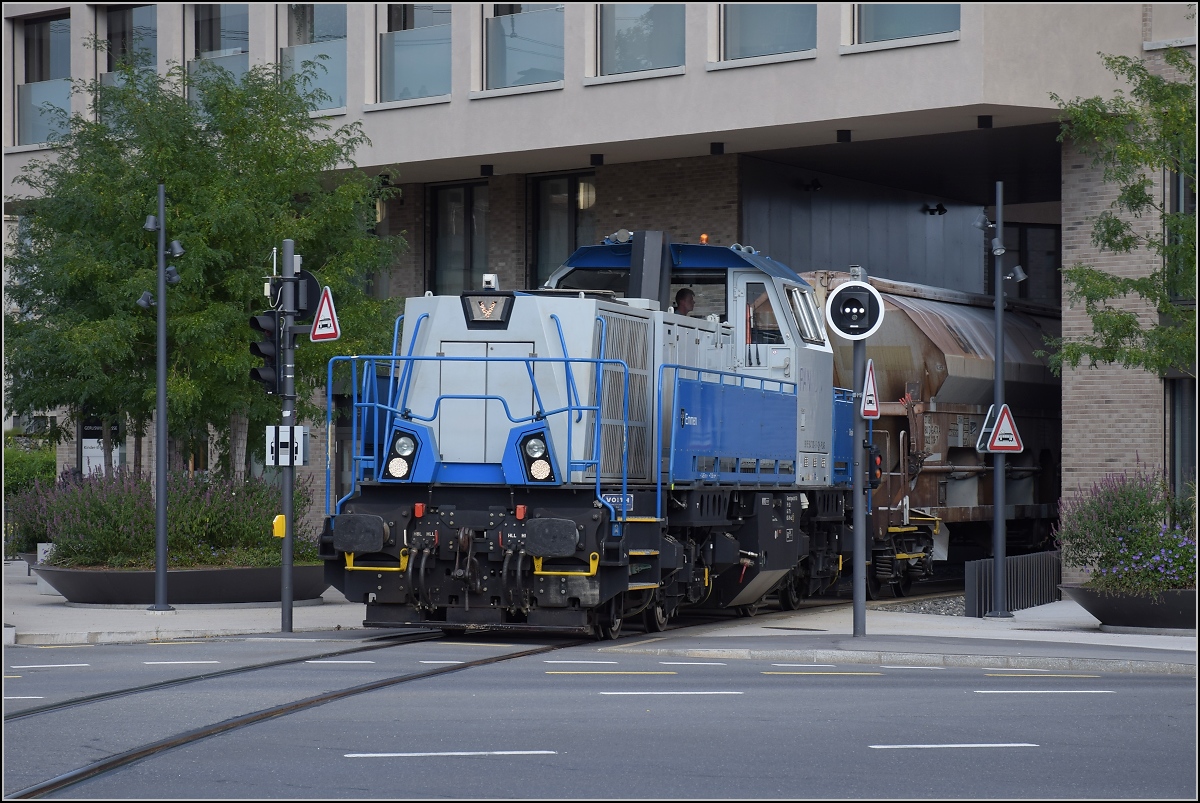 Gravita Am 847 003 'Littau' schiebt einen schweren Stahlzug von der Emmenwaid durch das Eckhaus in den Bahnhof Emmenbrücke. Das kantige Design der Gravita passt zum modernen Eckhaus. Und die Dieselabgase wahrscheinlich auch durch die Isolierfensterfugen, wenn man 5 Minuten das Haus zudieselt... August 2021. 