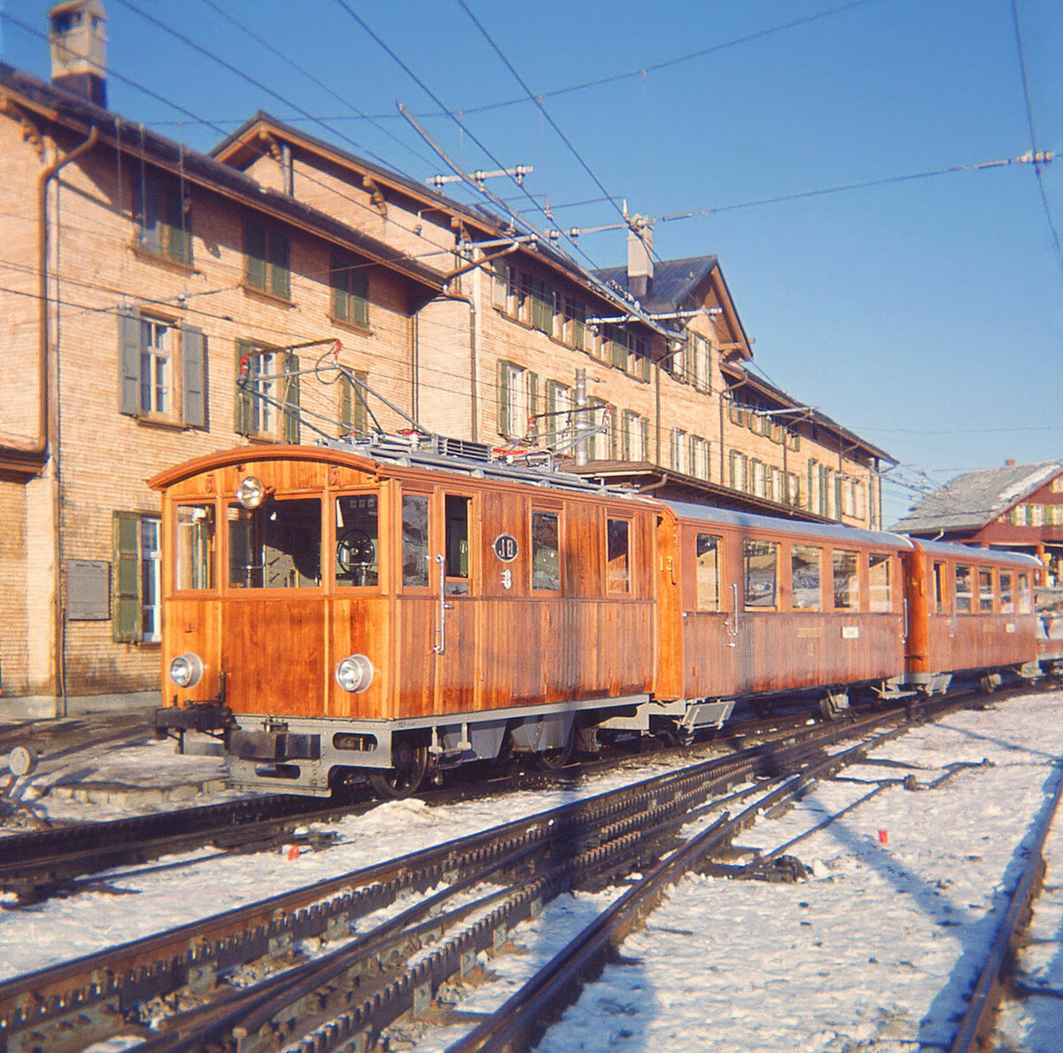 Lokomotive 8 der Jungfraubahn: Mit den Wagen 13 und 14 auf der Kleinen Scheidegg, Januar 1964. Diese beiden Wagen waren die ersten, die nicht mehr in der Coupé-Bauweise, sondern mit Mittelgang und Endtüren gebaut wurden (1911). Wagen 14 wurde 1970 ausrangiert, Wagen 13 als Touristikwagen für den Eiger Ambassador Express hergerichtet (1993/4). Heute ist Wagen 13 im World Nature Forum in Naters (Wallis), wo eine virtuelle Reise aufs Jungfraujoch von der Südseite her geplant (oder bereits möglich?) ist.  