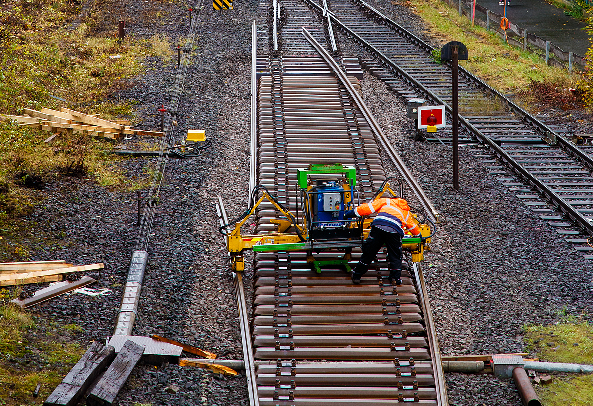 
Mittels einer hydraulischen Schienenumsetzmaschine vom Typ Giesmar MPRM 1032 werden am 15.10.2020 in Herdorf die letzten Meter Schienen auf die Schwellen gesetzt.

Die Schienenumsetzmaschine ist eine selbstangetriebene hydraulisch angetriebene Einheit zum Verlegen und Entfernen von langgeschweißten Schienen mit einem Bediener. Das Gerät stützt sich auf den Schwellen ab, die Schienen werden aufgenommen und können dann bis zu 500 mm angehoben werden. Nun erfolgt die seitliche Verschiebung und die Schienen werden auf die richtige Position auf der Schwelle abgelegt. Das Gerät ist geeignet für Scheinen mit einem Metergewicht von 37 bis 70 kg, die max. Hubkraft beträgt 4.500 kg. Es ist zudem möglich einen hydraulischen Schienenzieher ATR 6 anzuschließen. Das Eigengewicht von dem Gerät beträgt ca. 1.065 kg. 

Der hydraulische Antrieb erfolgt mittels einer HATZ-Hydraulikpumpen-Einheit (Hatz-Außenzahnradpumpe und Dieselmotor). Die Pumpe wird angetrieben von einem HATZ luftgekühltem Einzylinder-4-Takt Dieselmotor mit Direkteinspritzung und horizontale Kurbelwelle vom Typ 1D42C. 
