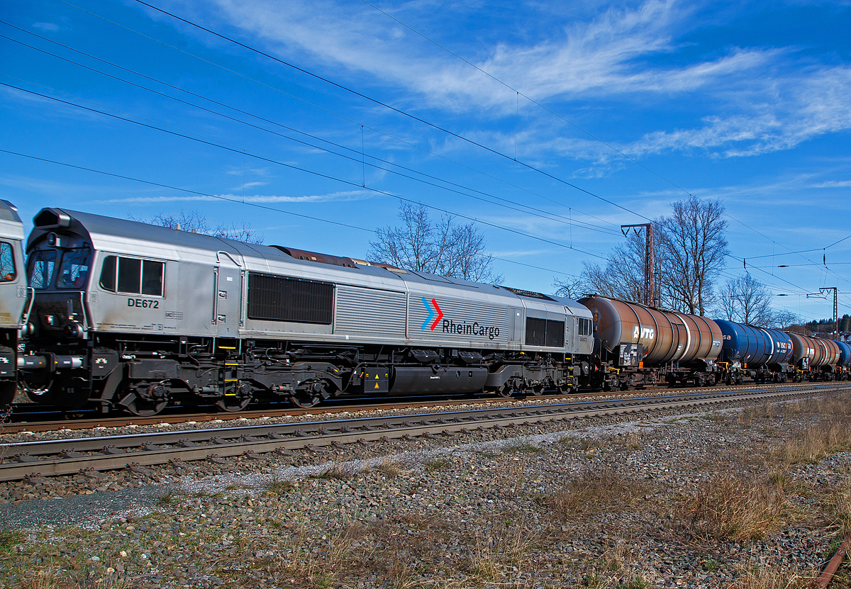 Nochmals im Detail...
Die RheinCargo DE 672 (92 80 1266 072-8 D-RHC), ex HGK DE 172, u.a. geschleppt von der RHC 2056 bzw. 185 588-1 (91 80 6185 588-1 D-RHC, die am 20.03.2021mit den beiden Class 66 (DE 670 und DE 672) und einem Kesselwagenzug, durch Rudersdorf (Kr. Siegen) über die Dillstrecke (KBS 445) in nördlicher Richtung fährt.

Die Lok wurde 2003 von EMD (Electro-Motive Division eine Tochter von General Motors) unter der Fabriknummer  20028453-5 gebaut, Eigentümer und Vermieter ist die Beacon Rail Leasing Ltd in London.

Die Lok ist eine EMD JT42CWR (auch bekannt als Class 66). Diese sind diesel-elektrische 6-achsige Schwerlastlokomotive. Sie besitzt einen 12 Zylinder 2-Takt-Turbodieselmotor vom Typ 12N-710G3B-EC, der einen Generator vom Typ EM AR8/CA6 antreibt der wiederum den Strom für die 6 Gleichstrommotoren vom Typ D43TR erzeugt welche die 6 Achsen angetrieben. Die Lokomotive wird von einem Board-Computer (EM 2000) überwacht und verfügt über verschiedene Mess- und Diagnosefunktionen. Die Lokomotive hat Zulassungen für Deutschland und Belgien.

Die JT42 CWR basiert auf der Entwicklung der 70er Jahre. Die Lokomotive erweist sich als eine grundsolide Baureihe, die dank dem einfachen Design und den Gleichstromantriebsmotoren einen zuverlässigen Posten in jeder Flotte darstellt. Die dreiachsigen HTCR-E Drehgestelle verfügen über gegenläufig radialgelenkte Endachsen, die Mittelachse ist seitenverschiebbar, diese ermöglichen den Betrieb dieser 6-achsigen-Lokomotive auf Strecken die in der Regel auf 4-achsige Lokomotiven eingeschränkt sind (Kleinster befahrbarer Radius 80 m). Die seitlichen Schiene-Kräfte sind dadurch auch gesenkt.
 
TECHNISCHE DATEN: 
Achsfolge: Co`Co`
Spurweite: 1.435 mm
Länge über Puffer: 21.349 mm
Drehzapfenabstand: 14.140 mm 
Breite: 2.692 mm
Höhe: 3.912 mm
Gewicht: 126 t
Dieselmotorleistung:  2.462 kW (ca. 3.200 PS)
Motorbauart:  V 12-Zylinder-2-Takt-Turbodieselmotor 
Motortyp:  12N-710G3B-EC
Drehzahl: 235 – 904 U/min
Tankinhalt: 6.400 l
Generator: AR8/CA6 
Fahrmotoren: 6 Stück D43TRC (DC / Gleichstom)
Leistung an den Rädern: 2.268 kW / 3.072 PS
Höchstgeschwindigkeit: 120 km/h
Anfahrzugskraft: 400 kN