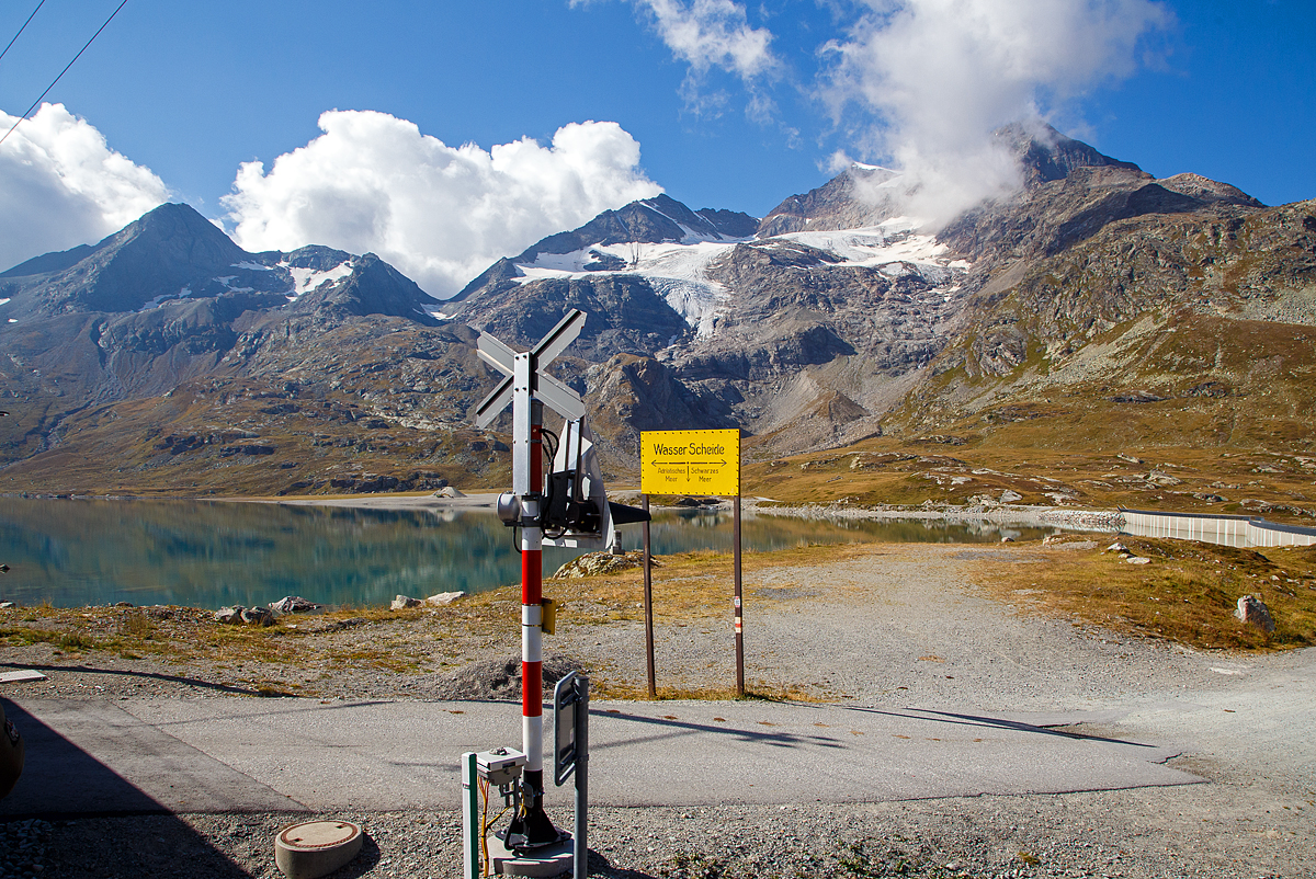 Nun erreichen wir am 06.09.2021den Lago Bianco auf einer Höhe von 2.223 Metern über Meer. 

Hier oben bei der Staumauer befindet sich auch zugleich die Wasserscheide zwischen Donau und Po. In Richtung Süden (Tirano) fließ das Wasser in den Po und somit ins Mittelmeer, in Richtung Norden (St. Moritz) fließ das Wasser über den Inn in die Donau und somit ins Schwarze Meer.

Der Lago Bianco ist ein Stausee am Berninapass zwischen dem Valposchiavo und dem obersten Seitental des Engadins, dem Val Bernina, in der Schweiz. Er liegt damit auf der Grenze zwischen den Bernina- (westlich) und Livigno-Alpen (östlich). Früher bestanden im Gebiet des heutigen Stausees zwei natürlichen Seen, der größere Lago Bianco, , und der kleinere südlich anschließende Lago della Scala. In den Lago Bianco mündeten mehrere kleine Bergbäche von den Höhen der Umgebung. Die beiden Gewichtsstaumauern Scala (Südseite) und Arlas (Nordseite) wurden zwischen 1910–1911 errichtet, so dass sich ein Stausee mit einem Volumen von 18,6 Mio. m³ bildete.

Unmittelbar am Nordende des Lago Bianco liegt die kontinentale Wasserscheide zwischen den Einzugsgebieten des Po und des Inn-Donau-Flusssystems. Wenige Meter nördlich des Lago Bianco liegt der Lago Nero (Schwarzsee) am Oberlauf des Berninabaches, dem folgt dann der kleinere Lago Pitschen (Pitschensee).
