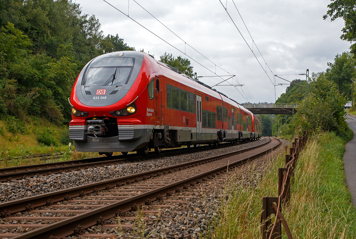 Vermutlich auf einer Überführungsfahrt, wobei der Zugzielanzeiger Kraków Główny (Krakau Hauptbahnhof) zeigt, was ich nicht ganz glaube....
Zweigekuppelte dreiteilige PESA LINK III – 633 048 / 933 048 / 633 548 und 633 542 / 933 042 / 633 042 der DB Regio Bayern fahren am 26.08.2021 bei Wissen (Sieg) über die Siegstrecke (KBS 460) in Richtung Siegen.

Die PESA LINK III wurden 2019 von PESA - Pojazdy Szynowe PESA Bydgoszcz SA in Bydgoszcz (deutsch Bromberg) gebaut,
vorne der 633 048 ff unter der Fabriknummer A643BNA085 und der hintere 633 042 ff unter der Fabriknummer A643BNA079.

Eigentlich war für Dezember 2017 schon der Einsatz im Dieselnetz Allgäu geplant, aber die Triebzüge passten nicht ins deutsche Lichtraumprofil, sie waren wenige Millimeter zu breit  und so gab es keine Zulassung. Der polnische Hersteller PESA musste die Züge umkonstruieren. Danach gab es weitere Probleme, die Fahrzeuge entsprachen nicht den bestellten technischen Anforderungen hinsichtlich des Gewichtes und des Antriebes, so musste PESA erneut eine Umkonstruktion an dem Fahrzeugmodell vornehmen. Am 30. Mai 2018 hat das Eisenbahnbundesamt EBA die Zulassung für den Einsatz der zweiteiligen Züge vom Typ Pesa Link II (BR 632) für die DB Regio nun erteilt. Für die dreiteiligen Pesa Link III (BR 633) wurde sie mittlerweile auch erteilt. 

Warum es aber solange braucht um Normen und Lastenhefte zu lesen entzieht sich meiner Kenntnis. 

Der PESA LINK (Projektname DMU 120) ist ein Dieseltriebwagen des polnischen Herstellers PESA (Pojazdy Szynowe Pesa Bydgoszcz SA). Die ČD (Tschechische Bahnen) vermarkten sie als „RegioShark“ (RegioHai). Hai war auch mein erster Eindruck, im September 2014 auf der InnoTrans 2014 in Berlin, als das erste Vorserienfahrzeug 631 001-4 vorgestellt wurde.

Es werden verschiedene Varianten von ein- bis vierteiligen Triebzügen, mit unterschiedlichen Motorleitungen, angeboten.

Der Innenraum des Pesa Link ist im Mittelteil in Niederflurbauweise ausgeführt, während die Fahrgastbereiche an den Fahrzeugenden hochflurig ausgelegt sind. Die Bodenhöhe des Niederflurbereichs beträgt in der DB-Version im 600 mm. Je ein Motor treibt jeweils beide Achsen eines Drehgestells (Enddrehgestell) am Fahrzeugende an. Zwischen den Endwagenteilen und dem mittleren Wagenteil befinden sich jeweils nicht angetriebene Jakobsdrehgestelle. 

Der Antrieb erfolgt diesel-hydromechanisch durch 2 Stück MTU 12 Zylinder, 4-Takt Dieselmotor (PowerPack) mit Abgasturbolader und Ladeluftkühlung vom Typ 12V 1600 R70LP mit einer Leistung von 625 kW, über ein 6-Gang-Automatik-Getriebe ZF EcoLife Rail (480 kW), jeweils auf die beide Achsen eines Enddrehgestelles

Technische Daten der BR 633 (DB):
Spurweite: 1.435 mm (Normalspur)
Achsformel: B’(2’)(2’)B’
Länge über Puffer:  57.130 mm
Höhe: 4.206 mm
Breite: 2.800 mm
Drehzapfenabstand: 17.040 mm
Achsabstand im Drehgestell: 2.100 mm
Dienstgewicht: 120,4 t
Achslast: 18,9 t
Höchstgeschwindigkeit: 140 km/h
Installierte Leistung: 2 x 625 kW (2 x 838 PS)
Beschleunigung:  0,74 m/s²  bei 0-30 km/h
Antrieb: MTU Powerpack 12 Zylinder, 4-Takt-Dieselmotor mit Abgasturbolader und Ladeluftkühlung vom Typ MTU 6H 1800 R85L
Motornenndrehzahl: 2.100 U/min
Motorhubraum: 21  l
Getriebe: 6-Gang-ZF-Automatikgetriebe EcoLife Rail (480 kW),
Kraftübertragung: diesel-hydromech.  
Fußbodenhöhe (Niederflurber.):   600 mm                              
Fußbodenhöhe (Hochflurber.):   1.290 mm
Kleinster bef. Halbmesser: 100 m (Werkstatt) / 150 m (Betrieb)
Kupplungstyp:  Scharfenberg Typ 10
Sitzplätze in der 1. Klasse: 12
Sitzplätze in der 2. Klasse: 94 und 54 Klappsitze
Fahrradstellplätze: 36 (dann keine klappsitze)
Stehplätze: 196