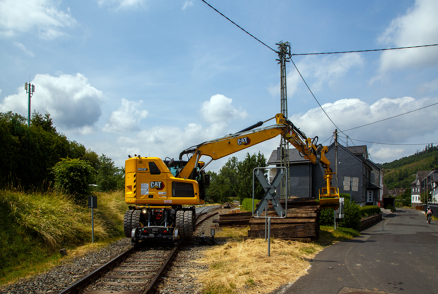 Bei dem Rangierbahnhof der KSW (Kreisbahn Siegen-Wittgenstein) in Herdorf der Betriebssttte FGE -Freien Grunder Eisenbahn (KSW NE447 / DB-Nr. 9275) wurden und wird der Unterbau der Gleise erneuert. Der Umbau erfolgt ohne groe Einschrnkungen des Tagesablaufes. 

Hier stapelt der Caterpillar CAT M323F Zweiwegebagger mit hydrostatischem Schienenradantrieb (Serien-Nr. RH600 189), Kleinwagen Nr. D-ZBM 99 80 9902 521-0 der ZEPPELIN Baumaschinen GmbH (Garching), wohl ein Mietbagger, am 26.06.2023 bei der Talbahnstrae Schellen.

Der Zweiwegebagger wurde 2022 unter der Fabrik-Nr. CAT M323FERH600189 gebaut.

Schienenradantrieb
Der CAT Zweiwegebagger mit hydrostatischem Schienenradantrieb (vom franzsischen Spezialmaschinenbauer UNAC) ist konsequent fr den Einsatz auf der Schiene entwickelt. Mit seinem kurzen Heck, dem innovativen Radantrieb und Bremssystem fr alle Gleisrder und dem ausgefeilten, aber einfach bedienbaren Kontrollsystem erschliet der Cat M323F den Anwendern entscheidende Vorteile.Anders als bei den bisher blichen Zweiwegebaggern bewegt sich die Maschine auf der Schiene damit nicht abgesenkt auf den herkmmlichen Rdern voran, sondern ohne Bodenkontakt auf den Schienenrdern selbst. Die hohe Bodenfreiheit gewhrleistet dabei, dass die Sicherheitseinrichtungen im Gleisbett beim Fahren nicht beschdigt werden. Mit dem Bremssystem im lbad an beiden Achsen und den Scheibenbremsen fr alle Gleisrder gewhrleistet der Cat M323F sicheren Vortrieb und kraftvolle Beschleunigung bis auf 20 km/h.

Klassische Zweiwegebagger sind vielfach noch mit Reibradantrieb ausgestattet. Die Reifen des Baggers werden dabei auf die Schienen oder Rolle gepresst und bertragen so die Antriebs- und Bremskrfte. Die Nachteile: hoher einseitiger Reifenverschlei und oft Beschdigungen von Sicherheitseinrichtungen im Gleisbett.

Kurzheckbauweise
Durch den kompakten Aufbau und die geringe Heckausladung von nur
1.566 mm kann der Schienenverkehr auf dem Nachbargleis problemlos
weiterlaufen. Auch mit dem optional verfgbaren Zusatzkontergewicht bleibt der kurze Heckschwenkradius unverndert. Trotz des kompakten Hecks bietet die Maschine mit dem robusten Verstellausleger auch auf dem Gleis viel Reichweite und hohes Hubvermgen.

Die Konstruktionsweise sowie das bis zu 7,5 t schwere Kontergewicht stellen dabei sicher, dass die Maschine dennoch ber eine hohe Standsicherheit, Reichweite und Hubvermgen verfgt.

Motor
Angetrieben wird der neue CAT Zweiwegebagger von einem Vierzylinder-Viertakt-Reihendieselmotor mit zwei Turboladern (Reihenturboaufladung) und Ladeluftkhlung (TTA) vom Typ CAT C4.4 ACERT TTA, Emissionen EPA Tier 4 Final (USA) bzw. Stufe V (EU) und Dieselpartikelfilter.

Motordaten:
Leistung: 129,4 kW (173 PS)
Maximales Drehmoment: 750 Nm bei 1400 U/min
Nenndrehzahl 2.200 U/min
Bohrung x Hub: 105 x 127 mm
Motorhubraum: 4,4 l
Verdichtungsverhltnis: 16,5 :1
Ansaugsystem: Turboladern und Ladeluftkhlung (TTA)
Verbrennungsverfahren: Direkteinspritzung
Abmessung: 845 x 742 x 868 mm
Gewicht (trocken) 420 kg

Der C4.4-Motor kann entweder mit extrem schwefelarmem Dieselkraftstoff oder mit B20-Biodiesel betrieben werden und erfllt die Emissionsnormen der EU-Stufe IV. Die Leerlaufabschaltung, die automatische Motordrehzahlregelung und das bedarfsgesteuerte Khlsystem verringern den Kraftstoffverbrauch.

TECHNISCHE DATEN:
Spurweite: 1.435 mm (Normalspur)
Eigengewicht: 23.400 kg
Hchstgeschwindigkeit: 19,9 km/h (20 km/h auf Strae)
Zul. Anhngelast: 220 t
Schienenbodenfreiheit: 195 mm
Straenbodenfreiheit: 360 mm
Zugkraft auf Strae: 104 kN
Zugkraft auf Schiene: 45 kN

Quellen: CAT, ZEPPELIN und Anschriften
