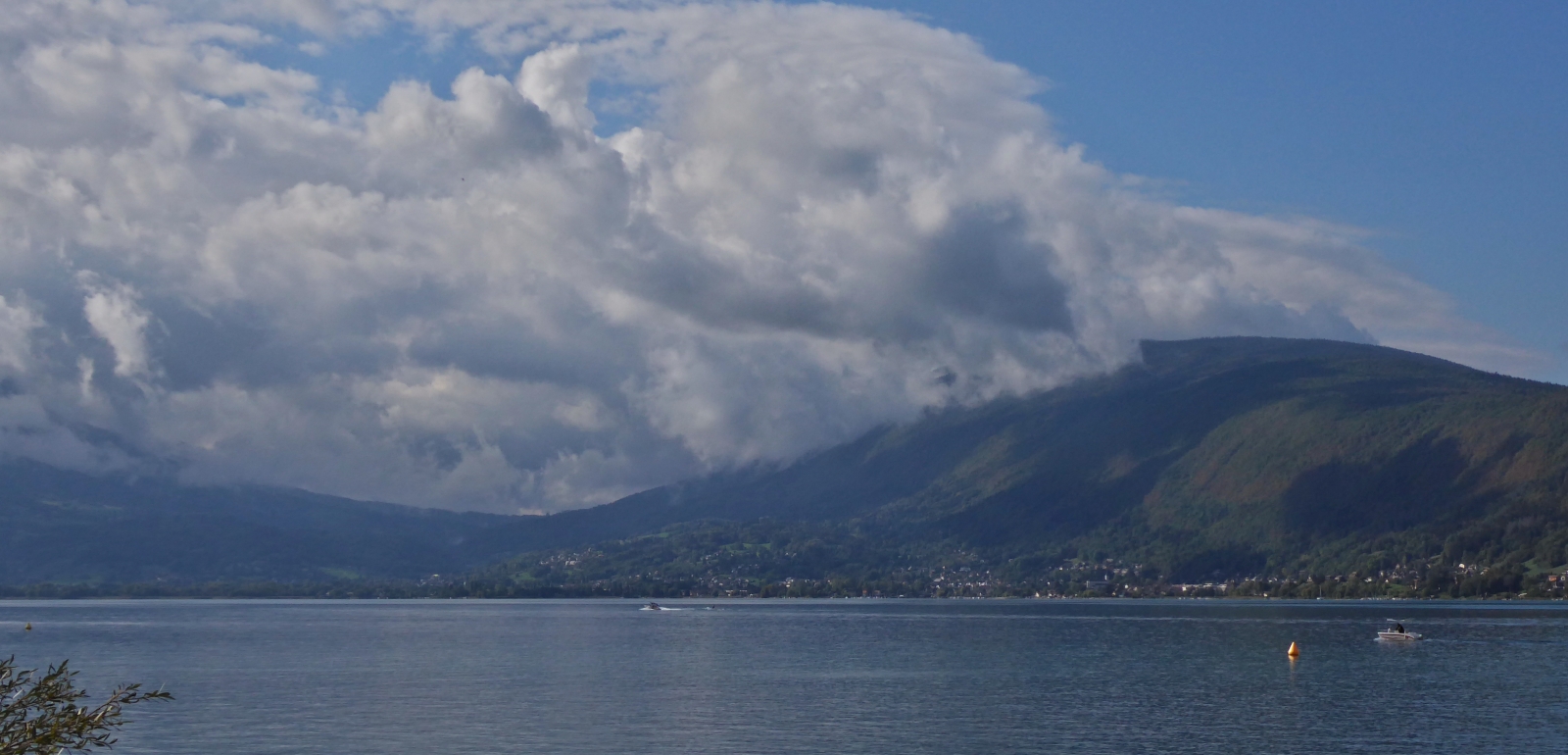 Blick über den See von Annecy auf das hügeliges Gelände und die tief hängenden Wolken an den Bergspitzen. 09.2022