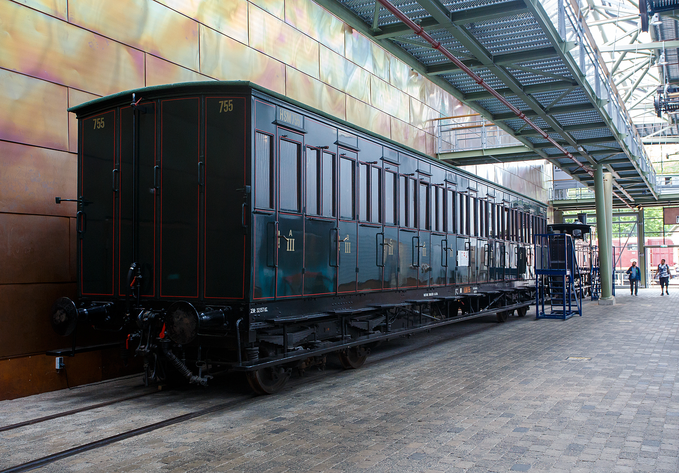 Der „viele Tren Wagen“ ein 3. Klasse Abteilwagen mit Seitentren ohne Durchgangsmglichkeit, HSM C 755 der damaligen HSM - Hollandsche IJzeren Spoorweg-Maatschappij (Hollndische Eisenbahn-Gesellschaft), ab 1922 NS C 5055, am 24. Juni 2025 im Het Spoorwegmuseum (bis 2005 NSM - Nederlands Spoorwegmuseum / Niederlndischen Eisenbahnmuseum) in Utrecht im ehemaligen Bahnhof Maliebaan.   

Ende des 19. Jahrhunderts hatten diese Wagen die Form eines langen, rechteckigen Kastens mit zahlreichen Tren an den Seiten, die Zugang zu den Sitzabteilen boten. Eine lange, auen angebrachte Stufe ermglichte dem Schaffner den bergang von einer Tr zur anderen. Die Sitzbereiche waren nur von auen zugnglich, einen Gang im Wageninneren gab es nicht. Anfang des 20. Jahrhunderts gab HSM 135 dieser Abteilwagen in Auftrag. Diese neue Wagengeneration war grer als die zuvor gebauten Wagen. Es gab 11 Abteile mit 10 Sitzpltzen fr 110 Personen. Dies brachte den Wagen den Spitznamen „Schafstall“ ein. Diese Wagen waren im ganzen Land bis in die 1950er Jahre im Einsatz, als neue Wagen und Triebwagen die veralteten Abteilwagen ersetzten.

Der Wagen vom Typ C11 (Serie 707 - 766 III) wurde 1907 von der Nederlandsche Fabriek van Werktuigen en Spoorwegmaterieel in Amsterdam (ab 1929 Werkspoor N.V.) gebaut und an die HSM geliefert.

Bedingt durch den Ersten Weltkrieg wurde 1917 eine Zweckgemeinschaft der unabhngigen Eisenbahngesellschaften HSM beziehungsweise HIJSM (Hollandsche IJzeren Spoorweg-Maatschappij) und SS (Maatschappij tot Exploitatie van Staatsspoorwegen) gegrndet. Die beiden Gesellschaften errichteten einen gemeinsamen Bahnbetrieb, blieben aber rechtlich unabhngig. Dies nderte sich 1938, als HIJSM und SS vollstndig fusionierten und in der AG NS (Nederlandse Spoorwegen, frher Nederlandsche Spoorwegen geschrieben) aufgingen. Das Rollmaterial wurde bereits 1921 zusammengelegt.

TECHNISCHE DATEN:
Spurweite: 1.435 mm (Normalspur)
Achsen: 4 (in 2 Drehgestellen)
Lnge ber Puffer: 18.300 mm
Leergewicht: 32.157 kg
Sitzpltze: 110 in der 3. Klasse in 11 Abteilen  10 Personen
Hchstgeschwindigkeit: 80 km/h