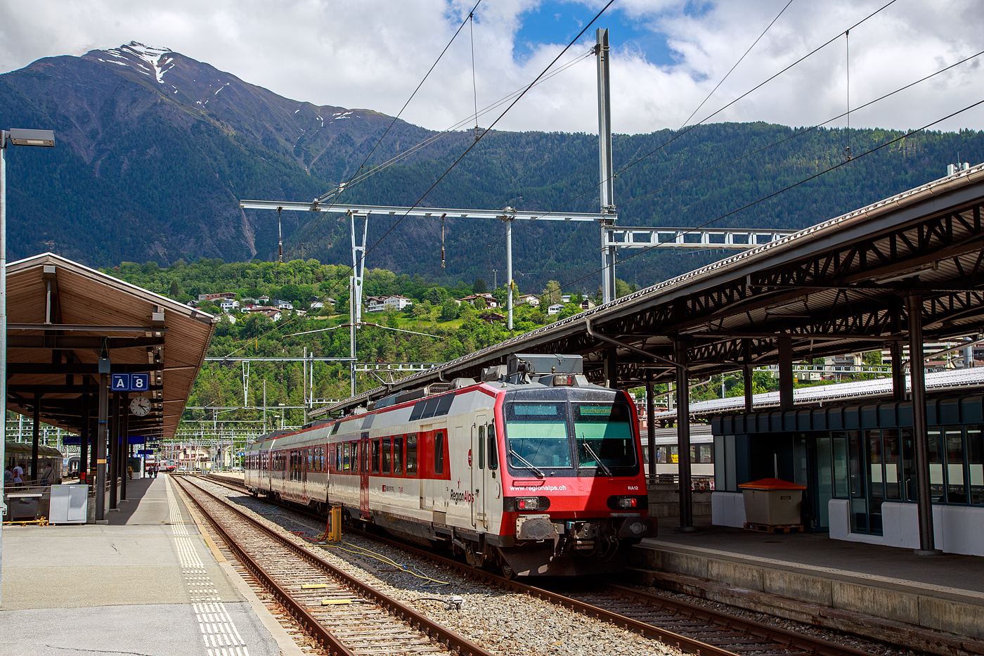 Der dreiteilige NPZ Domino RA12 der RegionAlps (ex SBB RBDe 4/4) hat am 25.05.2023 als Regio (St-Gingolph–St-Maurice –Martigny–Sion–Brig), Steuerwagen voraus, seinen Zielbahnhof Brig erreicht.

Der NPZ Domino besteht aus:
1./2. Klasse Steuerwagen ABt NPZ DO RA 50 85 39-43 948-1 CH-RA
Modernen 2.Klasse INOVA-Zwischenwagen mit Niederfluranteil B NPZ DO RA 50 85 29-43 407-0 CH-RA
und dem 
Triebwagen RBDe 560 DO RA 94 85 7 560 412-9 CH-RA, ex SBB RBDe 560 010-1 (Umbau 2009), hier rechts im Vordergrund.

Die Regionalps (RA) ist ein Eisenbahnverkehrsunternehmen im Kanton Wallis, mit Sitz in Martigny hat. Eigentümer derim Jahr 2003 gegründete Gesellschaft  sind die Schweizerischen Bundesbahnen (SBB) mit 70 %, die Transports de Martigny et Régions (TMR) mit 18 % und der Kanton Wallis mit 12 %. Die RA betreibt den Regionalverkehr vor allem im Rhonetal zwischen dem Ostufer des Genfersees und Brig. Inzwischen gehören Regionalps 16 dreiteilige NPZ Domino (Trieb-, Zwischen- und Steuerwagen ex SBB) und 4 RABe 525 NINA (ex TMR).

Als RBDe 4/4 wurden die Triebwagen der Schweizerischen Bundesbahnen (SBB) bezeichnet, die ab 1984 für die als Neuer Pendelzug (NPZ) bezeichneten Regionalzugskompositionen mit den dazugehörenden Steuerwagen angeschafft wurden. Sie tragen seit 1990 die Baureihenbezeichnung RBDe 560. Aus Kostengründen wurde damals auf die Beschaffung neuer Zwischenwagen verzichtet, verwendet werden stattdessen umgebaute Einheitswagen (EW I und EW II).

Die meisten von 1987 bis 1996 gebauten Fahrzeuge RBDe 560, 561 und 568 durchliefen 2008 bis 2013 ein Komplett-Modernisierungsprogramm. Aus aufgearbeiteten Trieb- und Steuerwagen sowie neu beschafften Zwischenwagen entstanden Regionalverkehrs-Kompositionen mit der Bezeichnung «Domino». Die Triebwagen werden dabei einheitlich als RBDe 560 (94 85 7 560 XXX-X) bezeichnet. Sie können in Vielfachsteuerung verkehren.

TECHNISCHE DATEN (Komposition RBDe 560, B und ABt) :
Spurweite:  1.435 mm (Normalspur)
Achsformel:  Bo’Bo’ +2´2´+2´2´
Länge über Puffer:  25.000 mm / 24.700 mm / 25.000 mm
Drehzapfenabstand: 17.600 mm / 18.900 mm /17.600 mm
Achsabstand im Drehgestell: 2.700 mm (ZW 2.500 mm)
Treib- und Laufraddurchmesser: 950 mm
Höhe:  3.750 mm
Breite:  2.860 mm
Dienstgewicht:  72 t (Triebwagen) + 36 t (ZW) + 38 t (Steuerwagen)
Höchstgeschwindigkeit: 140 km/h
Dauerleistung:  1.650 kW (2.250 PS)
Anfahrzugkraft:  182 kN
Dauerzugkraft: 78 kN
Anzahl Fahrmotoren: 4
Stromsystem:  Wechselstrom 15 kV 16,7 Hz
Sitzplätze: 54 (TW) / 60 (ZW) / 12+60 (SW) = 186 (12 in der 1. Klasse)
Ladegewicht: 0,3 t (Triebwagen)
Kupplungstyp: Schraubenkupplung