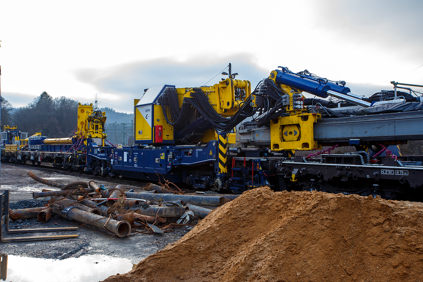 Der Gleisgründungszug der HERING Bahnbau GmbH (Burbach-Holzhausen) ist am 05 Februar 2026 auf den WEBA-Gleisen in Scheuerfeld/Sieg abgestellt. Hier das 8-achsigen gleisgebundenen Trägergerät (Baujahr 2023 durch TECHNE KIROW GmbH in Leipzig unter Fabriknummer MT 2020 171031), D-HGUI 99 80 9410 012-5, Gewicht 108.000 kg, LüP 15.000 mm.

Die Höchstgeschwindigkeit beträgt 100 km/h geschleppt, bei Eigenfahrt 5 km/h. 