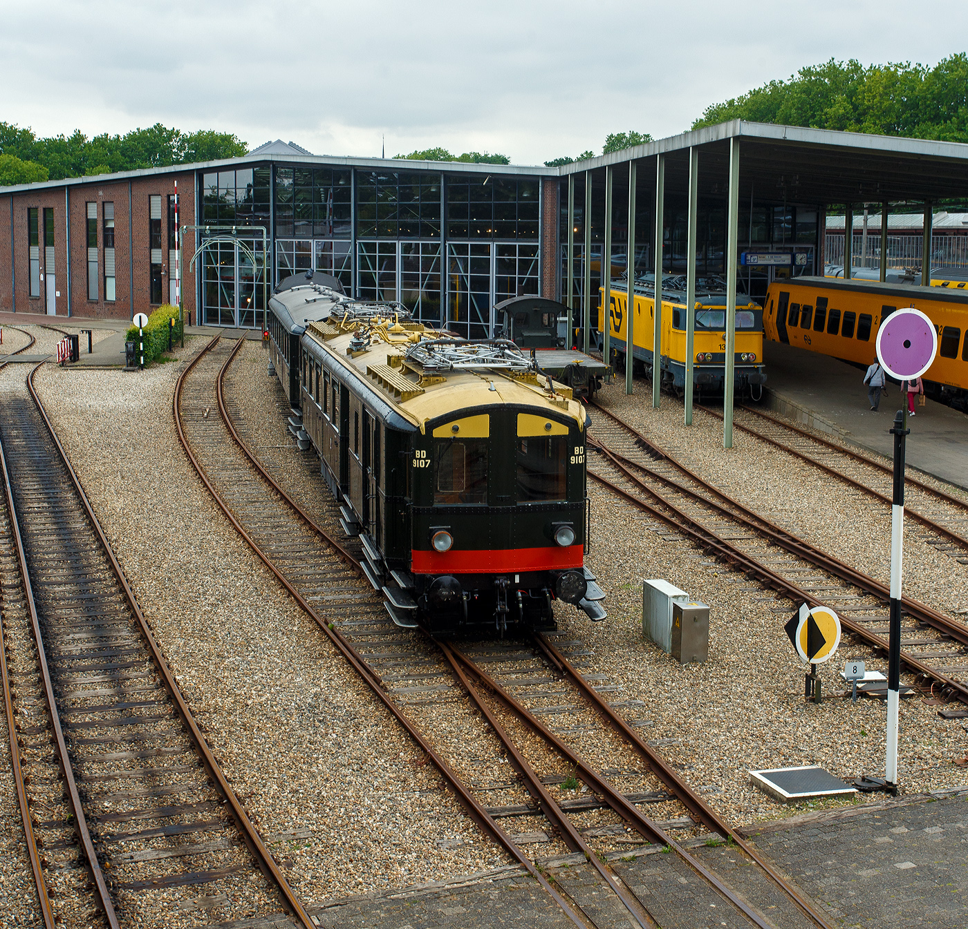 Der NS Mat ’24-Triebwagenzug (BD 9107, C 8553 und C 8104) „Blokkendozen“ (Kastendose) am 24 Juni 2025 im Het Spoorwegmuseum (bis 2005 NSM - Nederlands Spoorwegmuseum / Niederländischen Eisenbahnmuseum) in Utrecht im ehemaligen Bahnhof Maliebaanstation. Ein Eisenbahnmuseum das zum Verweilen einlädt. Hier im Vordergrund der Steuerwagen NS C 8104 (Ces) mit 88 Sitzplätzen der 3. Klasse und Durchgangsmöglichkeit, ex Triebwagen NS C 9411 (mCv).

Die NS-Baureihe Mat ’24 oder Materieel ’24 war eine (die erste) Serie von Elektrotriebzügen, die von der NS - Nederlandse Spoorwegen (Niederländischen Staatsbahnen, heute Niederländische Eisenbahnen AG) ab 1924 in großer Zahl eingesetzt wurde. Diese Züge sind unglaublich robust und schwer. nd der Tatsache, dass die Trainer wie Bausteine zusammengestellt werden können. Im Volksmund erhielten sie wegen des eckigen Äußeren und der Tatsache, dass die Wagen wie Bausteine zusammengestellt werden konnten, den Spitznamen „Blokkendozen“ (Kastendose). Ein weiterer Spitzname war „buffermaterieel“, weil sie im Unterschied zu anderen, mehr windschlüpfig aussehenden elektrischen Triebzügen mit üblicher Schraubenkupplung versehen waren. Wegen der Verbindung über Schraubenkupplung mit zwei Puffern konnten die Einheiten sehr flexibel kombiniert werden. Meist bestand ein Zug aus zwei Triebwagen und zwei oder drei antriebslosen Mittelwagen. Die lauten Geräusche der Motoren und Antriebe erinnerten manche Fahrgäste an Staubsauger, so dass auch dieser weitere Spitzname  Staubsauger  verwendet wurde. 

Ab Mitte der 1950er Jahre wurden die Mat ’24 zunehmend durch die neue Baureihe Mat ’54 ersetzt. Bei einigen Triebwagen wurden die Stromabnehmer und Motoren demontiert, sie wurden als einfache Beiwagen weiterverwendet. Da die Mat ’24 sehr robust waren, wurden einige Einheiten später auch als Postwagen oder für Dienstzwecke eingesetzt. Mehrere Wagen blieben museal erhalten.

Der Steuerwagen C 8104:
Der Steuerwagen C 8104 (Ces) wurde ursprünglich als Elektrotriebwagen C 9411 (mCv) 1928 bei NV Werkspoor in Zuilen mit einer elektrischen Installation von Heemaf in Hengelo gebaut. Er verfügte über 88 Sitzplätze der 3. Klasse und war als Spitzenverstärkung für die Hauptstrecke Amsterdam – Rotterdam vorgesehen. Durch einen Brand schwer beschädigt, wurde er 1944 zur Reparatur an Werkspoor gegeben, das inzwischen Teil der Gemeinde Utrecht geworden war. Erst nach dem Krieg im Jahr 1946 wurde C 9411 wieder in Dienst gestellt.

Der C 9411 war 1956 der erste Mat ’24-Triebwagen (Blokkendozen- Motorwagen) der in einen gezogenen Personenwagen, für den Einsatz hinter Elektrolokomotiven, umgebaut wurde und hauptsächlich als Spitzenverstärkung auf längeren Strecken innerhalb der Niederlande dienen sollte. Es erhielt daraufhin die Nummer B 5841 (Bz), wobei die 88 Sitzplätze auf Holzbänken unverändert blieben. Eine Einschränkung des Einsatzes war das Fehlen einer Toilette.

Aufgrund der Verfügbarkeit neuer und besserer Ausrüstung wurde der nunmehrige B 5841 im Jahr 1973 überflüssig. Anschließend wurde er zum Ausstellungswagen 99-31 003 umgebaut. Als solcher wurde er bis 1982 verwendet und dann für Museumszwecke reserviert.

Im Jahr 1983 begann man mit einer behutsamen Restaurierung, bei der zunächst die Innenausstattung mit Bänken und Türen eines zuvor abgerissenen „Blokkendozen“-Wagens (Kastendose-Wagens) wiederhergestellt wurde. Er erhielt erneut 88 Sitzplätze auf Holzbänken. Auch der voll ausgestattete Steuerstand wurde umgebaut. In den Jahren 1987 – 1989 erfolgte eine Generalüberholung und erhielt nun die Nummer C 8104 (Ces), da er nun mit den ursprünglichen Steuerwagen C 8101 – 8103 (Ces) identisch war. Der einzige Unterschied zwischen mCv und Ces besteht im Fehlen von Fahrmotoren und der dazugehörigen Elektroinstallation beim Ces.

Abkürzungen:
C = 3. Klasse
e = elektrischer Zwischenwagen
m = Triebwagen
s = ausgestattet mit Steuerstand
v = ausgestattet mit Steuerstand mit Balgdurchgang
z = ohne Toilette

Der dreiteilige Zug von Mat’24 des Niederländischen Eisenbahnmuseums, bestehend aus BD 9107, C 8553 und C 8104, war aufgrund einer Überholung des C 8104 und dem Fehlen der seit dem 1. April 2009 vorgeschriebenen automatischen Zugbeeinflussung ATB vorübergehend außer Betrieb. Die Überholung der Drehgestelle des C 8104 fand 2009 statt. Der Einbau der vereinfachten Version der ATB (ATBe) und deren Abnahme erfolgten im Mai und Juni 2010 bei Strukton in Zutphen. Im September wurde die Einsatzbescheinigung ausgestellt, danach fand am 9. Oktober wieder die erste Fahrt für ehrenamtliche Helfer des Eisenbahnmuseums statt.

Aufgrund größerer Wartungsarbeiten ist der Kastendosenzug aber z.Z. vorübergehend außer Betrieb.

TECHNISCHE DATEN:
Hersteller:	Werkspoor NV, Zuilen
Baujahr:1928
Typ:	Mat'24 ursprünglich '28 mC / seit 1989 Ces, Serie C 8101 – 8103 (8104)
Historischen Nummer:	ab 1928 - C 9411 / ab 1956 - B 5841 / ab 1973 - 99-31 003 / seit 1989 - C 8104
Spurweite:	1.435 mm (Normalspur)
Achsfolge:	2'2' (4 Achsen in zwei Drehgestellen)
Gewicht: 39 t
Länge über die Puffer:	19.800 mm
Höchstgeschwindigkeit: 120 km/h
Kupplung: Schraubenkupplung (UIC-Kupplung)
Betriebsfähigkeit: ja

