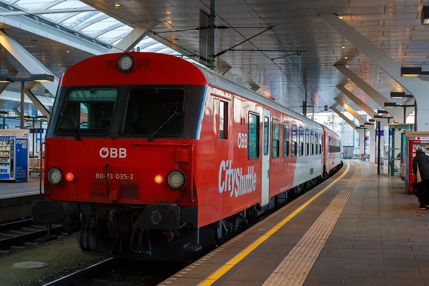 Der ÖBB REX 21 (REX 5873) von Salzburg Taxham Europark über Salzburg Hbf und Neumarkt am Wallersee nach Braunau am Inn, verlässt am 13 Januar 2025 den Hauptbahnhof Salzburg. Hier am Zugschluss der 2.Klasse ÖBB Inlandsreisezug-Steuerwagen (CityShuttle-Wagen) A-ÖBB 50 81 80-73 035-2 der Gattung Bmpz-s. 

Als Inlandsreisezugwagen der ÖBB (offiziell Inlandsreisezugwagen Typ neue Generation) wird eine Bauart von Reisezugwagen der ÖBB bezeichnet, die in den Jahren 1980 bis 1989, von den Herstellern SGP Graz und Jenbacher Werke, gebaut und von den 1990er-Jahren bis circa 2006 zu den bekannten CityShuttle-Wagen umgebaut wurden.

Entstehung der Steuerwagen:
Mitte der 1990er Jahre begann in den TS-Werken Floridsdorf und St. Pölten der Umbau in Wendezugwagen, bei dem 152 Zwischenwagen zu Steuerwagen (Bmpz-s) umgebaut worden sind. 

TECHNISCHE DATEN: 
Spurweite: 1.435 mm (Normalspur)
Länge über Puffer: 26 400 mm
Drehzapfenabstand: 18.300 mm
Achsstand im Drehgestell: 2.500 mm
Laufraddurchmesser: 840 mm (neu)
Höhe über SOK: 3.700 mm
Leergewicht: ca. 40 t
Höchstgeschwindigkeit: 160 km/h
Sitzplätze (in der 2. Klasse): 44 und 21 Klappsitze
Fahrradstellplätze: 7
Toiletten: 1
Bremse: O-PR-A
Zugelassen in: A, CH, D und H (MAV)