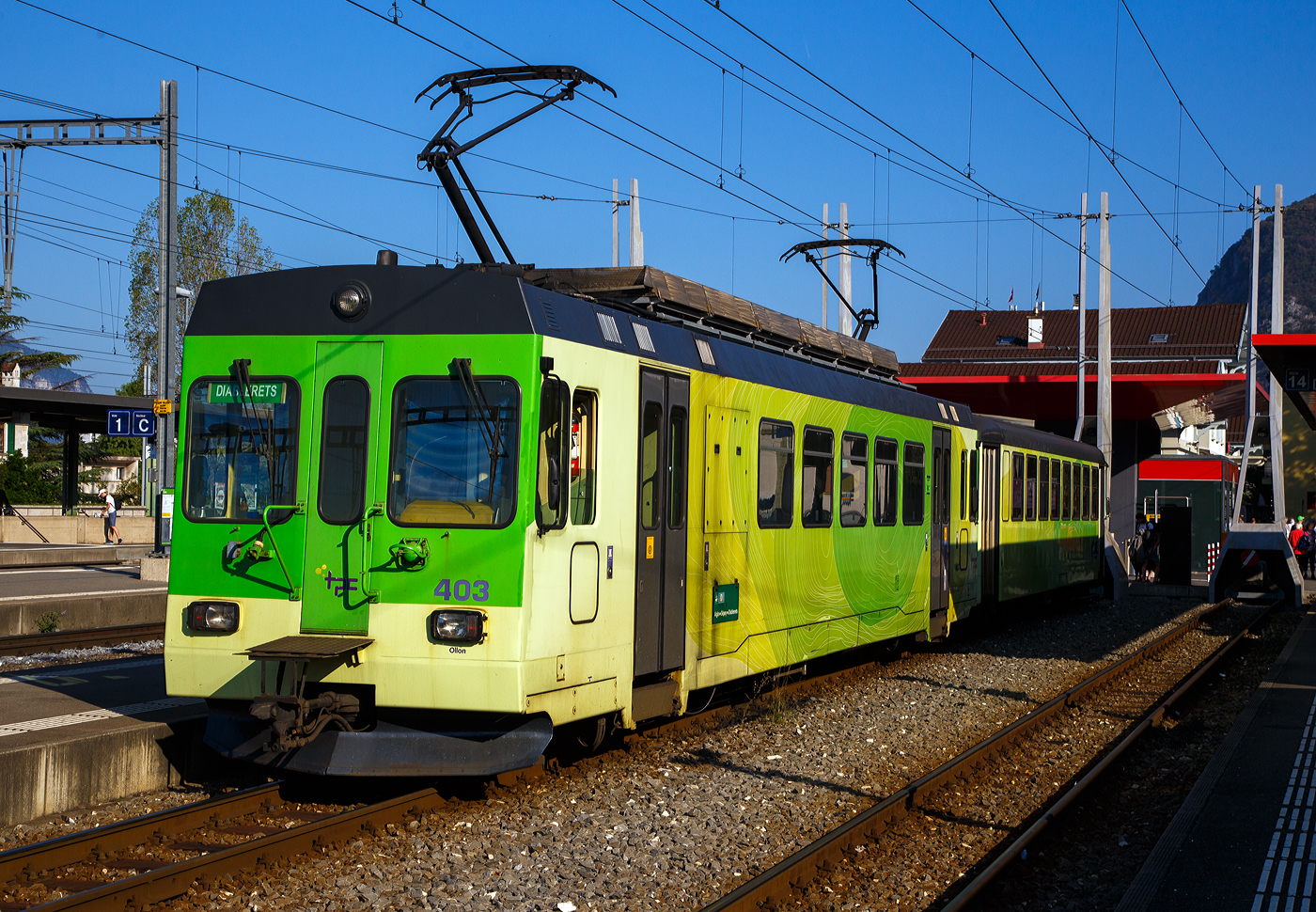 Der Triebwagen tpc ASD BDe 4/4 403 „Ollon” mit dem Steuerwagen tpc ASD Bt 431 haben am 10 September 2023, als ASD (Aigle–Sépey–Diablerets) Regionalzug R 24 von Les Diablerets via Le Sépey, nun den Bahnhof Aigle erreicht. Die 23,3 Kilometer lange Strecke der ASD (Aigle–Sépey–Diablerets) ist eine reine Adhäsionsbahn und führt von Aigle über Le Sépey nach Les Diablerets.

Der elektrische Personen-Triebwagen mit Gepäckabteil wurde 1987 von Vevey ACMV (Ateliers de constructions mécaniques de Vevey) in Vevey gebaut, die elektrische Ausrüstung ist von der BBC (Brown, Boveri & Cie.). Er ist ein sogenannter ACMV Westschweizer Meterspurtriebwagen der zweiten Generation. 

Die Westschweizer Meterspurtriebwagen sind elektrische Triebwagen, die 1985 bis 1992 von den Ateliers de constructions mécaniques de Vevey ACMV und 1996 von Vevey Technologies an sechs Westschweizer Privatbahnen für verschiedene Stromsysteme und zum Teil mit gemischtem Adhäsions- und Zahnradantrieb geliefert wurden. Die Fahrzeugfamilie ist modular aufgebaut und ließ sich bezüglich ihrer Größe und Ausstattung an die Erfordernisse der jeweiligen Bahngesellschaft anpassen. Die Triebwagen wurden elf Jahre produziert und während dieser Zeit der technischen Entwicklung angepasst.

Die Fahrzeuge sind in leichter Stahlbauart konstruiert und 2,65 Meter breit. Die Schürzen, der Unterteil des Kastens, wurden aus Aluminium-Stangpressprofilen hergestellt, die nach einer Kollision mit Kraftfahrzeugen ausgewechselt werden können. An den Stirnwänden wurden bei weniger beanspruchten Elementen Formteile aus glasfaserverstärktem Kunststoff verwendet. Die Wagenkästen der Triebwagen sind für die Aufnahme der elektrischen Ausrüstung verstärkt und mit Befestigungspunkten versehen. Für die Laufdrehgestelle wurde eine Bauart übernommen, die schon bei Steuerwagen der Chemin de fer Bière–Apples–Morges und Chemin de fer Yverdon–Ste-Croix verwendet wurde. Die Triebdrehgestelle verfügen über einen Rolldrehkranz und zwei längs angeordnete Fahrmotoren, die je eine Achse über Kardanwellen antreiben.

Neben einer Rekuperations- und einer Widerstandsbremse sind die Triebwagen mit einer selbsttätigen Druckluftbremse ausgerüstet. Weil deren Hauptleitung durch die Elektronik gesteuert wird, kann der Zug einhändig mit dem Fahrschalter bedient werden.

Die Aigle–Sépey–Diablerets-Bahn (ASD), seit 1999 Teil der Transports Publics du Chablais (TPC), konnten 1987 neues Rollmaterial beschaffen, so auch vier dieser Triebwagen BDe 4/4 (401 bis 404). Wegen ihrer engen Kurven dienten die kurzen NStCM-Triebwagen als Basisfahrzeug. Als Steuerwagen dienen der ASD Fahrzeuge der ehemaligen Birsigthalbahn, die sie von der Baselland Transport (BLT) erworben werden konnte. Für den Einsatz auf der ASD wurde der Führerstand, bei den ex BTB-Steuerwagen neu aufgebaut.

Auch die AOMC (Aigle-Ollon-Monthey-Champéry-Bahn) hat drei solcher Triebwagen (BDeh 4/4 501 bis 503) beschafft, diese waren aber durch den Zahnradbetrieb und das andere Stromsystem der AOMC doch anders ausgeführt, u.a. auch in besonderer Leichtbauweise. Um die technischen Normalien ihrer Strecken zu vereinheitlichen, bauten die TPC im Jahr 2016 die Linie von Aigle nach Champéry um. Sie ersetzten das bisherige Zahnstangensystem Strub durch eine Abt-Zahnstange und erhöhten die Fahrleitungsspannung auf 1500 Volt. Damit verloren diese BDeh 4/4 501–503 und die zugehörigen Steuerwagen ihr Einsatzgebiet.

TECHNISCHE DATEN:
Baujahr: 1987 (4 Stück)
Spurweite: 1.000 mm
Achsformel: Bo’Bo’
Wagenkastenmaterial: Stahl
Länge über Puffer:18.800 mm
Breite: 2.650 mm
Gewicht: 32,4 t
Höchstgeschwindigkeit: 65 km/h (ursprünglich 25 km/h)
Leistung: 820 kW
Stromsystem: 1500 Volt DC (Gleichstrom)
Elektrische Ausrüstung: Schützensteuerung
Sitzplätze: 32
Kupplungstyp: BSi -Kompaktkupplung 

Die BSI-Kompaktkupplung ist eine mechanische Vorrichtung zum Verbinden zweier Schienenfahrzeuge zu einem Zug. Sie überträgt die Zug- und Druckkräfte innerhalb eines Zugverbandes und lässt sich automatisch kuppeln und entkuppeln. Sie findet überwiegend bei Straßenbahnwagen und Regionaltriebwagen der Eisenbahn Verwendung. Die Kupplung wurde vom ehemaligen Unternehmen Bergische Stahl-Industrie-Gesellschaft in Remscheid entwickelt, inzwischen Teil der Wabtec-Gruppe.


Der Steuerwagen tpc ASD Bt 431,  ex BTB/BLT (Bt 26):
Die Geschichte:
Anlässlich der Modernisierung des BTB-Rollmaterials und für die Bildung von die Betriebsabwicklung stark vereinfachenden Pendelzügen wurden 1966 auch sieben Steuerwagen Bt 21 bis 27 beschafft. Diese standen jedoch lediglich sechs neuen Triebwagen ABe 4/4 11 bis 16 gegenüber. Der zusätzliche Steuerwagen wurde ab 1977 für einen Pendelzug mit den entsprechend angepassten Be 4/4 der Serie 8 bis 9 aus dem Jahre 1951 benötigt.

Die Steuerwagen entsprachen bezüglich des wagenbaulichen Teils so weit als möglich den Motorwagen. Es waren zwei Fahrgastabteile (Raucher/Nichtraucher) vorhanden. Auf der führerstandslosen Seite befanden sich die Plattformen mit den beidseitigen, pneumatisch betätigten Falttüren ganz am Wagenende, um im Wageninnern möglichst viele Sitzplätze anordnen zu können. Als Drehgestelle kamen solche elastischer Bauart mit Flexicoil-Lagerung und Gummi-Zusatzfedern sowie Klotzbremse zum Einbau.

Der Führerstand entsprach jenem der Motorwagen (ABe 4/4). Er war von Anfang an so ausgelegt, dass auch die entsprechend angepassten Be 4/4 8 und 9 ferngesteuert werden konnten. Eine Stirnwandtüre ermöglichte das Mitführen von Zusatzwagen oder das Einreihen eines Steuerwagens in der Zugsmitte. 1972 wurde der Zugfunk nachgerüstet.

Mit der Fusion der Basler Vorortsbahnen 1974 gingen alle sieben Steuerwagen, welche immer Seite Rodersdorf an die Züge gestellt wurden, an die neugegründete Baselland Transport AG (BLT) über ,so wurde dieser zum BLT Bt 26.

Nach der Betriebsumstellung im Herbst 1984 verkaufte die BLT alle sieben Fahrzeuge in die Westschweiz. Die Bt 22, 23, 24 und 25 kamen als Bt 132, 133, 134 und 131 zur Schmalspurbahn Aigle–Ollon–Monthey–Champéry (AOMC).

Die Bt 21 sowie 26 und 27 fanden den Weg zur Aigle–Sépey–Diablerets-Bahn (ASD). Ab September 1985 wurden sie bei ACMV in Vevey für den Betrieb mit den für 1987 bestellten Triebwagen BDe 4/4 401 bis 404 hergerichtet. Die Anpassungen umfassten im Wesentlichen:
• Neuanstrich
• Verschließen der vorderen Stirnwandtüren
• Einbau eines neuen Führertisches
• Anpassungen an den Steuerstromkreisen
• Anpassungen der elektrischen, pneumatischen und mechanischen Kupplungen (BSi)
• Einbau von Schienenbremsmagneten in beide Drehgestelle

Die Inbetriebsetzung erfolgte ab Juni 1987 als Bt 431 bis 433.

TECHNISCCHE DATEN bei Inbetriebsetzung (1966):
Spurweite: 1.000 mm
Typenbezeichnung: Bt
Anzahl Wagen: 7
Länge über alles: 17.212 mm
Größte Breite: 2.500 mm
Höhe über Dach: 3.450 mm
Drehzapfenabstand: 11.000 mm
Achsabstand im Drehgestell: 1.800 mm
Eigengewicht: 17.000 kg
Sitz-/Stehplätze: 64 / 66 (zusätzlich 2 Klappsitze)
Höchstgeschwindigkeit: 65 km/h
Anschaffungskosten/Wg.: CHF 356.205,–

Abweichende heutige Daten:
Eigengewicht: 18 t 
Sitz-/Stehplätze: 56/ 60 
Max. Ladegewicht: 2,5 t (so müsste er eigentlich BDt 431 heißen)

Als vierter Steuerwagen stieß 2000 der jahrelang abgestellte und nie in Betrieb genommene Bt 131 der AOMC (ex BTB/BLT Bt 25) hinzu. Dieses Fahrzeug erfuhr dieselben Anpassungen wie die Bt 431 bis 433,  wobei jedoch in Abweichung dazu die Stirnwandtüre belassen wurde.