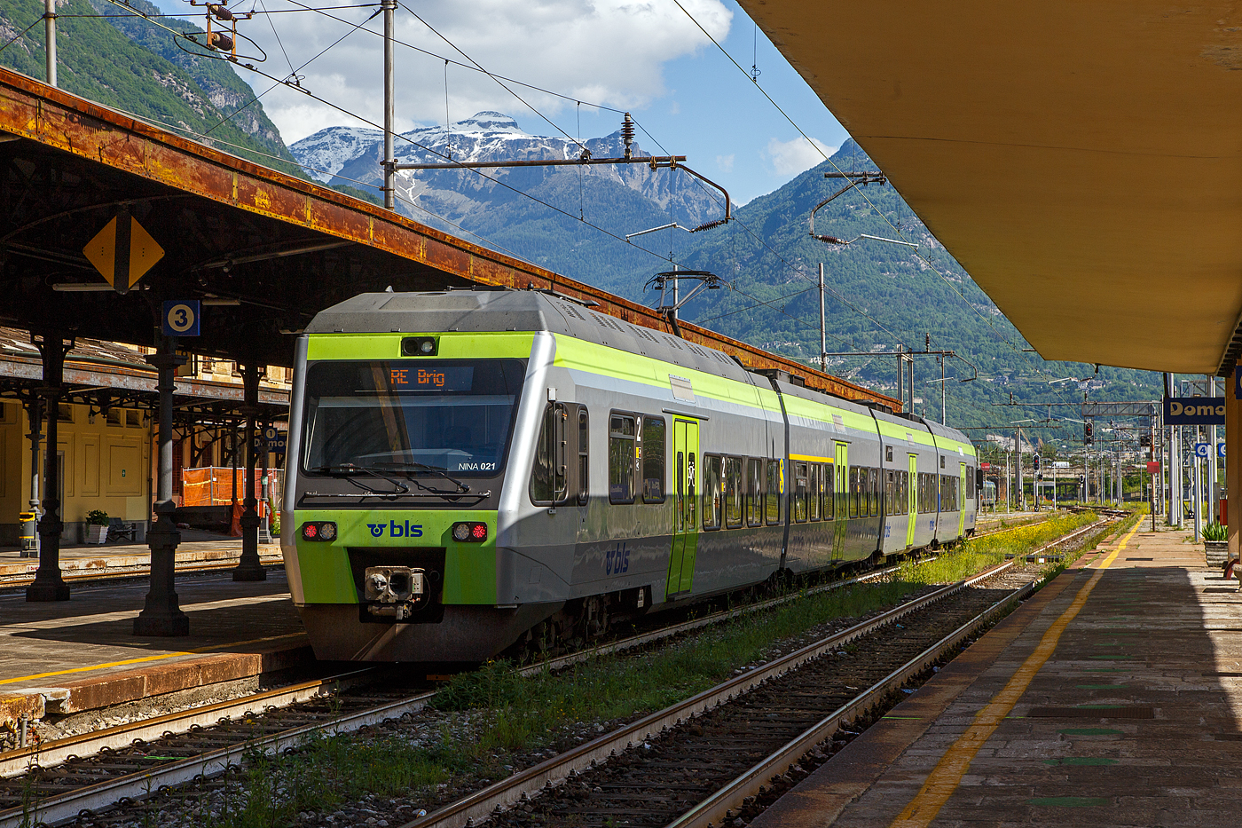 Der vierteilige BLS NINA 021 - RABe 525 021(94 85 7525 021-2 CH-BLS) steht am 26. Mai 2023 als RE nach Brig im Bahnhof Domodossola zur Abfahrt bereit.

Eigentlich sollten die BLS RABe 528 “MIKA” von Bern ber die Ltschberg-Bergstrecke (Kandersteg) und Brig nach Domodossola fahren, aber diese haben noch keine Zulassung fr Italien, die sie hinter dem SBB) Simplontunnel bis Domodossola brauchen. Und so wird der Zuglauf in Brig gebrochen und “NINA” fahren (min. bis zum Sommer) als Ersatz.

Von den BLS NINA (Niederflur-Nahverkehrszug) wurden 41 Stck zwischen 1998–2005 in 5 Serien von Vevey Technologies SA in Villeneuve (vormals ACMV - Ateliers de constructions mcaniques de Vevey) ab 2001Bombardier Transportation zusammen mit Bombardier-Talbot in Aachen (D)gebaut, die elektrische Ausrstung wurde von Alstom/Traxis (vormals Holec) zugeliefert. An die zweite Bestellung der BLS schlossen sich auch die Transports de Martigny et Rgions (TMR) und die Transports Rgionaux Neuchtelois (TRN) an, diese werden jedoch als RABe 527 gefhrt. 

Die klimatisierten Niederflur-Nahverkehrszge „NINA“ bieten modernen Fahrkomfort in erfrischendem Design und verkehren sowohl als 3-teilig wie auch als 4-teilige Komposition. Tiefe Einstiege und groe Plattformen sorgen fr Bewegungsfreiheit, und Geschwindigkeiten von bis zu 140 km/h garantieren attraktive Fahrzeiten. Die dreiteiligen bieten 
148 und die vierteiligen 191 Sitzpltzen. Es knnen bis zu 4 Triebzge aneinandergekoppelt werden (maximal 592 bis 764 Sitzpltze).

Das Fahrzeug wurde Mitte der 1990er-Jahre von Vevey Technologies zusammen mit Bombardier-Talbot in Aachen (D), entwickelt und gebaut. Das Niederflurkonzept und die Drehgestell-Technik stammen weitgehend vom Triebzug Talent, der von Bombardier-Talbot in Aachen entwickelt wurde. Die Drehgestelle weisen eine fast gleiche Konstruktion auf, die lediglich fr die NINA angepasst wurde. Fr die Elektrotechnik war die Firma Holec Machines & Apparaten – die sptere Alstom/Traxis – aus Ridderkerk (NL) zustndig, die, wie die Vevey Technologies zu dieser Zeit auch, zur Begemann-Gruppe aus den Niederlanden gehrte. Seit 2001 firmiert das Unternehmen Vevey Technologies als Bombardier Transportation (Schweiz). Die Fahrzeuge wurden weiterhin im Werk in Villeneuve VD hergestellt.

Die NINA wurden als zwei- bis vierteilige Triebzge angeboten. Angetrieben werden sie von zwei zweiachsigen Triebdrehgestellen unter den Fhrerstnden. Zwischen den einzelnen Wagen sind Jakobsdrehgestelle angebracht. Der Zug zhlt wie der Stadler GTW zu den Leichtbaufahrzeugen. Eine dreiteilige Einheit wiegt leer nur 78 Tonnen (zum Vergleich eine Re 465 Lok  wiegt 84 Tonnen). Die Hchstgeschwindigkeit betrgt 140 km/h.

Die BLS beschaffte 1998 eine erste Serie von acht dreiteiligen Einheiten. Diese Fahrzeuge wurden nachtrglich mit einem WC ausgerstet. Im Jahre 2000 folgte eine Nachbestellung ber sechs Fahrzeuge, denen eine dritte Serie ber 18 Fahrzeuge folgte, die Ende 2002 bestellt wurden. Mit der im Jahre 2003 erfolgten vierten Bestellung ber vier Fahrzeuge erhhte sich der Bestand auf insgesamt 36 Einheiten. Um die Sitzplatzkapazitt zu erhhen, wurden im Jahre 2007 die dreizehn RABe 525 015 bis 027 um je einen Zwischenwagen zu vierteiligen Triebzgen verlngert. Ab 2009 erhielten die NINA eine Klimaanlage.

An die zweite Bestellung der BLS schlossen sich auch die Transports de Martigny et Rgions (TMR) und die Transports Rgionaux Neuchtelois (TRN) an. 

TECHNISCHE DATEN:
der RABe 525 NINA dreiteilig nach Refit, in Klammern vierteilig
Spurweite:  1.435 mm (Normalspur)
Achsfolge:  Bo'2'2'Bo'   (Bo'2'2'2'Bo')
Lnge ber Puffer: 47.740 mm  (61.900 mm)
Achsabstand im Triebdrehgestell: 2.500 mm
Achsabstand im Laufdrehgestell (Jakobsdrehgestell): 2.700 mm
Hhe: 4.315 mm
Breite: 3.030 mm
Gewicht: 79,0 t  (96.0 t)
Dauerleistung: 1.000 kW / 1.360 PS
Anfahrzugkraft: 105 kN
Hchstgeschwindigkeit: 140 km/h
Stromsystem: 15 kV 16⅔ Hz AC
Sitzpltze in der 1. Klasse: 20  (20)
Sitzpltze in der 2. Klasse: 114  (159)
Rollstuhlpltze: 1  (1)
Fahrradpltze/Velopltze: 3  (9)

Quellen: BLS, wikipedia