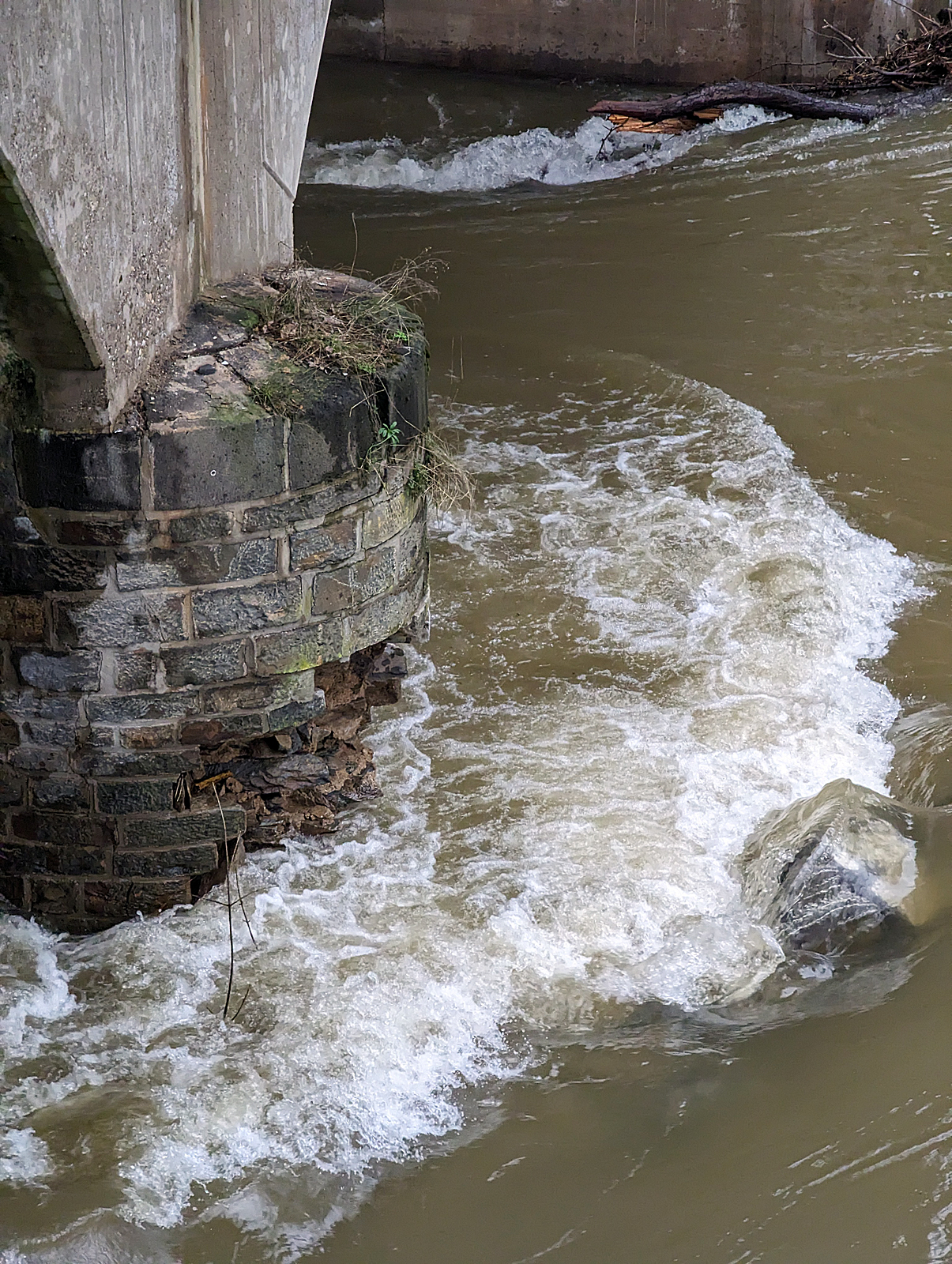 Detailbild (mit Smartphone) von dem betroffenen Fundament des Brückenpfeilers der Eisenbahn-Siegbrücke mit Fußgängersteg in Kirchen (Sieg), der KBS 460 Siegstrecke. Wie weit der Schaden im/unter Wasser ist kann man nicht erkennen, aber ich würde es auch nicht verantworten wollen. Hier am 03.01.2024.