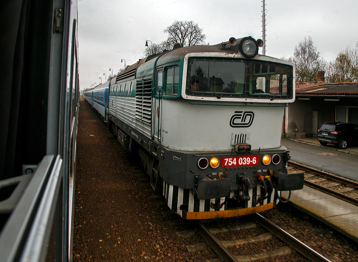 Die „Taucherbrille“ ČD 754 039-6 (CZ- ČD 92 54 2 754 039-6) steht am 22.11.2022 mit einem Regionalzug im Bahnhof Nýřany (Nürschan). 

Die ČD-Baureihe 754, ehemalige ČSD-Baureihe T 478.4 (der ehemaligen Tschechoslowakischen Staatsbahn), ist eine dieselelektrische Universallokomotive mit elektrischer Zugheizung (3000 V=). Durch das markante äußere Erscheinungsbild mit den blendfreien Führerständen verdanken die Lokomotiven ihren Spitznamen „Brejlovec“ (Brillenschlange) bzw. in Deutschland eher Taucherbrille.

Die Lokomotiven sind eine Weiterentwicklung des Vorgängertyps T 478.3 (ab 1988 Baureihe 753), dabei erhielten sie stärkere Motoren und eine elektrische Zugheizanlage. Die ersten beiden Prototypen entstanden 1975 bei ČKD in Prag. In den Jahren 1978–1980 wurden dann 78 Serienlokomotiven gefertigt. Mit der Einführung des EDV-Nummernsystems im Jahre 1988 erhielten die Lokomotiven die neue Baureihennummer 754 mit nur noch 3-stelliger Ordnungsnummer.

Die Maschinen sind bei den heutigen České dráhy (ČD) und Železničná spoločnosť (ZSSK) noch im Einsatz.Fünf Lokomotiven der ČD sind seit 2014 an das polnische Eisenbahnverkehrsunternehmen PKP Intercity verliehen, das die Fahrzeuge auf nicht elektrifizierten Strecken vor hochwertigen Fernreisezügen einsetzt. Der Mietvertrag wurde im Dezember 2020 verlängert.

Fahrzeugaufbau:
Die Lokomotiven haben einen Brückenrahmen, auf dem das Gerippe für die Seitenwände aus schräglaufenden Profilstreben aufgebaut ist. Der Kasten verfügt über gesickte Seitenwände. In den Seitenwänden befinden sich sechs runde Fenster. Die beiden vorderen Führerstände
sind über einem zentralen begehbaren Maschinenraum verbunden. Die Drehgestelle wurden H-förmig aufgebaut und sind vollständig geschweißt. Im mittleren Querträger befindet sich die Führung für den Drehzapfen. Die Lagerungen sind seitenverschiebbar ausgeführt. Der Zapfen stützt sich in der Längsachse des Triebfahrzeuges auf Gummimetalleinlagen. Den Seitenverschub der Drehgestelle begrenzen Gummimetallanschläge.

Die Achslagerführung besteht aus Schwingarmen. Sie sind mit den Drehgestellrahmen über in Gummimetallbuchsen eingesetzten Zapfen verbunden. Die Abfederung der Achsen, die alle über Schwenklager in Schwingarmen gelagert sind, erfolgt einzeln vertikal. Dabei werden je ein Paar zylindrische Schraubenfedern und hydraulische Dämpfer verwendet.

Das Dach ist in drei Segmente unterteilt und kann bei Montage- und Demontagearbeiten vollständig abgenommen werden. Unter dem Dachvorderteil befinden sich u. a. die Haupt- und Hilfsluftbehälter, im hinteren Teil befinden sich die Kühlanlage und der Lüfter. Im mittleren Teil des Daches befinden sich die Ansaugkanäle des Abgasschalldämpfers.

Die Lokomotive verfügt über acht Sandkästen mit einer Gesamtkapazität von 350 kg Sand, der unter Druck unter den Rädern transportiert wird.

Maschinenanlage:
Der Motorgenerator besteht aus einem Verbrennungsmotor und einem direkt angeschlossenen Traktionsgenerator. Andere Antriebe sind von beiden Seiten mit dem Motorgenerator verbunden. Der Dieselmotor ist ein OHV wassergekühlter V12 Zylindern-Viertakt-Dieselmotor mit Direkteinspritzung zwei Abgas-Turboladern und Ladeluftkühlung vom Typ ČKD K 12 V 230 DR mit einer Leistung von 1.460 kW (1.985 PS). Jeder Zylinder hat eine eigene Einspritzpumpe. Der Motor hat zwei Nockenwellen. In jedem Zylinderkopf befinden sich je zwei Einlass- und Auslassventile mit einer Einspritzdüse in der Mitte. Die Kolben sind mit vier Kolbenringen ausgestattet. Der Motorhubraum 	beträgt 129,36 Litern Zylinderdurchmesser 230 mm, Kolbenhub 260 mm, das Kompressionsverhältnis ist 12,5 : 1. Die Nenndrehzahl beträgt 1.100 U/min, die Leerlaufdrehzahl 480 U/min. Der Motor wiegt 11.575 kg ohne Generator.Die Motorleistung wird kontinuierlich von einem Motorregler mit Drehzahlregler gesteuert, aber alle Motorbefehle werden zuerst vom elektronischen Regler verarbeitet. Der Kraftstofftank ist zusammen mit der Batterie zwischen dem Fahrgestell unter dem Hauptrahmen aufgehängt. Der Motorstart wird durch den Traktionsgenerator sichergestellt. 

Der angeflanschte Generator ist vom vom Typ TD 804 B, der technisch auf dem Generator TD 802 E der Baureihe 753 basiert, eine vierpolige fremderregte Gleichstromlichtmaschine mit eigener Belüftung. Der Traktionsdynamo treibt den Heizungsgenerator A 403 II an, eine Drehstrom-Wechselstrommaschine, die mit einer Spannung von 3.000 V DC nicht nur die elektrische Zugheizung, sondern auch die Erregung des Traktionsdynamos bereitstellt. Das Batterieladegerät D 206p wird vom Heizungsgenerator gespeist.

Die Lokomotive kann manuell oder automatisch gesteuert werden. Im manuellen Modus gibt der Lokführer die Motordrehzahl kontinuierlich mit dem Fahrhebelregler ein, während im automatischen Geschwindigkeitsregelungsmodus der Lokführer mit demselben Hebel die gewünschte Geschwindigkeit wählt, die dann von der Automatik gehalten wird. 

TECHNISCHE DATEN der BR 754, ex T 478:
Hersteller: ČKD Praha
Baujahre: 1978 bis 1980 (1975 Prototypen)
Hergestellt e Anzahl: 86
Spurweite: 1.435 mm (Normalspur)
Achsfolge: Bo'Bo'
Länge über Puffer: 16.540 mm
Höhe: 4.335 mm
Breite: 3 074 mm
Drehzapfenabstand: 6.700 mm
Achsabstand im Drehgestell: 2.400 mm
Treibrad-Ø: 1.000 mm (neu) / 920 mm (abgenutzt) 

Dieselmotor: wassergekühlter V12-Zylinder-Viertakt-Reihen- Dieselmotor mit Direkteinspritzung, Abgasturbolader und Ladeluftkühlung, vom Typ ČKD K 12 V 230 DR. Weitere Motodaten s. im Text.
Dauermotorleistung: 1.460 kW (1.985 PS)

Traktionsgenerator: Typ TD 804 B
Leistung des Traktionsgenerators: 1.200 kVA
Leistungsübertragung: diesel-elektrisch (Gleichstromübertragung)
Anzahl der Fahrmotoren: 4 vom Typ TE 005 E
Fahrmotorleistung: 4 x 300 kVA
Höchstgeschwindigkeit: 100 km/h
Kleinste Dauergeschwindigkeit: 32 km/h
Dienstgewicht: 74 t
Anfahrzugkraft: 215 kN
Dauerzugkraft: 123 kN
Max. Tankinhalt: 3.600 l
Kleinster bef. Halbmesser: R 100 m

Quellen: Wikipedia, atlaslokomotiv.net
