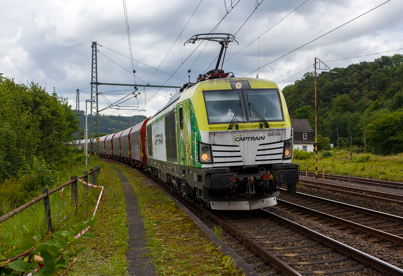 Die an die Dortmunder Eisenbahn GmbH (DE) vermietete SIEMENS Vectron Dual Mode 248 034-1  Phoenix  (90 80 2248 034-1 D-DE) der Captrain Deutschland GmbH fährt am 01 Juli 2024, mit einem Coilzug (Wagen der Gattung Shimmnis-ttu der Ermewa) durch Scheuerfeld/Sieg in Richtung Köln. 

Die SIEMENS Vectron DM wurde 2022 von Siemens Mobility GmbH in München-Allach unter der Fabriknummer 23185 gebaut und im Februar 2023 an die Captrain ausgeliefert. Die Lok hat die Zulassung für Deutschland und eine Höchstgeschwindigkeit von 160 km/h. Die Hybridlok (Vectron Dual Mode) kann die Antriebsenergie aus der Fahrleitung beziehen (2.400 kW Leistungen am Rad), oder mittels eines MTU 16V 4000 R84 V16-Zylinder-Dieselmotors (2.400 kW Motorleistung, 2.000 kW Leistungen am Rad) erzeugen.

Die Dortmunder Eisenbahn GmbH (DE) ist eine private Eisenbahngesellschaft aus Dortmund. Die Dortmunder Eisenbahn GmbH ist ein gemeinsames Tochterunternehmen der Dortmunder Hafen GmbH und der Captrain Deutschland GmbH. Sie ist zu 65 Prozent im Besitz der Captrain Deutschland GmbH (deutsche Tochter der SNCF) und 35 Prozent der Anteile hält die Dortmunder Hafen AG. Die DE Infrastruktur GmbH, mit ca. 50 Kilometern Gleislänge, gehört zu 81 Prozent der Dortmunder Hafen AG und zu 19 Prozent der Captrain Deutschland GmbH.