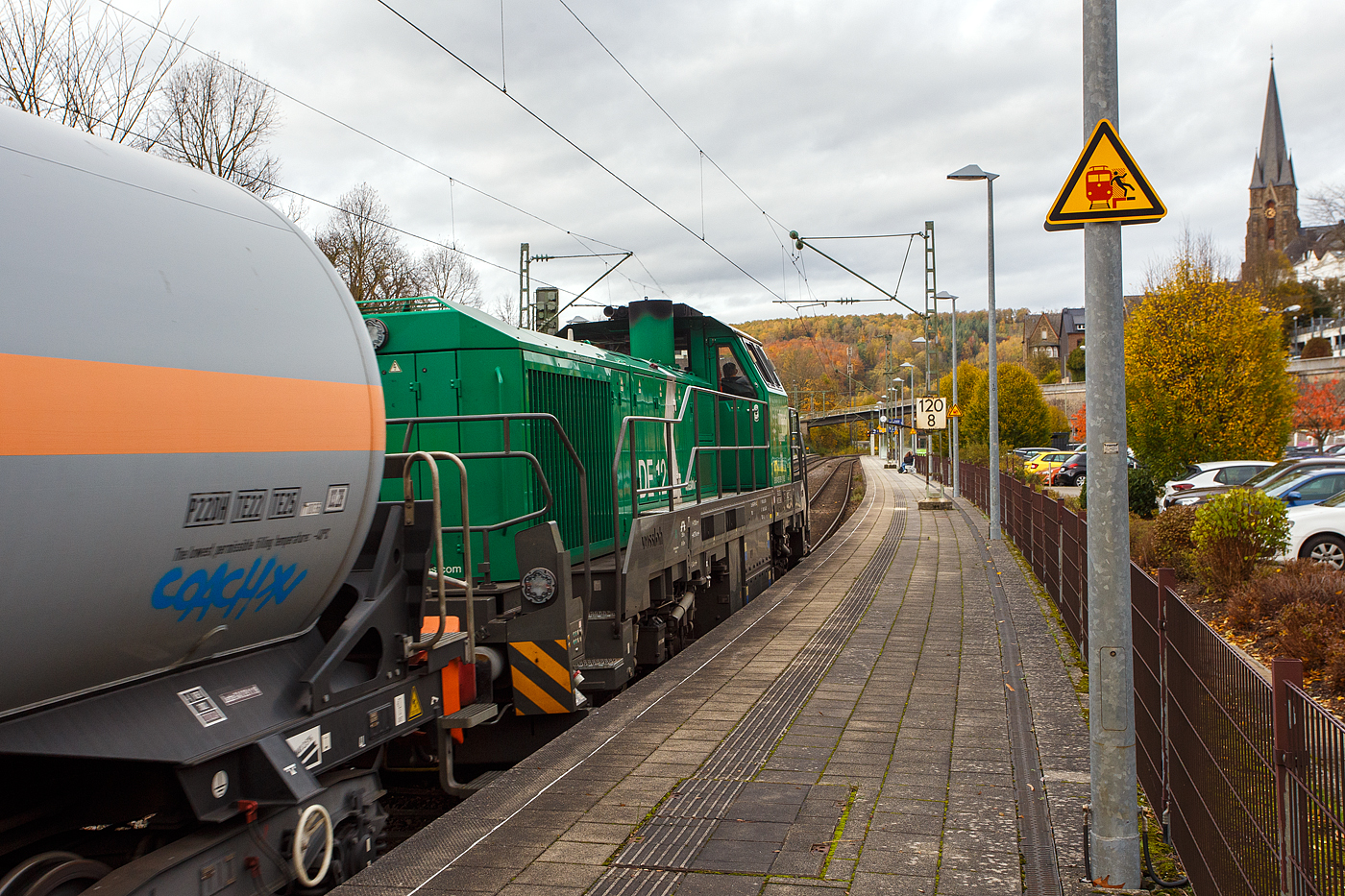 Die dieselelektrische Vossloh DE 12 / 4125 006-1 (92 80 4125 006-1 D-ISL) / Lok 11 der InfraServ Logistics GmbH (Frankfurt/M-Höchst) fährt am 29 Oktober 2025 mit einem Kesselwagenzug durch Kirchen (Sieg) in Richtung Siegen, vermutlich mit dem Ziel Frankfurt am Main-Höchst. Die Wagen waren laut Gefahrguttafelen (265/1017) mit Chor beladen. 

Die DE 12 wurde 2020 von Vossloh in Kiel unter der Fabriknummer 5402431 gebaut und an die InfraServ Logistics gefiefert.

Die InfraServ Logistics GmbH ist eine Tochtergesellschaft der Infraserv Höchst, diese ist Standortbetreiber des Industriepark Höchst in Frankfurt am Main sowie weiterer Standorte und ist eines der vielen Nachfolge-Unternehmen der aufgespaltenen Hoechst AG. Die InfraServ Logistics führt den werk sinternen Verkehr innerhalb des Industrieparks Höchst, aber auch den Güterverkehr auf dem Schienennetz der Deutschen Bahn im regionalen Bereich (Rhein-Main, Rhein-Necker und Rhein-Ruhr) durch. 

Die Vossloh DE 12 (BR 4125):
Die Vossloh DE 12 ist eine vierachsige dieselelektrische Mittelführerhaus-Lokomotive des Herstellers Vossloh, die für den schweren Rangier- und den leichten Streckendienst konzipiert ist. Von ihr wurden ab 2012 bis 2020 insgesamt z.Z. 13 Stück gebaut, somit ist sie weitaus erfolgreicher als das dieselhydraulische Einzelstück D 12 (4120 001-7). Die Lokomotiven besitzen im deutschen Fahrzeugeinstellungsregister die Nummer 92 80 4125 xxx-x. 

Entwicklung:
Als Weiterentwicklung der MaK DE 1002 bis MaK DE 1004 entstanden diese Lokomotiven 2012 bei Vossloh in Kiel. Der neue Lokomotivtyp wurde entsprechend den Anforderungen der TSI konstruiert und hergestellt. Somit ist ein europaweit länderübergreifender Einsatz vorbereitet.

Zusammen mit diesem Loktyp hat Vossloh auch eine dieselhydraulische Variante mit der Bezeichnung G 12 auf dem Markt gebracht, es blieb aber bei einem Einzelstück. Vorgestellt wurde die DE 12 erstmals auf der InnoTrans 2012. Wegen der Anpassungen an neue Bahnvorschriften wird der Typ als Vertreter der fünften Generation von Mak- bzw. Vossloh-Loks bezeichnet. Im neuen Bezeichnungsschema wird die Motorleistung (1.200 kW) geteilt durch 100 zum Ausdruck gebracht.

Technik:
Die Konstruktion der Baureihe DE12 ist für den schweren Rangier- und leichten Streckenbetrieb besonders nach den Gesichtspunkten Wirtschaftlichkeit und Ausfallsicherheit ausgelegt. Die bewährte Konstruktion der Vorgängermaschinen wurde nach den Grundsätzen neuester europäischer Normen überarbeitet. So sind der Lokrahmen sowie die Aufbauten der DE 12 nach der Crash-Norm EN 15227 ausgelegt und bieten somit noch mehr Sicherheit für das Lokpersonal bei Unfällen.

Als Antriebsmotor wurde der wassergekühlte MTU 90°-V8-Zylinder-Viertakt-Dieselmotor mit Common-Rail-Einspritzung, Abgasturbolader und Ladeluftkühlung vom Typ 8V 4000 R43L von der MTU (Motoren- und Turbinen-Union) Friedrichshafen GmbH verwendet. Dieser Motor ist nach der Abgasstufe EU Stage IIIA ausgelegt. Für noch größere Verringerung der Abgasemission kann zusätzlich noch ein Rußpartikelfilter verwendet werden. Die Kraftübertragung erfolgt dieselelektrisch mittels Drehstrom-Antriebstechnik. Die Radsätze sind mit Scheibenbremsen versehen.

TECHNISCHE DATEN:
Gebaute Anzahl: 13
Spurweite: 1.435 mm (Normalspur)
Achsfolge: Bo'Bo'
Länge über Puffer: 17.000 mm  
Größte Höhe:  4.310 mm  
Größte Breite:  3.080 mm
Drehzapfenabstand: 8.100 mm
Achsabstand im Drehgestell: 2.400 mm
Raddurchmesser: 1.000 mm (neu) / 920 mm (abgenutzt)
Dieselmotor: MTU 90°-V8-Zylinder-Viertakt-Dieselmotor mit Common-Rail-Einspritzung, Abgasturbolader und Ladeluftkühlung vom Typ 8V 4000 R43L
Dieselmotorleistung: 1.200 kW (1.630 PS) bei 1.800 U/min / 6.548 Nm
Motorhubraum: 38.1 l (Ø 170 mm Bohrung x 210 mm Hub)
Motorabmessungen: 2.000 x 1.565 x 1.860 mm
Motorgewicht: 6.270 kg (trocken)
Abgasvorschriften: EU/2004/26 Stufe IIIA/prepared for stage IIIB  
Leistungsübertragung: elektrisch
Stromrichter: IGBT
Traktionsmotoren: 4 Stück Drehstrom-Asynchronmotoren Drehstrom-Asynchron-Lokomotiv-Motoren (fremdbelüftet) vom Typ VEM DKLBZ 3510-4 (á 400 kW / 865 U/min). Übrigens die Marke „VEM“ ist eine der sehr wenigen ostdeutschen (DDR) Marken die die Wende und bis heute erfolgreich überstanden haben. Seit mehr als 130 Jahren entwickelt und fertigt VEM elektrische Maschinen für die Verkehrstechnik. Vermutlich sind auch der Generator und andere elektrischen Teile von VEM.
Höchstgeschwindigkeit: 120 km/h 
Anfahrzugkraft: 300 kN
Dauerzugkraft: 259 kN
Dienstgewicht: 90 t
Bremse: 2 x KE-GP-E mZ (D)
Max. elektrodynamische Bremsleistung: 1.450 kW
Kraftstoffvorrat: 3.000 bis 4.000 Liter
Kleinster befahrbarer Bogenradius: 55 m
Fährbootwinkel: 1° 30’
