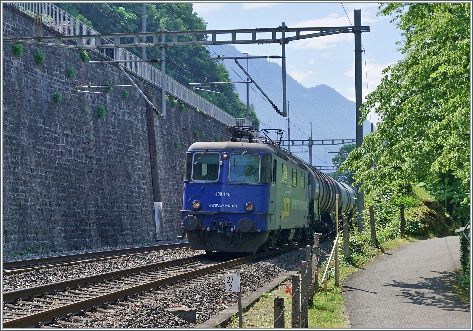 Die ehemalige SMB Re 4/4 181 ist heute als WRD Re 430 115 unterwegs; beim Château de Chillon im ungünstigen Gegenlicht auf der Fahrt in Richtung Lausanne. 

31. Mai 2023