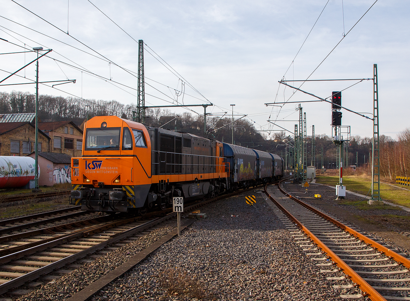 Die KSW 43 (92 80 1273 018-2 D-KSW), die asymmetrische Vossloh G 2000 BB der KSW (Kreisbahn Siegen-Wittgenstein) fhrt am 09.02.2023, mit ihrem Coilzug (VTG Coilwagen der Gattung Shimmns-ttu), von Betzdorf (Sieg) ber Siegen, Dillenburg und Haiger nach Herdorf, was einem Umweg von ber 62 km bedeutet. (Aufnahme vom Bahnsteig 106)

Eigentlich wrde der Zug hier auf die KBS 462 – Hellertalbahn abbiegen und er wre in 7,2 km am Ziel. Aber die Hellertalbahn bleibt, nach dem Felssturz am 23.12.2022 in Herdorf bis voraussichtlich zum kleinen Fahrplanwechsel am 09. Juni 2023 gesperrt. Ein weiterer Nachteil ist das die Strecke Haiger – Herdorf nur die Streckenklasse CE hat und zudem sehr Steigungsreich ist. Die 7,2 km lange Strecke Betzdorf – Herdorf hat die Streckenklasse D4, so knnen die Coilwagen auch nur abgelastet zugestellt werden.

Nochmal einen lieben Gru an den netten Lokfhrer zurck.

Zudem habe ich es hier nicht verstanden, warum der KSW-Zug erst auf den Regionalverkehr warten musste bevor es weiter ging. Denn der Zug knnte doch ohne Halt durchfahren.
