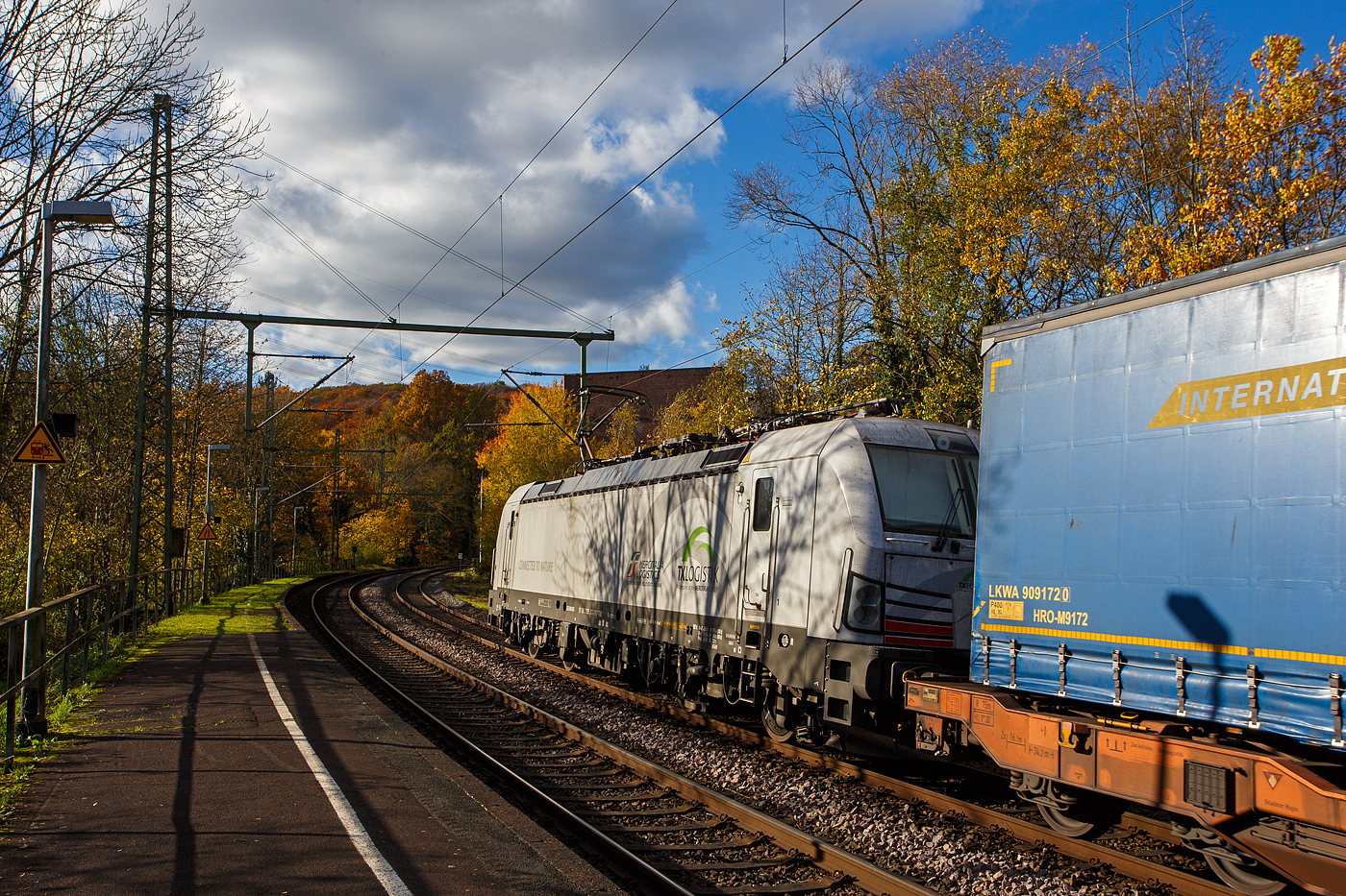 Die recht neue weiße TXL 7193 309 „Connected to Nature“ (91 80 7193 318-1 D-TXL) der TXL - TX Logistik AG (Troisdorf) fährt am 30 Oktober 2025 mit einem KLV-Zug durch Scheuerfeld/Sieg in Richtung Köln. Als Schlussläufer war am Zugschluss zudem die kalte, an die HSL Logistik GmbH vermietete, AKIEM 186 383-6.

Nochmals einen lieben Gruß an den netten Lokführer zurück.

Die SIEMENS Vectron MS (X4E) wurde 2024 von Siemens Mobility in München-Allach unter der Fabriknummer 24282 gebaut und am 24.01.2025 an die TXL ausgeliefert. Die mit 6.400 kW konzipierte Mehrsystemlok ist in der Variante A22-11i ausgeführt und hat so die und hat so die Zulassungen und entspr. Länderpakete für Deutschland, Österreich, Schweiz, Italien und die Niederlande (D / A / CH / I / NL).

Über TX Logistik AG
TX Logistik wurde 1999 als privates Eisenbahnverkehrsunternehmen gegründet und bietet mit Verbindungen in elf Ländern ein leistungsfähiges europäisches Netzwerk. Das Unternehmen verfügt über Tochtergesellschaften in der Schweiz, Österreich, Dänemark und Schweden sowie eine lokale Präsenz in Italien. In den Geschäftsbereichen Intermodal und Rail Freight entwickelt TX Logistik umfassende Schienenlösungen für kontinentale und maritime Verkehre sowie maßgeschneiderte Konzepte für konventionelle Fracht. Mit 650 Mitarbeitern und 8,6 Milliarden gefahrenen Tonnenkilometern erwirtschaftete das Unternehmen 2021 einen Jahresumsatz von 253 Millionen Euro. Seit Januar 2017 gehört TX Logistik zu 100 Prozent der Mercitalia Logistics S.p.A., einer Tochtergesellschaft der FS - Ferrovie dello Stato Italiane. Mittlerweile gehört das Unternehmen mit zu den Größten für den Schienengüterverkehr in Europa.

Das Unternehmen bietet den ganzen Umfang an Schienengüterverkehr, inklusive Containertransport und kombiniertem Verkehr an. Wichtigste Transportstrecken sind von den Häfen Hamburg, Bremerhaven, Rotterdam und Antwerpen nach Süddeutschland, Schweiz, Österreich und Italien.

TX Logistik setzt nun auf eigene Vectron Loks:
Anfang Oktober 2024 hat die TX Logistik AG ersten drei von 40 modernen Vectron-Lokomotiven des Herstellers Siemens Mobility aufs Gleis gesetzt, die das zur Mercitalia Logistics (FS Italiane Group) gehörende Schienenlogistikunternehmen im Mai 2023 bestellt hatte. Die Erweiterung der Fahrzeugflotte ist für TX Logistik eine wichtige Voraussetzung, um im intermodalen und grenzüberschreitenden Schienengüterverkehr weiter zu wachsen. Die neuen Lokomotiven werden vor allem auf dem Brenner- und dem Schweiz-Korridor eingesetzt, den strategisch wichtigen Nord-Süd-Achsen in Europa.

Beide Korridore sind stark frequentiert und stellen hohe Anforderungen an die eingesetzten Lokomotiven – von der Zugkraft über die Stabilität bis hin zur grenzüberschreitenden Systemkompatibilität. TX Logistik hat dazu die Maschinen mit verschiedenen Länderpaketen bestellt. 20 Vectron erhalten das Länderpaket für den Betrieb in Deutschland, Österreich, Schweiz, Italien und den Niederlanden (D-A-CH-I-NL) und sollen bis Anfang 2025 übergeben werden. Die Auslieferung der 20 Lokomotiven mit der Ausstattung für den deutsch-österreichisch-italienischen Korridor (D-A-I) soll bis zum Jahresende 2025 erfolgen.

Die Entscheidung für den Kauf der Vectron-Lokomotiven unterstreicht zugleich das Bestreben von TX Logistik, Schienengüterverkehre als umweltfreundliche und effiziente Alternative zum Straßentransport weiter voranzutreiben. Um dies zu unterstreichen und gleichzeitig für den Einstieg in den intermodalen Transport zu werben, hat die erste der drei Vectrons, die im Zughotel in Braunschweig übergeben wurden, eine spezielle Lok-Beklebung mit dem Schriftzug „Start now (Nature). Driven by Green Passion“ erhalten.

Die neuen Loks bieten mit ihrer Flexibilität und Leistungsfähigkeit ideale technische Voraussetzungen, um den steigenden Anforderungen des europäischen Güterverkehrs gerecht zu werden. Mit der modernen Vectron-Flotte, so TX Logistik, sei man mittelfristig nun in der Lage, die Kapazitäten auf dem Brenner- und dem Schweiz-Korridor deutlich zu erhöhen sowie die Effizienz und Zuverlässigkeit im Schienengüterverkehr weiter zu verbessern.
