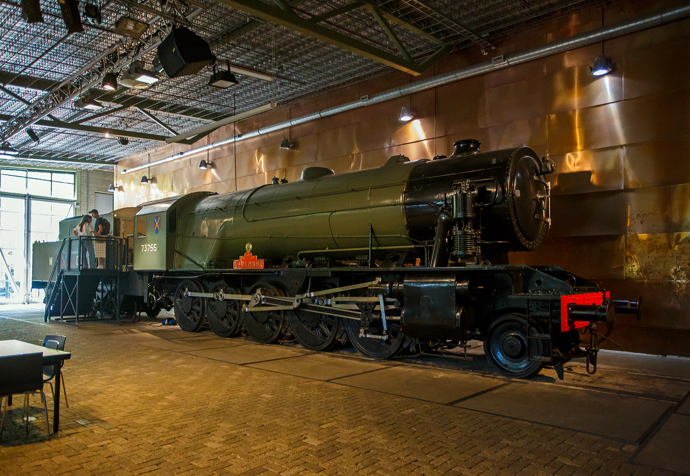 Die WD 73755 „Longmoor“, spätere NS 5085 (NS-Baureihe 5000), eine Dampflokomotive vom Typ WD Austerität 2-10-0 / LMR 600 Gordon, gekuppelt mit einem vierachsigen Tender, am 29 April 2025 im Het Spoorwegmuseum (bis 2005 NSM - Nederlands Spoorwegmuseum / Niederländischen Eisenbahnmuseum) in Utrecht im ehemaligen Bahnhof Maliebaan.  

Die 73755 wurde 1945 unter der NBL-Fabriknummer 25601 gebaut und als WD 3755 an die British War Department (WD) fürs Longmoor Military Railway Corps geliefert, später sie in WD 73755 umgezeichnet. Sie eine von 150 WD-Austerität 2-10-0, die alle von der North British Locomotive Company in Glasgow (GB) gebaut wurden. Sie war die 1000te britische Dampflokomotive, die zur Unterstützung der britischen Armee aufs europäische Festland nach Frankreich verschifft wurde. Nach ihren ereignisreichen Reisen mit den Alliierten wurden 60 Lokomotiven von der NS 1946 geleast. Weitere 43 kamen im Juni hinzu. 1947 gingen sie in den Besitz der NS über, die die Lokomotive übernahm, die diese als Baureihe/Serie 5000 einreihte (NS 5001 bis 5103). So wurde aus dieser die NS 5085. Die letzten Lokomotiven dieser Baureihe wurden 1952 außer Dienst gestellt.

Die NS 5000 war eine Reihe von Dampflokomotiven der NS - Nederlandse Spoorwegen (Niederländischen Staatsbahnen, heute Niederländische Eisenbahnen AG), die vom British War Department (WD) übernommen wurden. Sie hatten den Spitznamen „Grote Jeep“ (Großer Jeep).

Die Lokomotiven mit der Radanordnung 1'E (2-10-0) wurden zwischen 1943 und 1945 von der North British Locomotive Company in Glasgow für das britische Kriegsministerium gebaut, um Waren zur britischen Armee während des Krieges gegen Nazi-Deutschland im westeuropäischen Festland zu transportieren. 

Die britische Armee gründete ein separates Eisenbahnkorps, das Longmoor Military Railway Corps. Dieses Regiment war für den Betrieb von Militärzügen in befreiten Gebieten verantwortlich. Während des Zweiten Weltkriegs gab das britische Kriegsministerium eine große Anzahl dieser Lokomotiven in Auftrag, die die Invasionsarmee begleiteten. Zwei Serien wurden von der North British Locomotive Company gebaut. Die erste Lieferung von 100 Lokomotiven wurde 1943/1944 eingeführt, die zweite Lieferung von 50 Lokomotiven 1945. Ihre WD-Nummern waren 3650–3749 (später 73650–73749) und 73750–73799. Zunächst wurden sie in England eingesetzt, waren aber aufgrund ihrer Länge weniger geeignet. Die meisten wurden erst nach dem D-Day bei der britischen Armee in Frankreich in Dienst gestellt. Nach dem Krieg war der Großteil der Loks in den Niederlanden.

Die Loks mit der geringen Achslast von 13,7 Tonnen machte sie sehr geeignet für den Betrieb auf provisorischen oder reparierten Bahnstrecken. Während der britischen Besatzung wurden mehrere Lokomotiven in Gebieten südlich der Niederlande eingesetzt. Um den Oktober 1945 wurden die Loks außer Betrieb genommen und eingelagert.

Um den Eisenbahnverkehr nach der deutschen Kapitulation im Mai 1945 in Gang zu bringen, wurde die Klasse anstelle von niederländischen heimischen Dampfloks eingesetzt, die während des Krieges zerstört oder beschädigt wurden. Anfang 1946 wurde beschlossen, dass die NS etwa sechzig Lokomotiven als NS 5001-5060 für den Zugdienst anschaffen würde. Später wurde diese Zahl um weitere 43 Lokomotiven ergänzt, so dass die Baureihe NS 5001-5103 entstand.

Die NS senkte den Dampfdruck bald von 15,8 kg/cm² 225 psi auf 12 kg/cm² (170 psi) und machte die Schornsteine länger, um den Rauch aus dem Sichtfeld des Lokführers zu bringen. Zudem wurde das Führerhaus umgebaut und eine verbesserte Tenderkupplung angebaut. Diese Lokomotiven wurden bereits zwischen 1948 und 1952 wieder aus dem Dienst genommen. Die NS setzte schon früh auf Diesel- und Elektroantrieb. Da wurden für die Deutsche Bundesbahn noch neue Dampfloks gebaut, die letzte 1959 mit der bei Jung (Jungenthal) mit der Fabriknummer 13113 die 23 105. 

An die 1.000th gebaute Lokomotive, die nach Kontinentaleuropa verschifft wurde, wird erinnert. Diese Lokomotive mit dem Namen  Longmoor   wurde im Niederländischen Eisenbahnmuseum in Utrecht erhalten und in die Kriegsabteilung mit der Nummer WD 73755 zurückversetzt. Als Werbung erhielt sie den Namen Longmoor.

Das Longmoor Military Railway Corps wurde 1968 aufgelöst.

TECHNISCHE DATEN:
Hersteller: North British Locomotive Company, Glasgow (GB)
Anzahl bei der NS:103
Nummerierung: NS 5001-5103
Außer Dienststellung:  1948-1952
Spurweite: 1.435 mm (Normalspur)
Achsfolge: 1'E (engl. 2-10-0) 
Länge über Puffer: 20.580 mm (Lok 12.600 mm + Tender 7.980 mm)
Treibraddurchmesser: 1.435 mm (neu)
Laufraddurchmesser: 838 mm (neu)
Höchstgeschwindigkeit: 65 km/h (40 mph)
Gesamtheizfläche: 215,3 m²
max. Dampfdruck: 15,8 kg/cm² (225 psi) später 12 kg/cm² (170 psi)
Anzahl der Zylinder: 2 außenliegend (Ø 457 mm x 660 mm Hub)
Steuerung: Walschaerts (entspr. Heusinger)
Dienstgewicht: Lok 79,6 und Tender 56,4 t = 136 t
Anfahrzugkraft: 152,20 kN, später mit 12 bar Dampfdruck 95.12 kN
Wasservorrat: 22,7 m³
Kohlevorrat: 9,1 t

Quellen: Het Spoorwegmuseum, nmld.nl und Wikipedia (NL und GB)
Stand/Überarbeitung: September 2025

