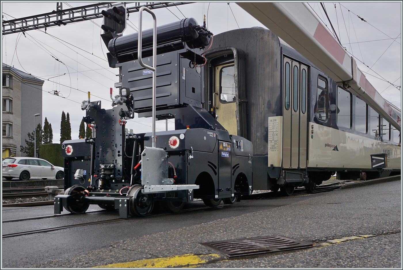 Ein Blick unter der Barriere in Chernex auf den neuen ZAGRO E-MAXI (mit Batterieantrieb). Das Bild zeigt, dass der ZAGRO E-MAXI vier Achsen aufweist, wobei die beiden inneren Achsen wohl gummibereif und ohne Spurkranz dem Antrieb auf Schiene und Strasse dienen. 

20. Februar 2026  
