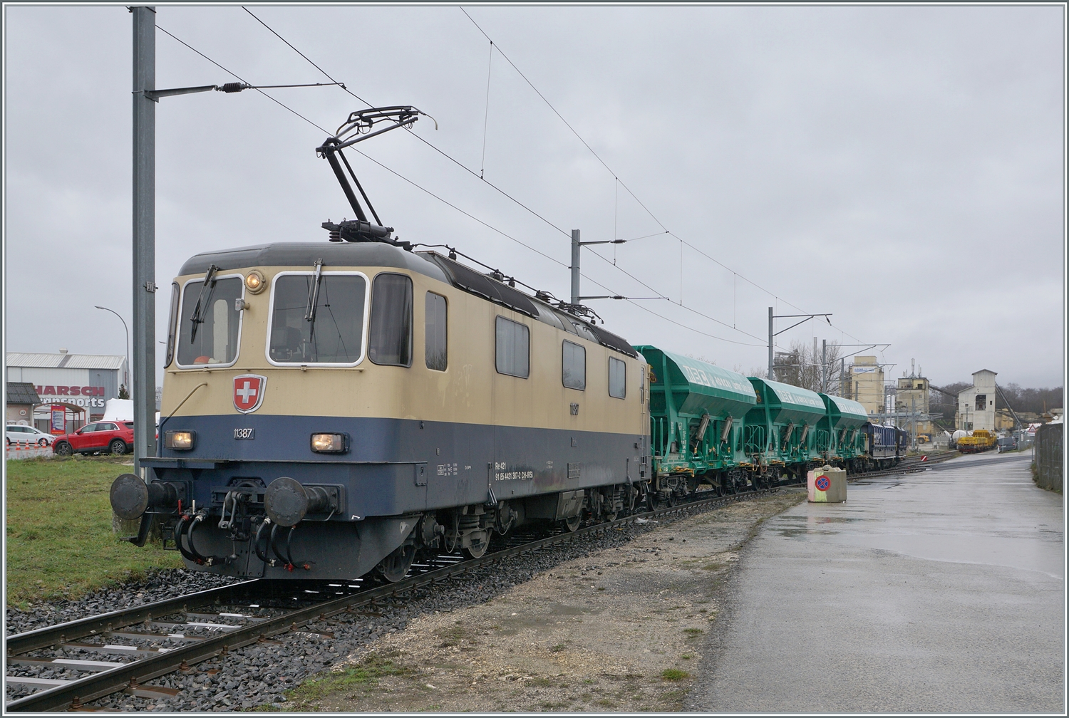 Etliche Regentropfen später kommt die IRSI/IGE  Rheingold  Re 4/4 II 11387 (Re 421 387-2) nun mi ihrem Güterzug nach Apples am Haken wieder aus dem Industrie Gelände bei Gland angefahren.

22. Februar 2024