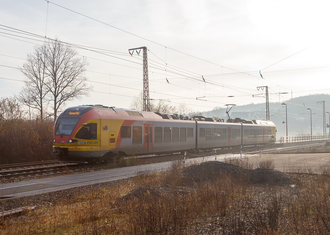 Noch im Dunst/Nebel, der 3-teilige Stadler FLIRT 427 042 / 827 042 / 427 542 (94 80 0427 124-3 D-HEB / 94 80 0827 124-9 D-HEB / 94 80 0427 624-2 D-HEB) der HLB Bahn (Hessischen Landesbahn) verlässt am 22.02.2023, als RE 99 Gießen – Siegen (Umlauf HLB 24556), den Hp Ruderdorf (Kreis Siegen) und fährt weiter in Richtung Siegen.