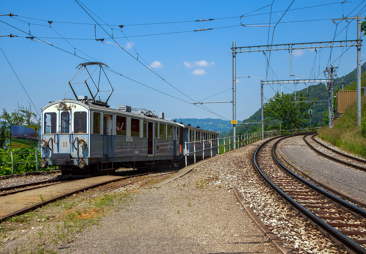 Pfingsten 2023 (Samstag 27. bis Montag 29. Mai 2023) fand bei der Museumsbahn Blonay–Chamby das Schweizer Dampffestival 2023 / Festival suisse de la Vapeur 2023 statt.

Der ex MOB BCFe 4/4 11 mit dem vierachsigen Personenwagen MOB BC 22 erreichen am 27.05.2023 den Bahnhof Chamby.

Der Triebwagen mit 2. und 3. Klassen- sowie Gepäckabteil wurde 1905 von der Schweizerischen Industrie-Gesellschaft (SIG) in Neuhausen am Rheinfall hergestellt und mit einer elektrischen Ausrüstung von der Elektrizitätsgesellschaft Alioth versehen. Der TW Nr. 11 ist der letzte erhaltene der Serie (von 14 Stück) und sogar als BCFe 4/4 11 betriebsfähig. Er ist Eigentum der Museumsbahn. Der vierachsigen Personenwagen MOB BC 22 wurde bereits 1902 von SIG gebaut. Der TW Nr. 11 ist der letzte erhaltene der Serie (von 14 Stück) und sogar als BCFe 4/4 11 betriebsfähig. Er ist Eigentum der Museumsbahn.

Die BCFe 4/4 7 bis 20 sind bzw. waren elektrische Meterspur-Triebwagen. Sie wurden zwischen 1904 und 1906 von der MOB (Montreux–Berner Oberland-Bahn, französisch Chemin de fer Montreux Oberland) beschafft. Diese Triebfahrzeugserie ist mit vierzehn Fahrzeugen die größte, die bis heute von der Montreux–Berner Oberland-Bahn beschafft wurde. Allerdings waren nur dreizehn Triebwagen gleich, einer hatte eine abweichende elektrische Ausrüstung von MFO. Verwandt mit diesen sind auch die beiden CFZe 4/4 1001 und 1002, welche sich nur im Kastenaufbau unterscheiden. Rahmen, Untergestelle und elektrische Ausrüstung sind gleich. Beide Triebwagenbaureihen wurden von SIG hergestellt und mit einer elektrischen Ausrüstung von der Elektrizitätsgesellschaft Alioth versehen, mit Ausnahme der Triebwagen BCFe 4/4 12 und CFZe 4/4 1002, die eine elektrische Ausrüstung von der Maschinenfabrik Oerlikon (MFO) erhielten.

Geschichte:
Für die Eröffnung des Bahnstrecken-Teilstückes Montbovon–Château-d'Oex–Gstaad im Jahre 1904 und Gstaad–Zweisimmen im Jahre 1905 stieg der Bedarf an Fahrzeugen bei der MOB an. Die entsprechenden Fahrzeuge wurden in den Jahren 1902 und 1903 bestellt. Insgesamt ging es dabei um eine Beschaffung von 16 Triebwagen, 21 zweiachsigen Personenwagen und 42 Güterwagen. Bei den 16 Triebwagen handelte es sich um die 14 BCFe 4/4 7 bis 20 und die beiden CFZe 4/4 1001 und 1002.

Technik:
Die Fahrzeuge hatten einen verblechten Holzkasten, der auf einem genieteten Stahlrahmen ruhte. Die vierpoligen eigenventilierten Gleichstrom-Motoren wurden als Einzelachsantriebe in den beiden zweiachsigen Drehgestellen ausgeführt. Über einen geschlossenen Tatzlager-Antrieb mit zweiteiligen elastischen Zahnrädern und einer Übersetzung (bei Ablieferung) von 1:4,33 wurde die Kraft auf die Achse mit Triebrädern von 860 mm Durchmesser übertragen. Bei 700 Volt an der Motorenklemme entwickelte jeder Motor an der Welle eine Stundenleistung von 65 PS (48 kW). Zusammen leisteten die vier Motoren somit 260 PS (192 kW).

Die Steuerung der Motoren erfolgte über einen Direktkontroller mit zehn Fahr- und fünf Bremsstufen. An den Motorenklemmen lag je nach Fahrstufe die volle Fahrleitungsspannung an. Es ist bereits beim Fahrzeugbau eine elektrische Widerstandsbremse eingebaut worden. Als Triebwagen- und Zugbremse wurde eine Vakuum-Bremse der Bauart Hardy eingebaut, die auf alle vier Achsen wirkte. Zusätzlich war als Hand- bzw. Feststellbremse eine Handspindelbremse sowie eine von der Fahrleitung gespeiste Magnetschienenbremse vorhanden. Die Fahrzeugbedienung erfolgte stehend.

Die anfängliche Höchstgeschwindigkeit von 45 km/h, wurde später auf 50 km/h erhöht.

Die Fahrzeuge besaßen gegenüber den Vorgängerfahrzeugen ein größeres Gepäckabteil, dafür ein kleineres 3.-Klasse-Abteil mit 16 Sitzplätzen auf Holzbänken. Die beiden 2.-Klasse-Abteile waren als geschlossene Seitengangabteile ausgeführt und hatten zwölf gepolsterte Sitzplätze. Im 6 m² großem Gepäckabteil gab es zehn Notsitze. Auch eine Toilette war vorhanden.

Eine Vielfachsteuerung war nicht vorhanden. Die Triebwagen wurden vor allem anfänglich viel in Mehrfachtraktion eingesetzt. Für die Kommunikation zwischen mehreren Triebfahrzeugen war eine Klingeleinrichtung eingebaut, durch die sich das Fahrpersonal mit festgelegten Zeichen verständigen konnte.

Die beiden 1908 nachbeschafften BCFe 4/4 21I und 22I waren praktisch baugleich, sie wogen mit 28 Tonnen 400 kg mehr als der Durchschnitt der früher gelieferten Fahrzeuge. Diese Triebwagen sind nicht zu verwechseln mit den später mit den gleichen Nummern bezeichneten Diensttriebwagen Xe 4/4 21II und 22II die aus den Triebwagen BFZe 4/4 1004 und 1005 hergerichtet wurden.

Umbauten
In den Jahren 1925 bis 1929 wurde bei den vier Triebwagen (7, 8, 10 und 11) die Motoren neu gewickelt und eine Fremdventilation der Fahrmotoren eingebaut sowie die Übersetzung auf 1:3,23 geändert. Dadurch stieg die Stundenleistung auf 340 PS und auch die Fahrgeschwindigkeit. Die entsprechenden umgebauten Triebwagen konnten nun zusammen mit den ursprünglich als BFZe 4/4 23–26 und den ursprünglich als CFZe 4/4 27–28 bezeichneten Triebwagen in Mehrfachtraktion eingesetzt werden. Zwischen 1965 und 1968 wurde diese Fremdventilation wieder ausgebaut. Im Jahr 1964 erhielt auch der Triebwagen 18 eine Fremdventilation, auch hier stieg die Stundenleistung auf 340 PS. Fahrzeuge mit eingebauter Fremdventilation waren rund 1 Tonne schwerer.

Im Jahr 1956 erfolgte eine Umzeichnung infolge Aufhebung der 3. Klasse in ABFe 4/4, 1962 folgte die Umzeichnung in ABDe 4/4.

Der Triebwagen ABDe 4/4 11 erhielt für das 75 Jahr-Jubiläum der Montreux–Berner Oberland-Bahn im Jahr 1976 einen Neuanstrich in den ursprünglichen Farben und mit den alten Anschriften sowie der alten Bezeichnung BCFe 4/4. 1993 wurde der Triebwagen in Chamby-Musée (Chaulin) stationiert. Im Jahr 2000 erfolgte die Abgabe an die Museumsbahn Blonay–Chamby (BC) die ihn wieder betriebsfähig aufarbeitete. Zwischen 2003 und 2004 erfolgte eine Totalrevision des Untergestelles und der Drehgestelle. Zwischen 2008 und 2012 erfolgte eine Totalrevision des Wagenkastens mit einem entsprechenden Neuanstrich.

TECHNISCHE DATEN:
Fahrzeugbezeichnung: BCFe 4/4, später ABFe 4/4, ABDe 4/4 
Anzahl Fahrzeuge: 14
Spurweite: 1.000 mm (Meterspur)
Achsanordnung: Bo'Bo'
Länge über Puffer: 14.210 mm
Länge Wagenkaten: 13.190 mm
Höhe: 3.340 mm (Dachoberkannte)
Drehzapfenabstand: 8.610 mm
Achsabstand im Drehgestell : 1.780 mm
Treibraddurchmesser (neu): 860 mm
Fußbodenhöhe: 1.205 mm
Dienstgewicht: 29 t
Höchstgeschwindigkeit: 50 km/h
Stundenleistung: 260 PS (4 x 48 kW =192 kW), Zwischenzeitlich mit Fremdventilation 340 PS (252 kW)
Anzahl der Fahrmotoren: 4
Getriebeübersetzung: 1:3,24
Sitzplätze: 12 in der 2. Klasse / 16 in der 3. Klasse 
Ladefläche Gepäckraum: 6 m² (2t)
Stromsystem: 850 V DC
Stromabnehmer: 1 Lyrabügel und 1 Scherenstromabnehmer

Quellen: Museumsbahn BC, x-rail.ch und wikipedia