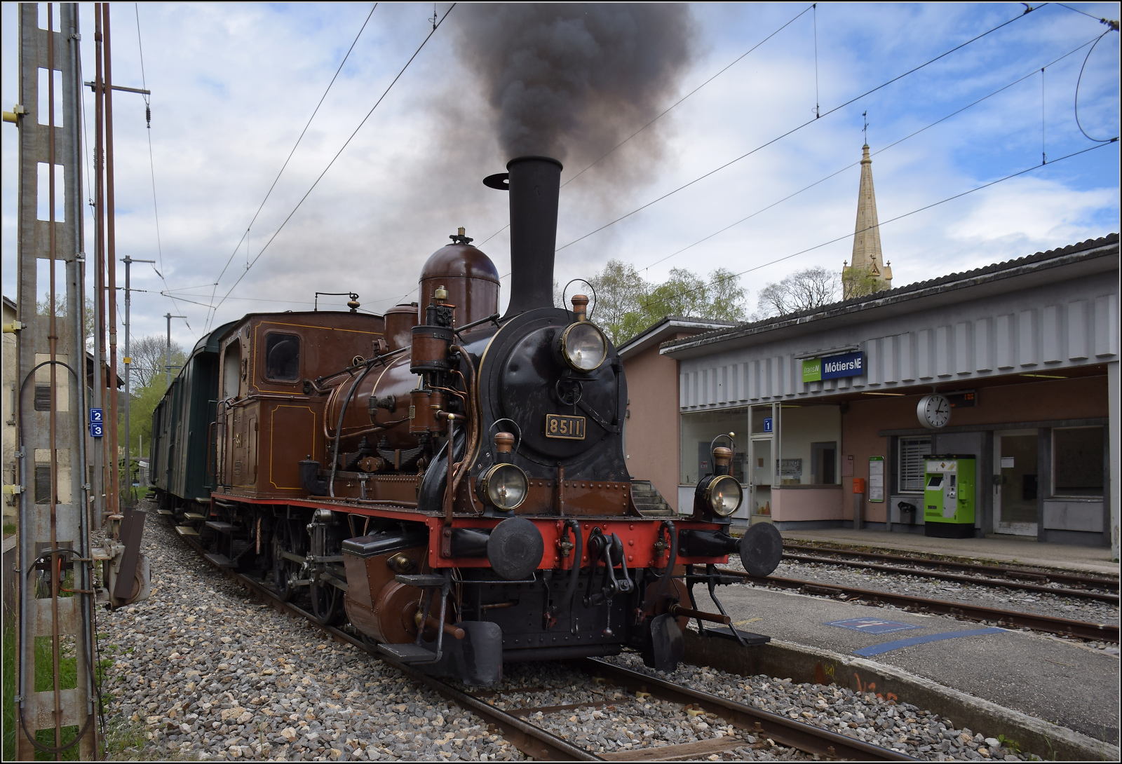 Train au fil de l'Areuse.

E 3/3 5811 in Môtiers. Das historisch bedeutsame Münster ist leider kaum in ein Foto zu integrieren. Lediglich die Kirchturmspitze ragt ins Bild. Angesichts des bevorstehenden Streckenumbaus darf bei diesen Bildern der Dampfzug die Nebensache sein. Mai 2024.