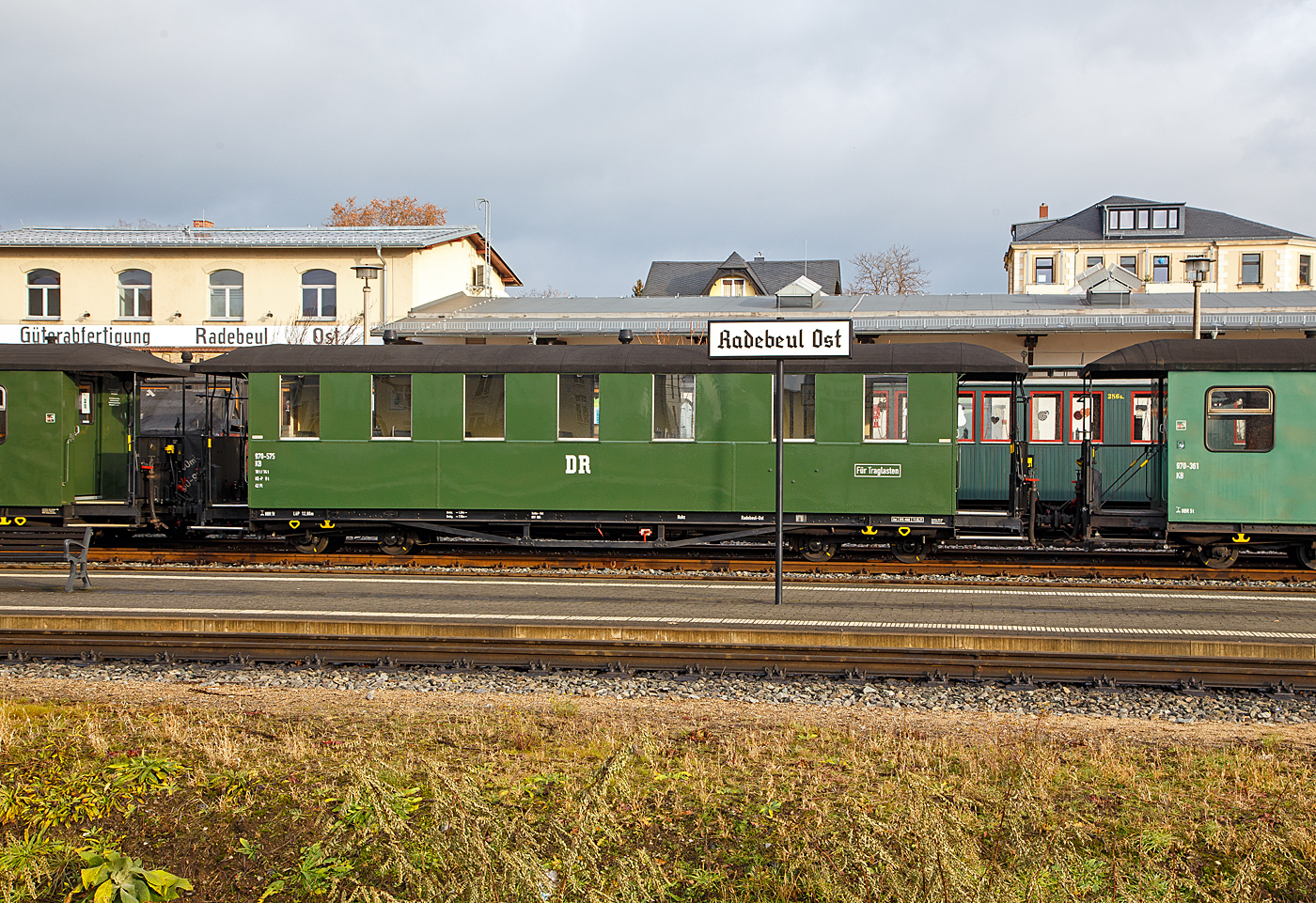 Vierachsiger 750 mm-Schmalspur 2.Klasse Altbau Personenwagen mit Traglastenabteil, offenen Plattformen und Holzdach, SDG 970-575 (ex DB 970-557, ex DR 970-557), der Gattung KB4 tr, der SDG - Schsische Dampfeisenbahngesellschaft mbH abgestellt im Zugverband am 07.12.2022 beim Schmalspur-Bahnhof Radebeul Ost (Lnitzgrundbahn). Hier in der ehem. DR Erscheinungsbild. 

Der Wagen wurde 1926 von der von der Waggon- und Maschinenfabrik Aktien-Gesellschaft vorm. Busch in Bautzen gebaut. Er ist als Traglastenwagen (fr Kinderwagen etc.) ausgefhrt. Die Altbau Ausfhrung kann man gut an den Fenstern erkennen, zum ffnen wird hier die ganze Scheibe noch unten geschoben.

Diese in den zwanziger Jahren gefertigten Wagen, haben gegenber den Erstserien nun blechbeplankte Auenwnde. Auch hielten Dampfheizung und Saugluftbremse Einzug. Die bei der Deutschen Reichsbahn verbliebenen Wagen wurden teilweise umgebaut und technisch angepasst. Ende der siebziger Jahre wurde ein Teil der Wagen modernisiert. Diese erhielten dabei ein vllig gendertes ueres Erscheinungsbild. Mehrere dieser Traglastenwagen sind heute noch bei verschiedenen schsischen Schmalspurbahnen und Museumsbahnen im Einsatz.

Die lteren Nummern der Deutsche Reichsbahn (1950 - 1958) 7.xxxx, der Deutsche Reichsbahn Gesellschaft / DR (1927 - 1950) K 3xx, sowie der Kniglich Schsische Staatseisenbahnen (1913 – 1927) xxx K, sind mir leider unbekannt.

TECHNISCHE DATEN:
Spurweite: 750 mm
Anzahl der Achsen: 4
Lnge ber Puffer: 12.800 mm
Drehzapfenabstand: 7.500 mm
Achsabstand im Drehgestell: 1.300 mm
Eigengewicht: 10 t
Sitzpltze: 42 (in der 2. Klasse)
Bremse: KE-P