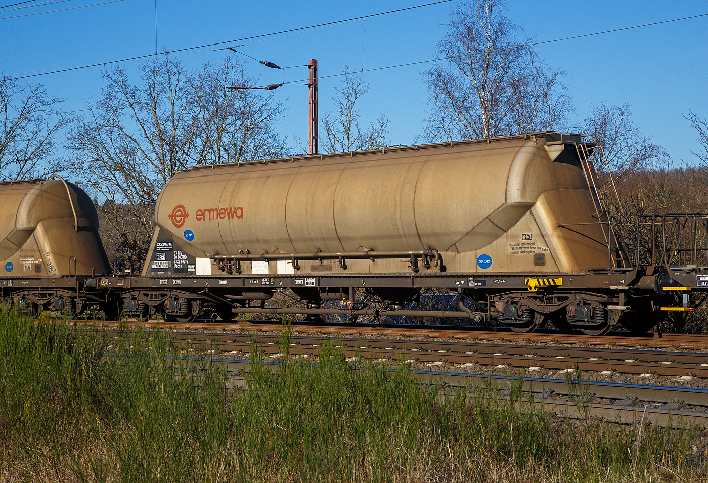 Vierachsiger 80m³ Silowaggon für SO 143 - Aluminiumoxid (Drehgestell-Staubgutwagen) 33 80 9326 673-6 D-ERMD, der Gattung Uacns (Type 6924 B0), französischen Vermietungsfirma ERMEWA S.A., am 07.02.2023 im Zugverband bei einer Zugdurchfahrt bei Wilnsdorf-Rudersdorf.

TECHNISCHE DATEN:
Hersteller: Feldbinder Spezialfahrzeugwerke GmbH, andere Quellen scheiben WB Graaff (1987) als Hersteller, dies kann sich aber nur aufs Fahrgestell beziehen, denn ich kann am Silo deutlich „Feldbinder“ lesen.
Gattung:  Uacns
Spurweite: 1.435 mm
Länge über Puffer : 18.100 mm
Drehzapfenabstand: 13.070 mm
Achsabstand im Drehgestell: 1.800 mm
Höchstgeschwindigkeit: 100 km/h 
Gesamtvolumen: 80 m³ (80.000 l)
Eigengewicht:  18.800 kg
Nutzlast:  71,2t (ab Streckenklasse D)
zul. Gesamtgewicht:  90,00 t
Max. Betriebsdruck: 2,50 bar 
Kleinster bef. Halbmesser:  36 m
Bremse: KE-GP-A (LL)
Bremssohle: IP 116
Intern. Verwendungsfähigkeit: RIV

Die Bedeutung der Gattungs- und Kennbuchstaben (hier Uacs):
U - Sonderwagen 
a - mit vier Radsätzen
c - mit Entladung unter Druck
n – bei mit vier Radsätzen höchste Lastgrenze über 60 t
s - Höchstgeschwindigkeit 100 km/h (beladen)