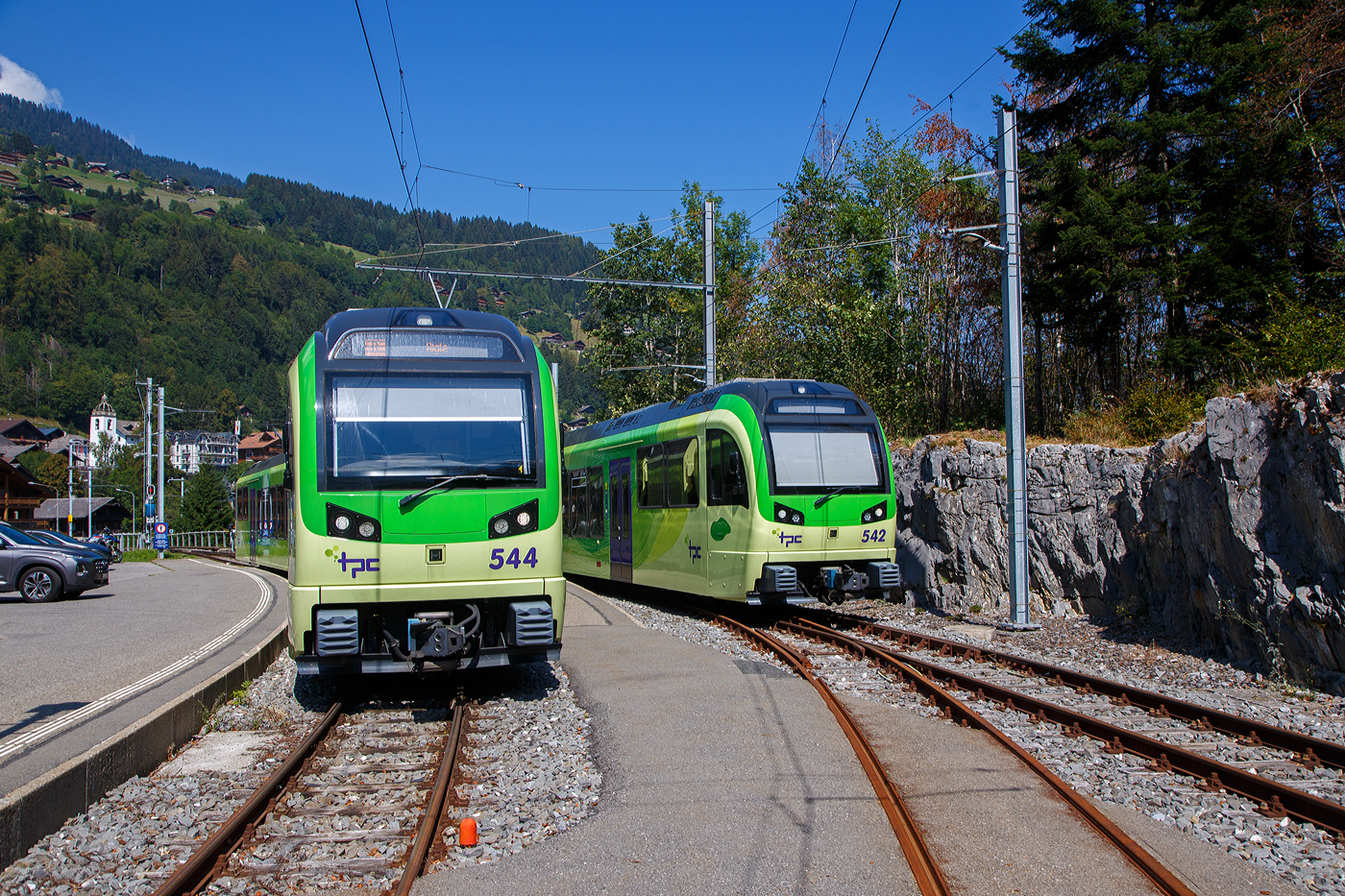 Zwei tpc AOMC/ACD Beh 2/6 meterspurige Triebzüge mit gemischtem Adhäsions- und Zahnradbetrieb vom Typ Stadler SURF stehen am 08 September 2023 im Endbahnhof der AOMC in Champéry (1.037 m ü. M.). Links der Triebzug 544 und rechts 542. SURF steht für Série Unifiée Romande pour Réseau Ferré métrique (Einheitliche Serie für das Westschweizer Meterspurige Schienennetz).

Die AOMC (Chemin de fer Aigle–Ollon–Monthey–Champéry, deutsch Aigle-Ollon-Monthey-Champéry-Bahn, war eine Eisenbahngesellschaft in den Schweizer Kantonen Waadt und Wallis. Sie entstand 1946 aus der Fusion der 1907 eröffneten Chemin de fer électrique Aigle–Ollon–Monthey (AOM) mit der 1909 eröffneten Chemin de fer Monthey–Champéry–Morgins (MCM) und fusionierte 1999 zu den Transports Publics du Chablais (TPC).

Die 23,4 Kilometer lange Strecke der verbindet Aigle durch das Rhonetal mit Monthey (reine Adhäsionsbahn) und führt anschließend als Bahn mit gemischtem Adhäsions- und Zahnradbetrieb nach Champéry im Val d’Illiez. Oben direkt neben dem Endbahnhof Champéry befindet sich die Talstation der Luftseilbahn Champéry-Croix de Culet (Planachaux). 

Im Sommer 2016 wurde die Strecke umfassend modernisiert. Dabei wurden die Zahnstangenabschnitte vollständig erneuert und das bisherige Zahnstangensystem Strub durch Abt-Zahnstangen ersetzt. Weiter wurde die Fahrleitungsspannung von 950 auf 1500 V erhöht. Somit besitzen alle ab Aigle verkehrenden Strecken der TPC das gleiche Zahnstangensystem und die gleiche Spannung. Der Verkehr wird nun vollständig mit den neu abgelieferten Beh 2/6 541–547 abgewickelt. Von den bestehenden Triebfahrzeugen der AOMC wurden einzig die beiden im Jahr 2001 gelieferten Doppeltriebwagen Beh 4/8 591–592 an das neue Zahnstangen- und Stromsystem angepasst.
